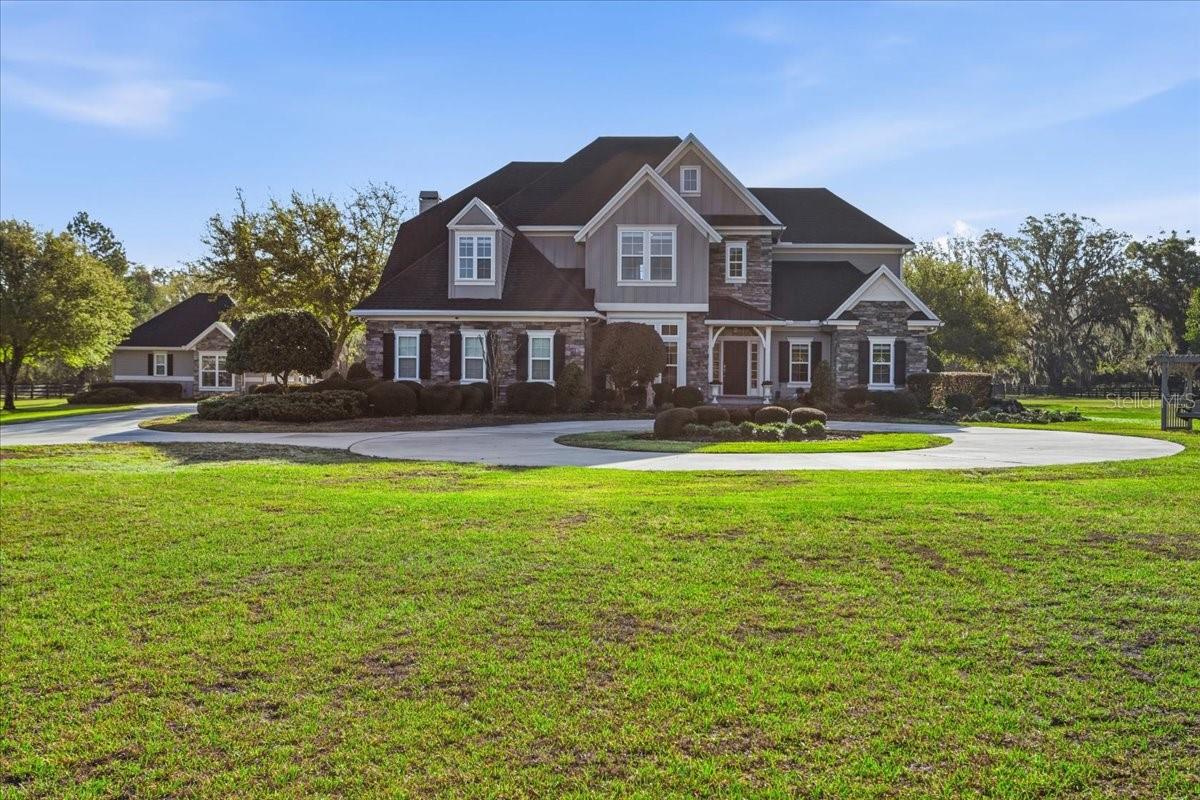 Custom Warring Homes estate home and guest house on 5 picturesque acres in the gated community of Red Oaks Estates located off scenic County Road 241 and NW 94th Avenue. Only minutes to Jonesville, I-75 and the City of Alachua.  When you enter Red Oaks Estates; you will be greeted by a stately community gate welcoming you to this beautiful equestrian  community. The home is absolutely pristine and shows like it was built today. This 5235 square feet estate is comprised of a 2012 custom-built main home featuring two-stories with 4 bedrooms, 4.5 bathrooms, a bonus room (or 5th bedroom), dedicated office, formal living room, great room, formal dining room, an upstairs great room/media room, two fireplaces, laundry rooms on both floors and a three car garage. The detached guest house was built by Warring Homes in 2015 and features a paver walk-way, two bedrooms, one bathroom,  full kitchen, living area, laundry room and a covered patio and fenced yard. The entire five acres is fenced as well as the backyards of each home are fenced with black aluminum fencing. 
As soon as you enter the main house; you are greeted by a stunning two-story foyer, a view of the formal dining room and leading to the formal living room surrounding a gas fireplace with ornate wood custom mantle & stone covered fireplace. The formal living room has coffered ceilings, built-in cabinetry and French doors leading to a covered brick back porch and paver patio. The kitchen is a chef’s dream kitchen with a spectacular island, quartz countertops, white subway tile, top of the line custom Busby Cabinetry, butler’s pantry and high-end luxury appliances. The kitchen is plumbed for gas if buyer desires a gas range. Off the kitchen is a spacious breakfast nook as well as the family room with a dramatic vaulted ceiling and wood-burning fireplace with custom built-in’s surrounding the fireplace.  The primary bedroom is downstairs and has an ensuite bathroom with a walk-in shower, jetted tub, double sinks, and a large walk-in closet with two designated areas. Head upstairs to 3 guest rooms, a bonus room (or 4th guest room), 3 full bathrooms, an impressive office with built-in cabinetry, and a large family room with vaulted ceilings, and a wet bar. All bedrooms have walk-in closets. The main house also features a generator which can power almost 2/3 of the main house in case of power outage. The guest house is perfect for houseguests or multi-generational living as it has 2bedrooms/1bathroom and features an open floor plan, kitchen island, a built-in daybed with storage underneath, and two sets of French doors that lead to a covered patio and fenced yard (separate from the main house). It also has its own generator in case of a power outage. Say goodbye to GRU Electric and enjoy Clay Electric, City of Alachua trash service, high-speed Windstream internet & DirectTV, and Suburban Propane for gas. Interior freshly painted, new flooring installed, new well pump and water tank, new gutters and recently pumped both septic tanks. There are not enough words to describe every detail of this quality constructed custom home by Warring Homes.