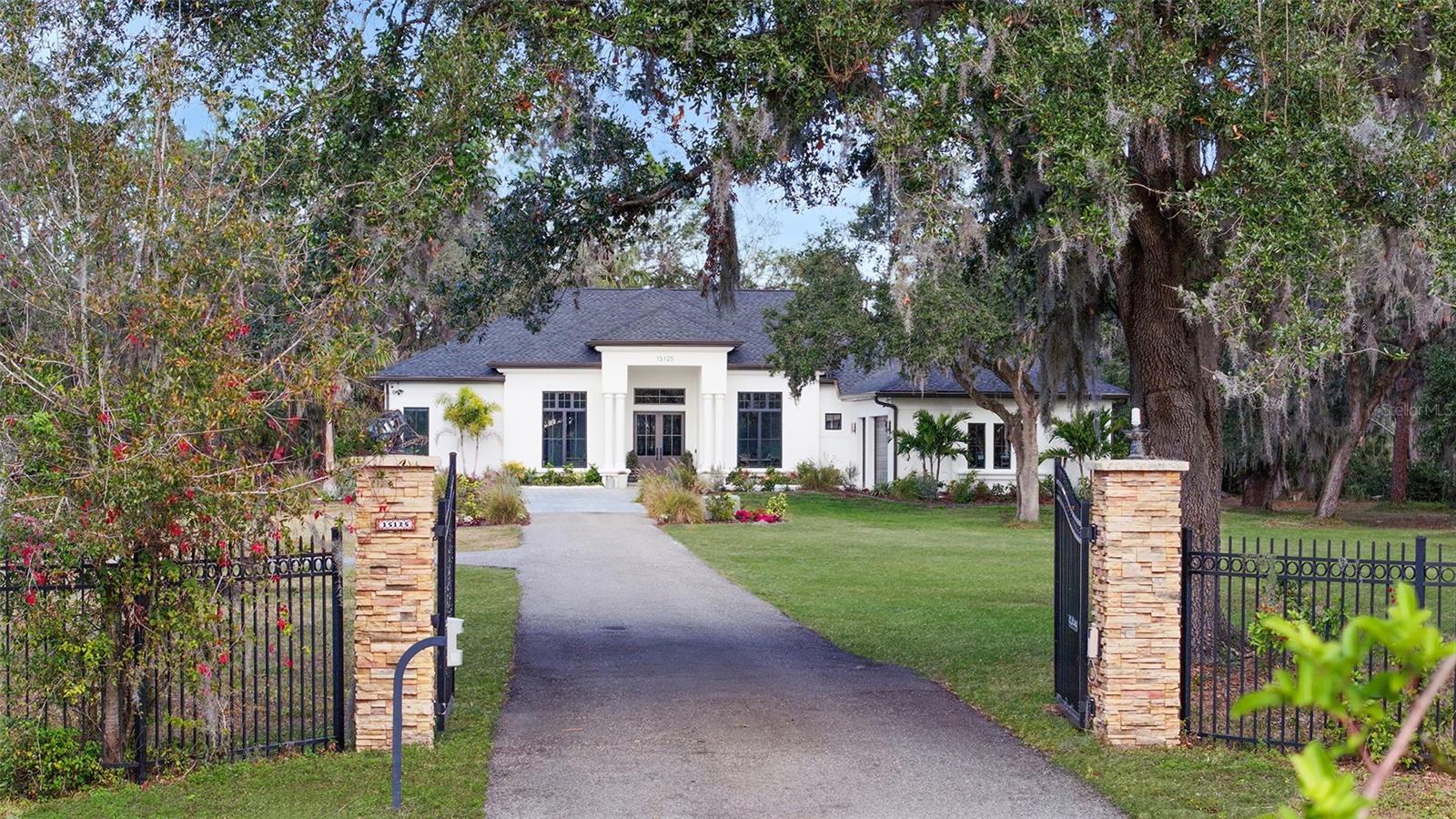 This stunning 4,100-square-foot dream home sits on 8.5 secluded acres and offers both modern elegance and practicality. Featuring 4 bedrooms, 4.5 baths, and garage space for 6 cars, the property includes an attached 3-car garage and a separate detached 3-car garage, perfect for use as a workshop or additional storage. The home features a private mother-in-law suite with an en-suite bathroom and an oversized walk-in closet, making it ideal for guests or multi-generational living. The luxurious primary suite includes his-and-her walk-in closets with custom built-ins, and the spa-like primary bathroom boasts a soaking tub, a spacious walk-in shower, and exquisite finishes. The gourmet kitchen is a chef’s dream, complete with a custom oversized range hood, soaring white oak cabinets, a walk-in pantry with built-in shelving, Dacor appliances, a built-in fridge and freezer, a double oven, and a kitchen nook. Adjacent to the formal dining room, you’ll find a coffee bar, a dry bar with a wine fridge, and a beverage fridge for effortless entertaining. Step outside to the expansive lanai, where a summer kitchen with a built-in grill creates the perfect space for outdoor cooking and dining. Recent upgrades include hurricane-impact windows, a new roof, a 2022 HVAC system, a new paver driveway, and a beautifully curated landscaping package. Interior highlights include custom built-ins, solid wood doors, feature walls, electric blinds, high-end lighting, and an abundance of storage throughout. The sleek, warm, and inviting design is complemented by a modern aesthetic. With no HOA or CDD fees, this property offers tranquility and privacy while being just minutes from conveniences like a new Publix, Costco, the interstate, and more. This rare opportunity combines the quiet beauty of nature with easy access to urban amenities. Don’t miss this one—it won’t last!