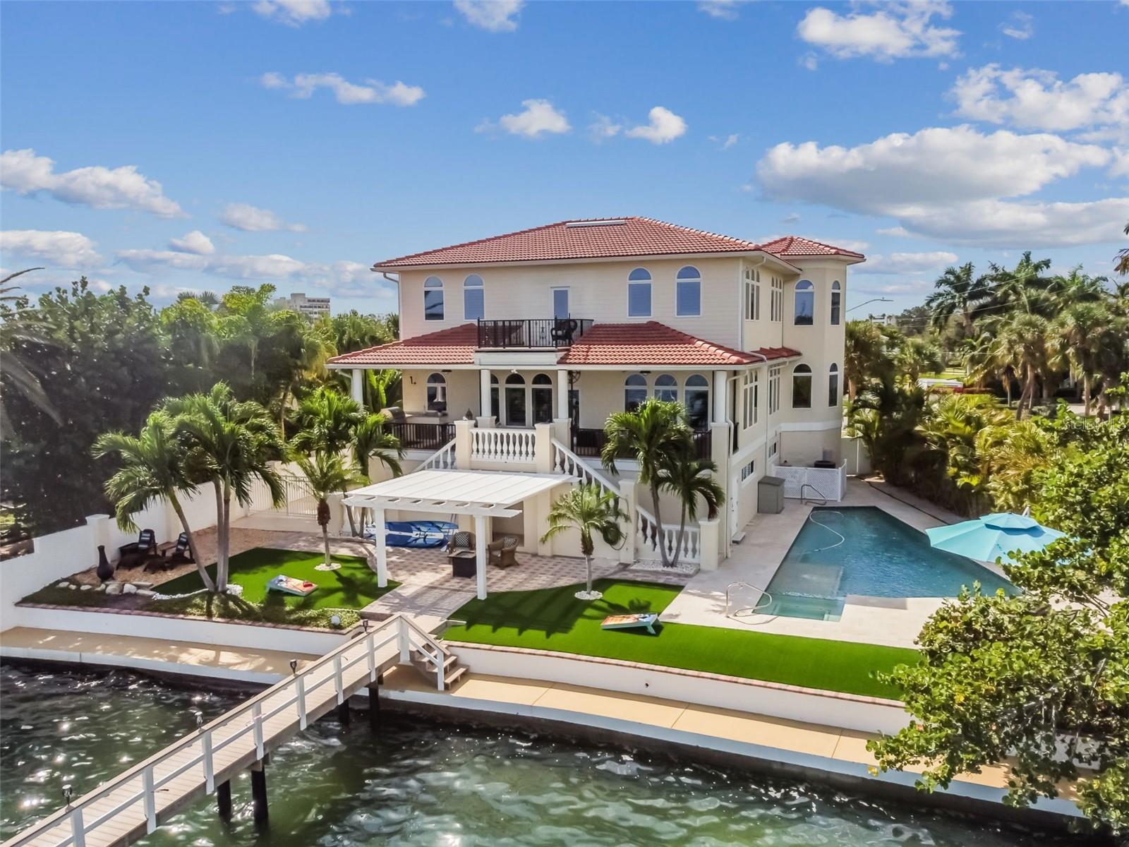 Nestled along its pristine shores and offering sweeping views, awe-inspiring sunrises, regular visits from manatees and dolphins, as well as unobstructed access to the Gulf of Mexico, this property is a true waterfront dream. This residence has been meticulously remodeled and professionally designed with an impeccable sense of style, highlighting unmatched craftsmanship and attention to detail in every corner. This stunning 3-bedroom, 3.5 bathroom home offers 3,181 square feet of living space and includes two well-appointed offices. Additionally, there are over 1,000 additional square feet of air-conditioned living space on the terrace level, which can serve as an excellent setting for a home theater, game room, home gym, or even a yoga studio. The main floor living space welcomes you with an open and inviting living room, graced by a linear plasma fireplace, built-in bookshelves, ceiling fans, and custom window treatments. An attached turret office/library offers an ideal space to work from home. The modern kitchen offers stunning bay views and is meticulously designed with a perfect blend of style and practicality, with fine custom cabinetry throughout. There is a formal dining room adorned with stunning tray ceilings and, for a more relaxed dining, a charming dining area is situated adjacent to the kitchen. The extremely spacious primary suite includes views in every direction, a walk-in closet, and a recently remodeled ensuite bathroom with a soaking tub and an enormous walk-in shower. The upper level also features a second turret office/library, two more bedrooms, and a jack-and-jill full bath. The beauty of this property extends outdoors with an oversized 420 sq ft waterfront veranda; equipped with an outdoor Blaze kitchen and fridge, a waterfront pergola, an upper-level "Lido Deck," and several porches, which allow you to relish stunning sunrises, full-moon rises, and "moon pennies" across the bay, all offering views of Boca Ciega Bay, Dolphin Cove, and downtown St. Petersburg. This property features a state-of-the-art heated saltwater pool, expertly designed and constructed by the renowned Landmark Pools of Tampa. The pool offers a dedicated lap lane for your aquatic workouts, a swim-up cocktail area, and dual shallow ends perfect for a competitive game of volleyball. Furthermore, the expansive infinity-edged spa offers dual-level seating, providing ample space for relaxation and socializing. As the sun sets, the pool and spa come alive with vibrant, state-of-the-art LED lighting, creating a magical atmosphere for evening gatherings and parties. The home also includes a workshop, an oversized two-car garage, abundant off-street parking, gated boat/RV parking and multiple storage areas throughout. It boasts various upgrades, such as a brand-new tile roof (installed in 2023), a new Speeler dock (2021), a 20K Neptune lift (upgradable to 30K, installed in 2021), a new pool/spa (2018), new HVAC systems (2018), and low-maintenance lush landscaping. A clean 4-point inspection was recently performed and is available for review. With its ideal location near pristine Gulf beaches and the vibrant coastal lifestyle, along with easy access to all the dining, shopping, and entertainment that St. Pete Beach offers, you'll be living in paradise.
