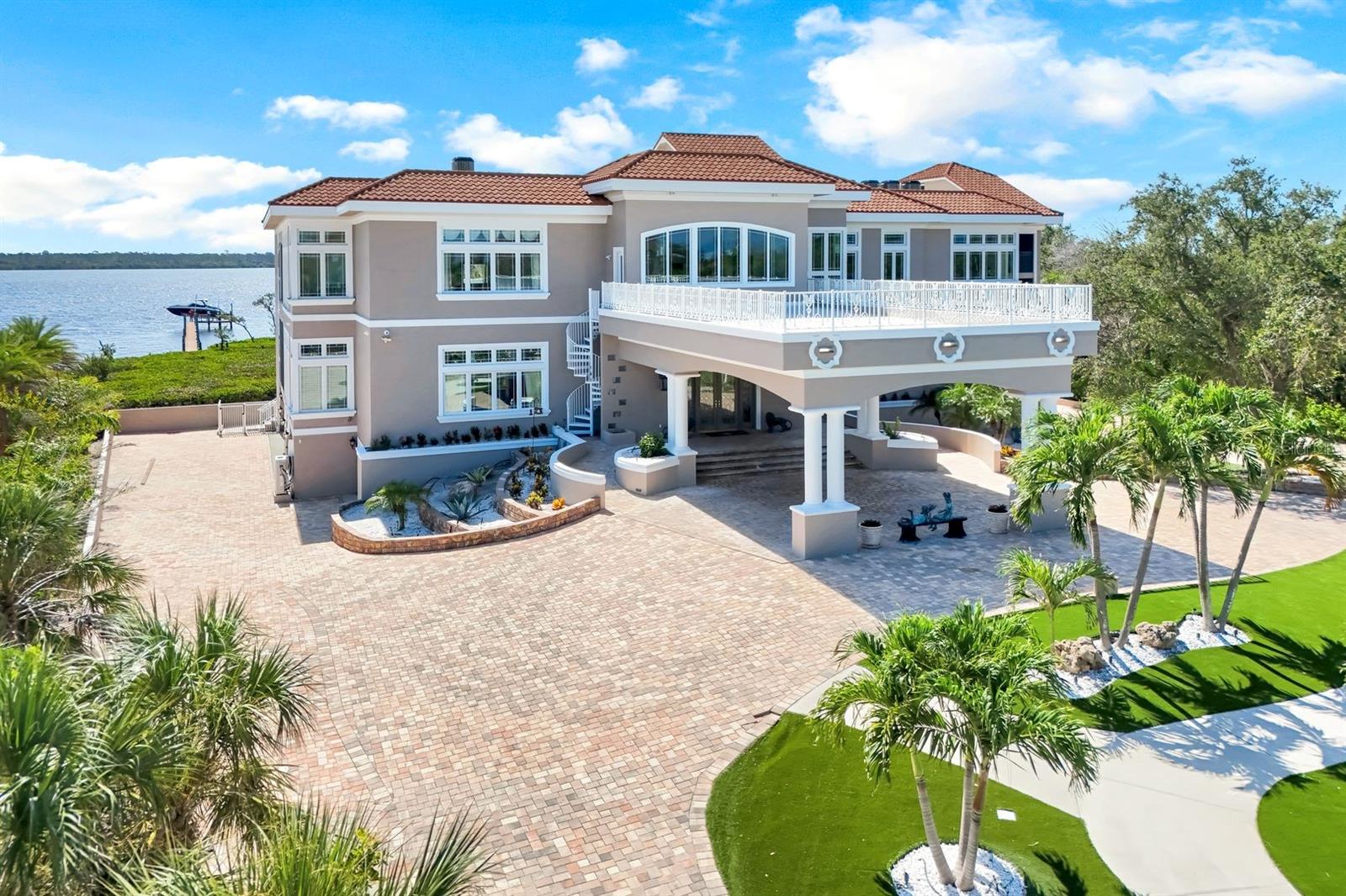 There are homes you can understand online, and then there are homes you must walk through to truly feel. This is one of them.

Set on nearly 3 private acres along Lemon Bay, this gated Mediterranean-inspired estate spans 12,789 sq. ft. of resort-style living with unmatched amenities on Florida’s Gulf Coast, all within this private estate. Enter through grand gates and follow a sweeping driveway framed by mature oaks, tranquil ponds, waterfalls, and curated sculptures. The grounds include manicured lawns, a putting green, bocce and volleyball courts, and expansive outdoor recreation. A dramatic porte cochère introduces a soaring two-story foyer with double glass doors, stained-glass transoms, and a glass elevator. Interiors showcase coffered and tray ceilings, stately columns, marble and travertine floors, extensive millwork, and eight fireplaces. The home offers six ensuite bedrooms, 9.5 total baths (primary bath has 3 bathroom sections but counted as 1 in the total), a library with wet bar, a media/family room with projector, fitness and meditation rooms, and rooftop terraces designed for sunset and Gulf views. The chef’s kitchen features dual islands, Sub-Zero and Wolf appliances, wine fridge, ice maker, and walk-in pantry, flowing seamlessly into both formal and casual dining areas. The primary suite includes bay views from a private screened terrace, fireplace, sitting area, spa-like bath, and custom closets, while guest suites offer private balconies, walk-in closets, and baths. Outdoor living is highlighted by a 30×50 resurfaced saltwater pool and spa, full outdoor kitchen, shaded terraces, pool bath, and recreation courts. The property extends to a private dock with boat lift and deeded Gulf beach access. A tiled garage provides capacity for up to 30 vehicles, complete with 10 mini-split A/C systems and extensive storage, ideal for collectors or large-scale entertaining.
