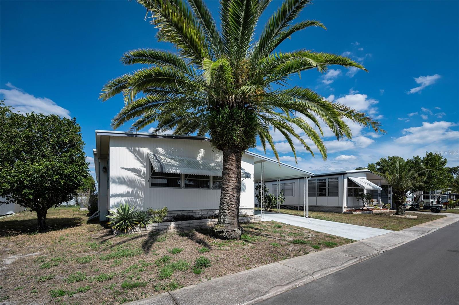This absolutely charming home is nestled in the sought-after Tanglewood Mobile Village Condominium. Unlike many similar subdivisions, the land is owned, not leased. A 55+ community, residents will enjoy a multi-amenity lifestyle that includes a safe, pet-friendly park along with shuffleboard and horseshoe courts, a heated community pool and a clubhouse. Additional huge advantages include a very reasonable HOA fee ($143/month) which includes trash removal, lawn maintenance, the amenities, and their care. An ideally quiet enclave close to US Highway 19’s restaurants and retail but far enough away to ensure serenity, you’ll enjoy proximity to the local beaches but still reside in a no flood zone. Because no leasing is permitted, you’ll appreciate the stability of a neighborhood in which everyone is invested. Inside this happy home, pride of ownership shines. Fabulous upgrades are evident throughout including a NEW heat pump (2019), NEW vanities in both baths (2019), NEW laminate flooring almost everywhere (2020), NEW kitchen appliances and sink (2020), and a NEW water softener (2024). Light and bright, the spacious living room is welcoming with its open concept plan. A total of (4) ceiling fans complete with light kits adorn the ceilings in both bedrooms, living room, and dining room; classic Levolor blinds dress the windows. The large, windowed dining room boasts stunning cabinetry with mirrored backing to beautifully showcase mementos. You’ll love the sleekly designed kitchen that offers a modern vibe and stainless-steel appliances. Combined with the adjacent family room, this space is the heart of the home for entertaining and supporting your treasured relaxation. Both baths are wonderfully appointed with linoleum flooring in the guest shower/toilet room; laminate flooring in the master bath. A set of sliders introduces the enclosed, temperature-controlled Florida room, surrounded by windows and rich with sunshine. The screened porch off the driveway reveals an expansive storage room that includes a washer and dryer. Lanark Drive is not just a place to live. It’s a place to love.