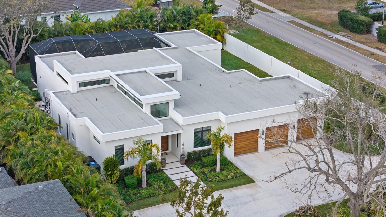 An Oyster Bay masterpiece, where legacy homes and new architectural statements coexist, this striking modern residence delivers volume, spatial continuity, and refined indoor/outdoor living just minutes from Siesta Key, dining and boating. Built in 2023 and thoughtfully composed on a single level, the home balances bold contemporary design with privacy, warmth and livability. A dramatic entry introduces soaring ceilings and immediate visual impact, opening into expansive living spaces designed for daily life and entertaining. Walls of glass, disappearing corner sliders, and ceiling heights approaching 17 feet create a sense of scale and light rarely achieved, while wide plank French oak flooring and curated designer lighting provide continuity throughout. The kitchen is a centerpiece, anchored by an oversized island and outfitted with high-end integrated appliances, custom cabinetry and a full walk-in pantry. It flows seamlessly into the great room and wet bar, making the home equally suited for quiet evenings or larger gatherings. Outdoor living takes center stage. The screened lanai features a fully equipped summer kitchen, generous covered seating and dining areas, and a resort-style heated saltwater pool and spa with fire bowls and cascading water features. Lush tropical landscaping, a precast concrete privacy wall, and a fully fenced yard create a sense of retreat while maintaining openness and light. The owner’s suite is a private sanctuary with direct lanai access, dual custom closets and a spa-inspired bath. Three additional en-suite bedrooms include a poolside cabana-style suite ideal for guests, while a dedicated office or den offers flexibility for work or relaxation. Additional highlights include a three-car garage with epoxy flooring and storage systems, impact-rated windows and doors, smart home automation, whole-house generator, tankless water heaters and refined finishes throughout. This is a modern Sarasota residence designed for those who value architecture, flow, and lifestyle in one of the city’s established and sought-after neighborhoods.