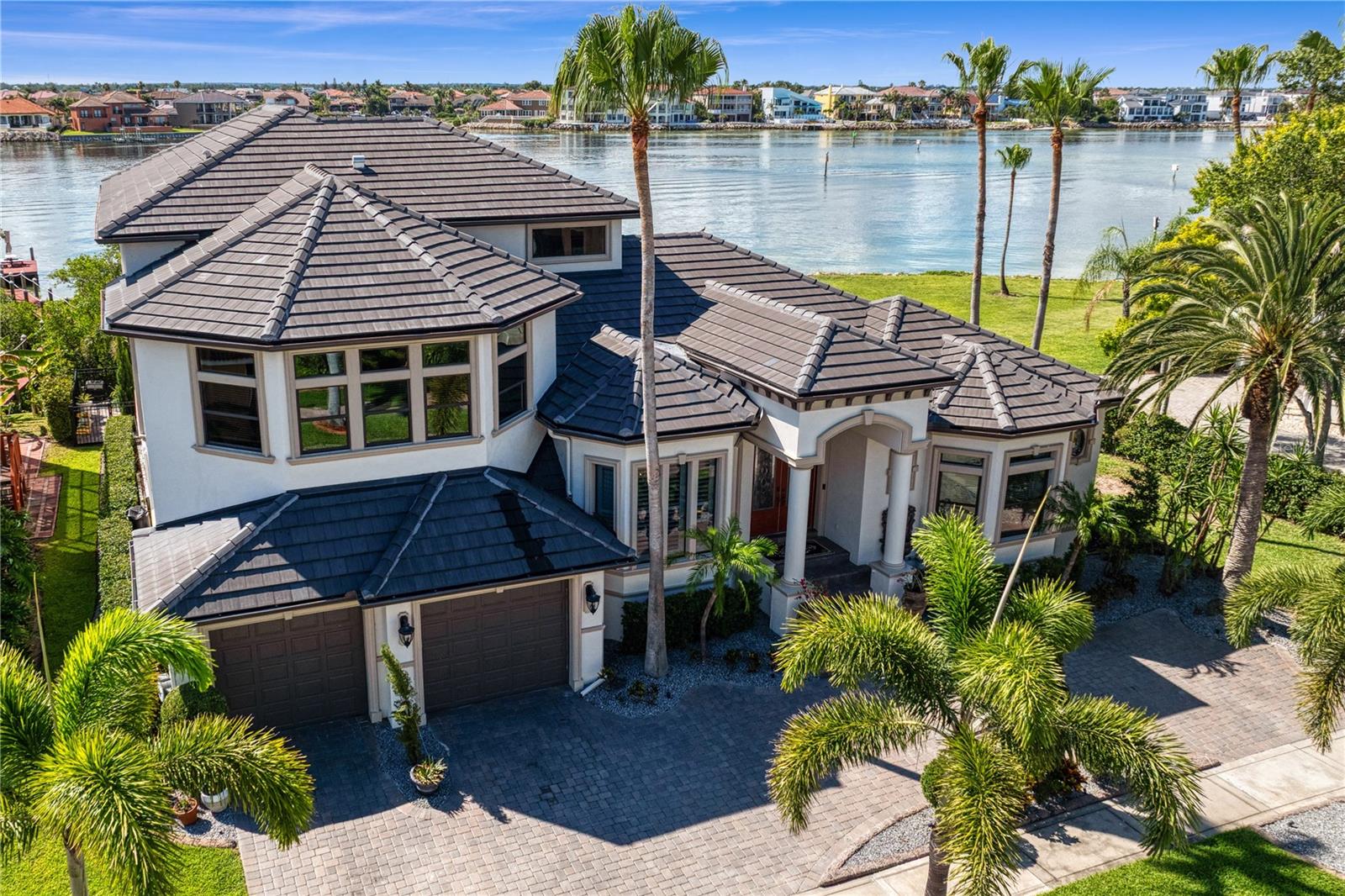 The Pinnacle of Andalucia Bayfront Living. Poised on open sailboat water, this extraordinary estate captures sweeping, unobstructed bay views and breathtaking sunsets. Set on 84 feet of premier bay frontage, the property offers unmatched privacy within the guard-gated Andalucia community. Designed for grand-scale entertaining and refined coastal elegance, this 4,820 sq. ft. 4 Bedroom, 6 Bath residence makes a striking first impression with a circular paver driveway and custom landscape and lighting. Inside, curated luxury finishes and a light-filled great room with a gas fireplace seamlessly flow through massive triple sliding doors to an expansive covered terrace—delivering the ultimate indoor-outdoor waterfront lifestyle. The chef’s kitchen is a culinary masterpiece, featuring a center island with an integrated cooktop, breakfast bar, and a casual dinette. Perfectly positioned for effortless entertainment, it flows seamlessly into a fully equipped wet bar boasting a wine refrigerator, dedicated dishwasher, sink, bespoke wine cabinetry, and raised bar seating. The thoughtfully designed first floor introduces grand spaces for hosting, including a sophisticated formal living room and a stately dining room. Essential amenities include a separate culinary pantry and a dedicated laundry studio. Accommodations on this level are exceptionally generous, comprising three full guest suites—each with its own dedicated bath—plus a stylish powder room. The entire second floor is dedicated to luxury and leisure. It features a spacious game room alongside the palatial primary suite—a private sanctuary boasting panoramic bay views and a secluded balcony with its own cozy fireplace. The spa-like primary bath features a deep soaking sports therapeutic tub, a walk-in shower, and a double vanity, complemented by an expansive walk-in closet. For ultimate convenience, the suite also includes dedicated, private washer and dryer hookups. The backyard is a resort-style oasis designed for the ultimate Florida lifestyle. An expansive patio leads to a luxury pool and a fully equipped exquisite outdoor kitchen and a built-in pizza oven. Gather around the custom sunken seating area and fire pit for unforgettable evenings, or head down to the private dock, which features two boat lifts and offers immediate access to open sailboat water. Beyond the gates, residents of Andalucia enjoy an unparalleled neighborhood lifestyle with exclusive access to a private bayfront clubhouse, a resort-style community pool, jetty, yacht club and lighted tennis courts. The neighborhood also features beautifully landscaped bayfront common areas and a private playground, adding to the community's coastal charm.