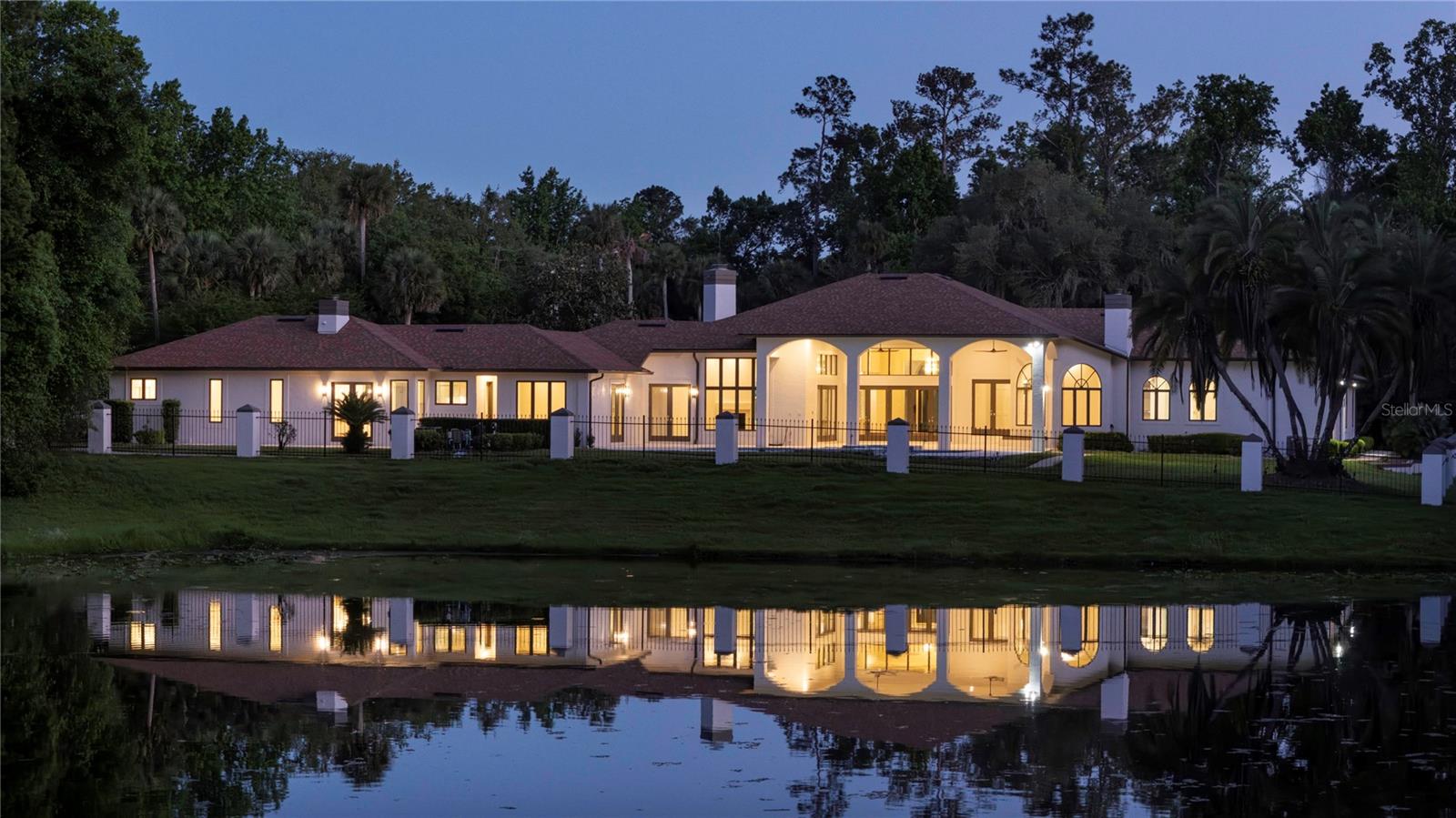 At the end of a quiet cul-de-sac and backing to the protected beauty of Wekiwa Springs State Park, this extraordinary waterfront estate offers a rare blend of privacy, scale and natural serenity in the desired Markham Woods Corridor. Fully fenced and positioned to capture sweeping conservation and water views, the setting alone places this residence in a category few can match. Impressive private gates and a brick paver circular drive introduce a dramatic arrival, where a grand porte-cochere and expansive six-car motor court set the tone. Inside, the home has been completely reimagined through a comprehensive renovation, unveiling soaring ceilings, walls of glass and abundant natural light. A striking 5-by-8-foot pivot door opens to a refined foyer with porcelain tile and white oak flooring, immediately drawing the eye to the shimmering pool and tranquil pond beyond. Designed for grand entertaining and effortless living, the main areas unfold in a seamless open-concept layout. With 14-foot ceilings and expansive living, dining, family and kitchen spaces flowing together, the home offers impressive volume and connectivity. Anchoring the heart of the home, a dramatic double-sided wood-burning fireplace creates a warm focal point between kitchen and family room. The chef’s kitchen is a showpiece, featuring Wolf appliances, built-in refrigeration and an oversized island with seating for six, finished with elegant waterfall-edge countertops. Outdoor living is equally captivating. A vast travertine lanai transitions to an oversized resort-style pool, all set against a breathtaking backdrop of water and untouched conservation. Nearly every room is oriented to capture these remarkable views, creating a constant connection to the landscape. The primary suite is a sanctuary of grand scale, offering serene water and wooded vistas. Its bespoke bath features leather-finished stone countertops, dual vanities, a soaking tub, and picture windows framing the natural setting. A spa-inspired steam shower with multiple shower heads and a built-in bench completes the experience. Dual custom walk-in closets elevate functionality, one with a center island and scenic window, the other concealing a hidden safe room. Versatility defines the additional spaces. A dedicated office with walk-in closet and direct bath access can serve as an additional bedroom. A generously sized bonus room is ideal for a home theater, library or lounge, while a separate gym with luxury vinyl flooring can easily function as a second office. A thoughtfully positioned flex space between the main residence and guest quarters opens to the lanai and pool bath, ideal for a cabana lounge or wellness retreat. The guest quarters is a residence unto itself, featuring two bedrooms, two baths, a spacious great room, full kitchen with center island, separate motor court access, and its laundry, offering exceptional accommodations for guests or multigenerational living. Homes of this caliber rarely come to market. The extensive renovation, remarkable scale, and exceptional attention to detail are paired with Seminole County’s desirable locations. Zoned for top-rated schools and ideally positioned near Longwood and Lake Mary, with convenient access to major highways, regional hospitals, airports, beaches and Central Florida’s world-renowned attractions, this is a legacy property that defines elevated Florida living.