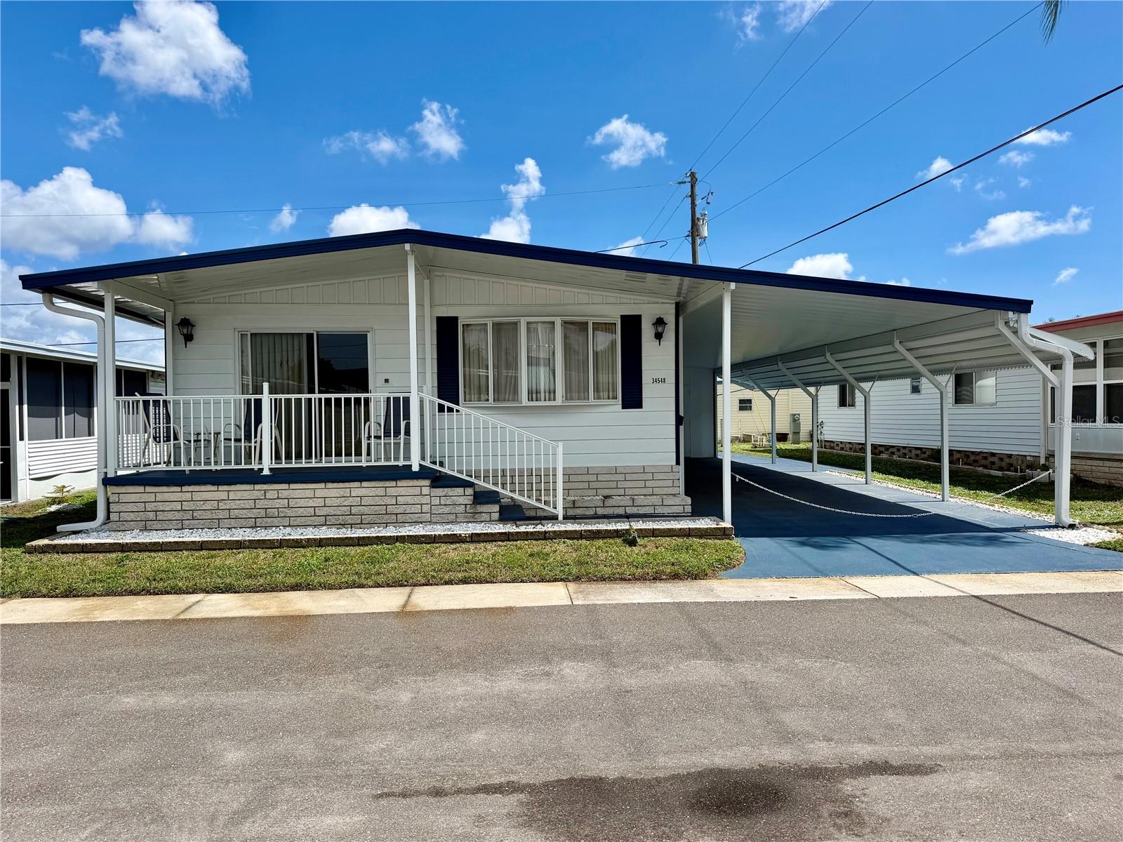 Sunset Palms was rated TOP 5 retirement communities for 2025! Well maintained home with lots of updates: New carport/front porch covering/Gutters/extended carport and painted driveway in 2025… HVAC 8/2024… thermal PANE WINDOWS… fresh exterior paint… recently installed vapor barrier… an aluminum ROOF-OVER in 2008/resealed 2025, partially updated bathrooms, newer o vinyl plank tiles, and part of the home, etc. Home features an inside laundry room, very spacious living area, bedrooms and bathrooms. This price includes the Share, valued at $55,000! Sunset Palms is Inexpensive living at only $210 per month which includes all the amenities one could want; owned clubhouse, escrows are fully funded, beautiful heated pool and spa, fitness center, library, shuffleboard, billiard table, and a small lake at the back of the park, laundry room, and your very own private entrance to the super Walmart… On foot, bicycle or golf cart… Etc., etc. Perfect location; for quick access to the beaches, Downtown St Pete, etc. Just hop on 275, which will get you to the Airports, Sarasota, Tampa, etc.
