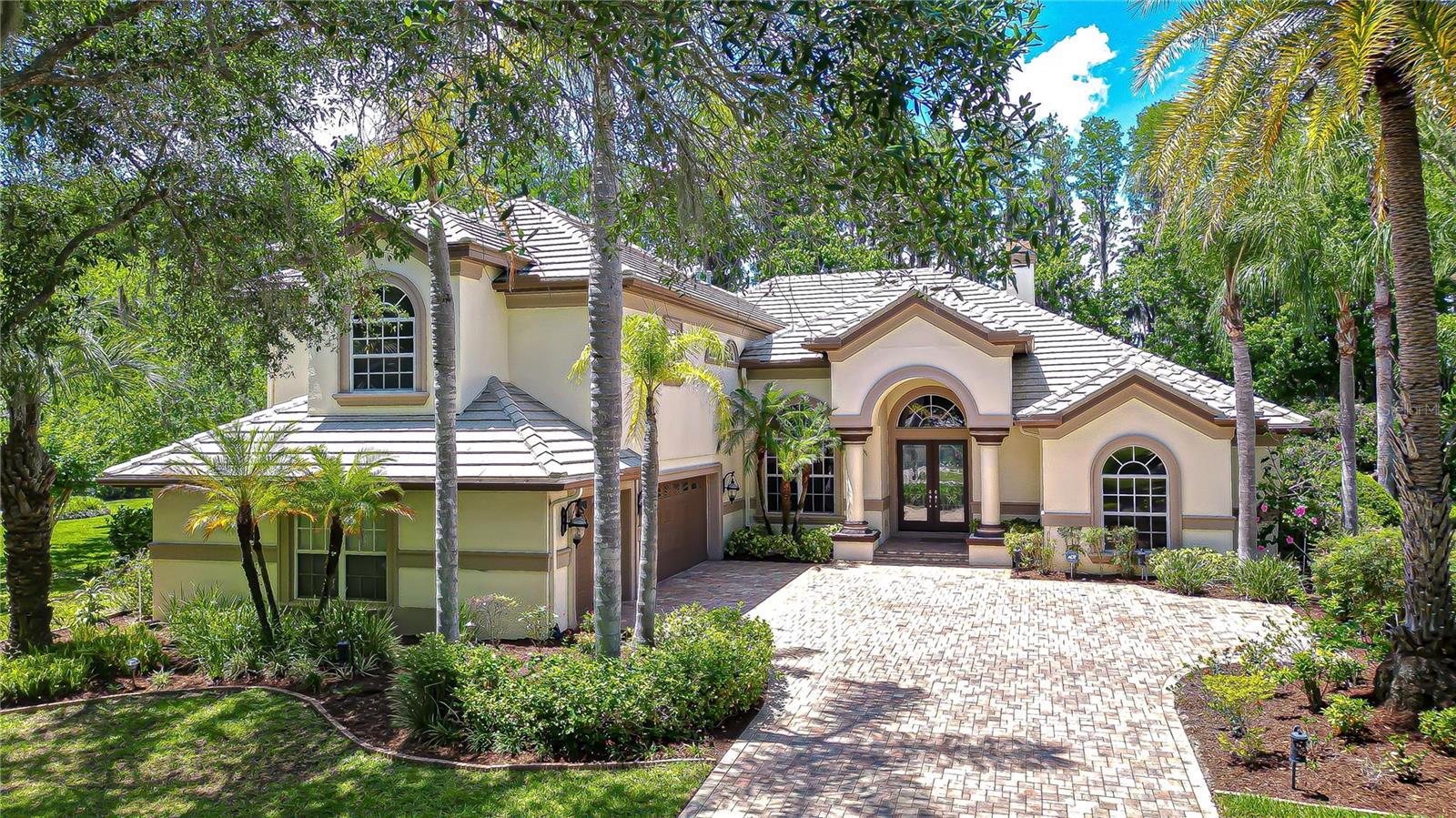 An extraordinary lakefront estate on the shores of Big Lake Vienna, where timeless elegance meets resort-style living in the exclusive gated community of Pasco Sunset Lakes. From the moment you arrive, you’ll be captivated by the artistry of the decorative paver driveway, expansive parking pad, and side-entry 3-car garage, framed by swaying palm trees that guide you to a grand portico entrance adorned with stately columns. Perfectly positioned on a sprawling .388-acre homesite, the property features a private dock, sparkling pool and spillover spa—a true backyard retreat. Step through the impressive 8-foot leaded glass double doors, crowned by an arched transom window, into a soaring tiled foyer highlighted by a hand-painted ceiling medallion and elegant crown molding. Inside, 4,410 sq ft of thoughtfully designed living space showcases soaring ceilings, large-format ceramic tile floors, faux-painted finishes, art niches, rounded corners, and graceful archways—an unmistakable display of architectural craftsmanship. Originally built as a Hannah-Bartoletta model home 2004, lovingly maintained by its original owners, the residence reflects exceptional quality, design, and pride of ownership. The formal living room, anchored by a wood-burning fireplace, captures breathtaking views of the lanai and lake beyond. A refined dining room with an art niche and buffet server sets the stage for memorable gatherings. At the center of the home, the chef’s kitchen is thoughtfully designed for everyday living and effortless entertaining, featuring a suite of stainless KitchenAid appliances—a 5-burner gas cooktop, built-in oven and microwave, and dishwasher. Rich wood cabinetry with crown molding is complemented by a diagonally tiled backsplash, decorative accents, granite counters, spacious center island, breakfast bar, and walk-in pantry. A sunlit “morning room” with bay windows overlooks the serene backyard; the adjacent family room opens seamlessly to the lanai through triple sliding glass doors—creating an indoor-outdoor living experience. Designed with a desirable three-way split floor plan, this home offers privacy and flexibility. The luxurious primary suite is a private sanctuary, complete with a double-door entrance where a decorative art niche and two walk-in closets that opens to the bedroom with a tray ceiling and crown molding, a sitting area with bay windows, and direct lanai access. The spa-like ensuite bath features a double vanity with dedicated make-up space, a jetted garden tub, doorless walk-in shower, and private water closet.
With 6 bedrooms, 5 baths, a dedicated office, and an upstairs bonus loft with its own bedroom and ensuite bath, there is space for multigenerational living or guests—enhanced by abundant, thoughtfully designed storage throughout, including 5 walk-in closets, 8 additional closets, and 2 dedicated storage closets. Outdoors, your private oasis awaits. The screened lanai features a resort-style pool with spillover spa, along with an outdoor kitchen complete with built-in grill, sink, and counter space—perfect for entertaining. Beyond, a lush expansive lawn leads to your private dock extending onto the stunning waters of Big Lake Vienna. Residents enjoy a golf cart–friendly lifestyle with exclusive access to Sunset Lakes Beach Club, featuring pavilions, grills, beach volleyball, playground, dock, and private boat ramp to Big Lake Vienna. Experience elegant, private waterfront living—schedule your showing today.