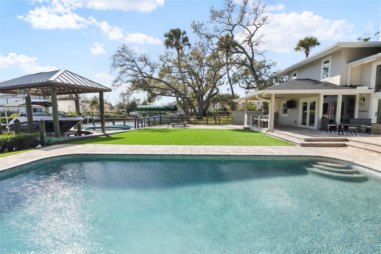 This stunning contemporary was completely TRANSFORMED in 2019 into the ideal entertaining home. The renovation included a new roof, impact rated windows, HVAC systems, plumbing and more!  Tucked away beyond the circular drive on an oversized lot, this beauty does not appear to be 5,621sf, but prepare to be impressed! As you approach the double door entry, note the exterior foyer lending itself to a special welcome for visitors throughout the seasons. Upon entering, take a moment to appreciate the abundance of natural light . Your eyes will be drawn to the wall of windows with views of the expansive back yard and canal. The family room offers space to mingle. Select your favorite bottle of wine from the temperature-controlled display and play a round of pool or relax by the fire. The dining room can accommodate a large dinner party. Guests can also sit and mingle with the chef at the large island. The kitchen features solid quartz counters, a six-burner gas cook top, double oven with speed cook and convection features and ample storage including a walk-in pantry. The French doors lead to a covered patio and outdoor grill with bar seating. Or open the wall of sliders off the family room to the outdoor sitting area. This is where you will want to gather! Imagine the events you can host on the pavered patio spanning over to the sprawling 16x32 feet pool. It's the perfect place to take a dip after a day on the boat. The covered dock offers a 13,000LB BOAT LIFT.  Another unique feature is the 528sf of added deck that is grandfathered on to the property. Back inside, past the powder bath, find a FIRST-FLOOR PRIMARY suite with two walk-in closets. The bath features a dual sink vanity, freestanding tub, and walk in shower. Upstairs features three more secondary bedrooms each with their own baths. The fifth bedroom is a sizable IN-LAW SUITE. It is connected to a spacious media room by a kitchenette. Or guests can enter via the back staircase that leads to the mudroom off the garage. Other features include a Control4 home system, an invisible pet fence, EV Charging outlet, whole house filtration and water softener system, closet shelving systems, exterior cameras, updated electrical, mosquito mist system, plumbing, HVACS, roof and more! Thanks to its location, you have easy access to Tampa International, St Pete, downtown Tampa and more! It is also zoned for A rated schools (Plant High School). There are some established neighborhoods that embody what makes south Tampa special. Sidewalks for strolling and visiting neighbors, deep canals leading to the open bay, and spacious lots with mature landscaping providing privacy and serene settings. BEACH PARK is such a place. And 5018 S THE RIVIERA is in the heart of it all!