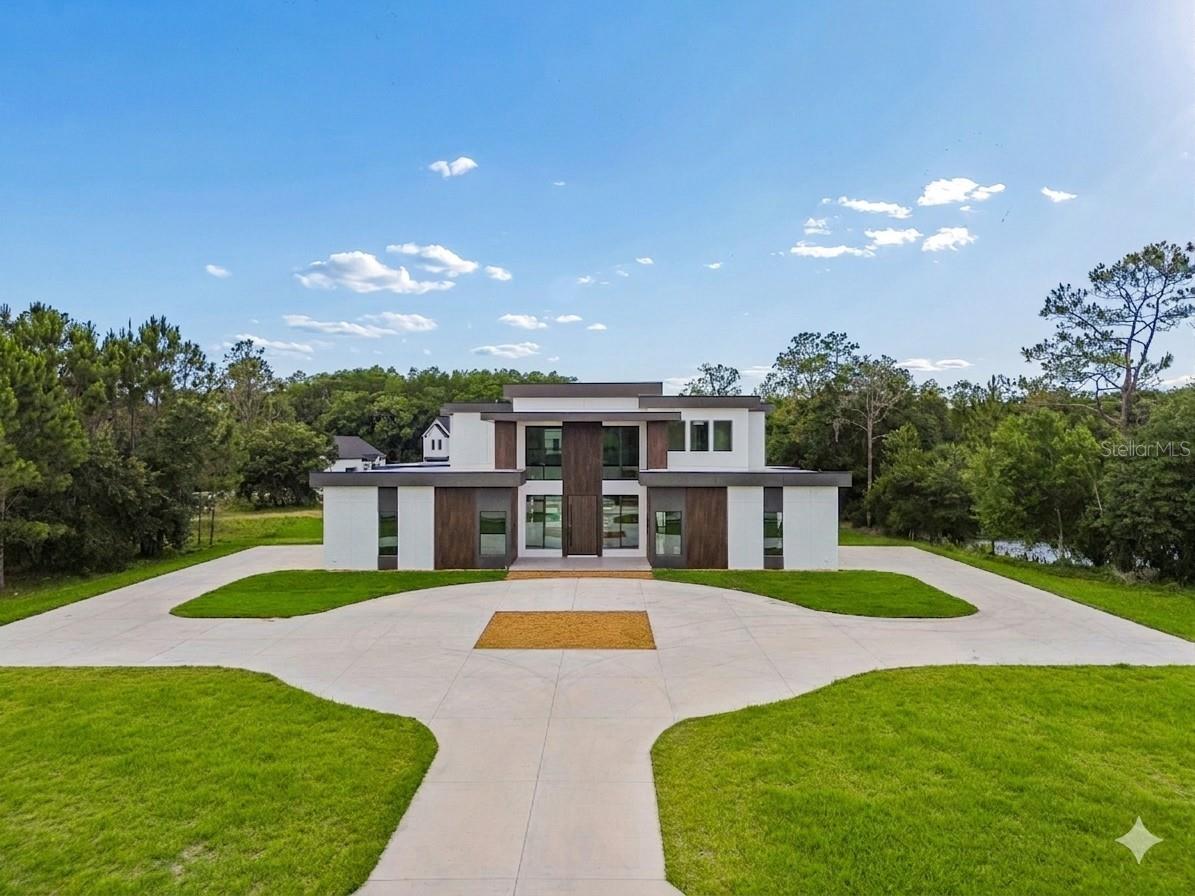 Located in the highly desirable East Lake area of Tarpon Springs, this custom new construction contemporary estate sits on a sprawling 2.5-acre lot within the exclusive gated Keystone Palms community. Backing to a private wetland conservation area, this architectural masterpiece blends a striking modern geometric design with luxury high-end finishes. The expansive floor plan features 4,928 square feet of heated living space and over 7,000 square feet under roof, anchored by a grand foyer and a soaring 2-story great room centered around a stunning feature wall and a sleek gas fireplace. True to its vision as an entertainer's dream, a spectacular floating staircase serves as a architectural focal point, ascending elegantly to the second level. Premium large-format porcelain tile runs seamlessly throughout the main living areas, which are beautifully illuminated by curated designer lighting fixtures. The gourmet chef's kitchen is equipped with professional-grade appliances, an oversized center island, and a walk-in pantry, transitioning effortlessly to the dining space and out to a large covered lanai. Upstairs, the elegant catwalk bridge overlooks the lower level, leading to an open and versatile loft space alongside a sophisticated upstairs bar area perfect for evening refreshments. This level hosts three generously sized guest rooms, two with large walk-in closets, providing ultimate comfort and privacy for family and visitors alike. French doors open from the second story to a wide upper covered deck patio that offers an elevated vantage point of the beautiful surroundings. Down below, this private oasis is encompassed by a spectacular double-story screened lanai that houses a heated saltwater pool and spa, a sunken firepit, a dedicated pool bath, and a cabana with a fully equipped outdoor kitchen. Zoned for top-rated schools, this exceptional Keystone Palms estate delivers the ultimate in privacy, security, and modern luxury.