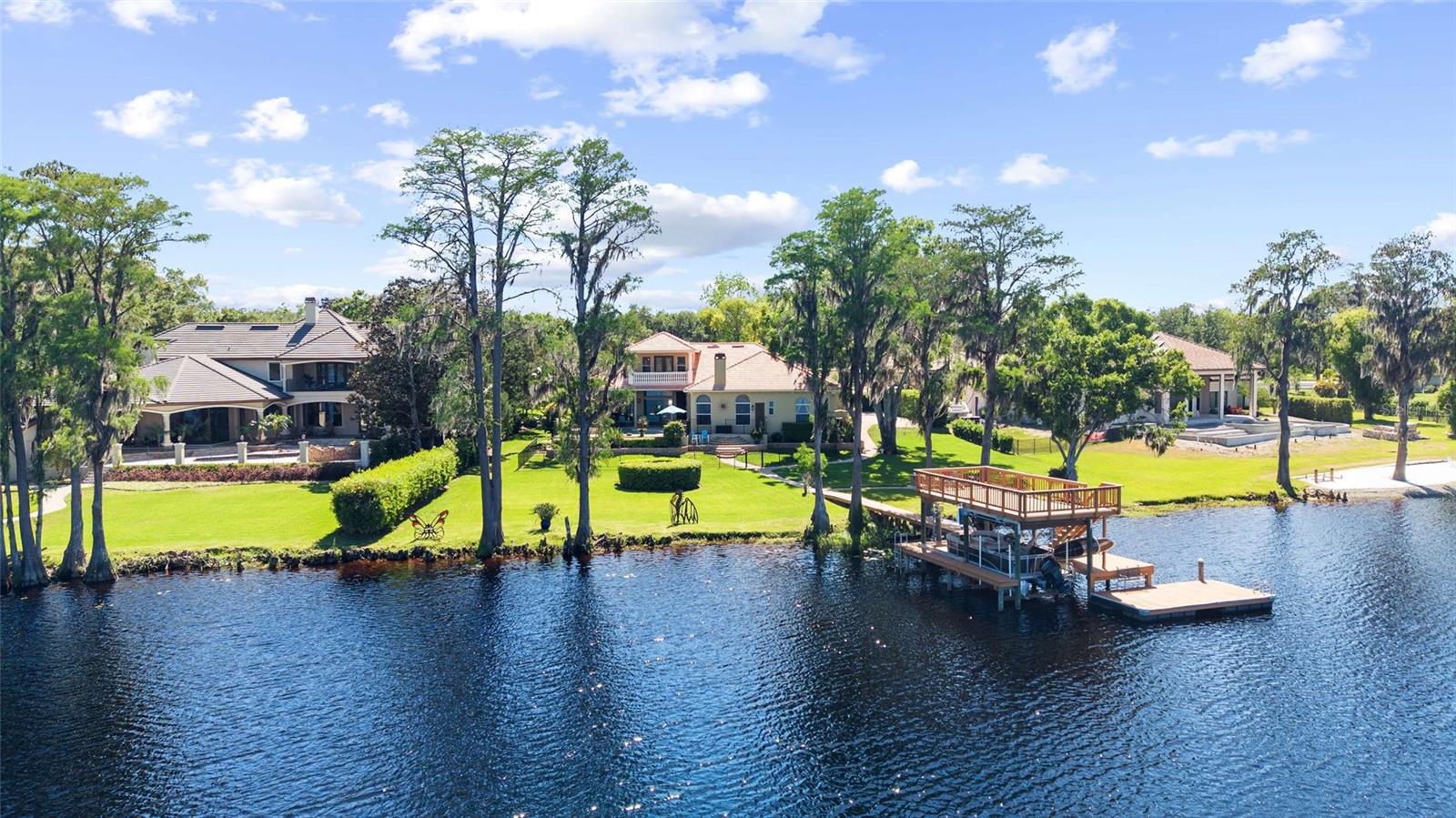 Under contract-accepting backup offers. Tucked away within the gated community of Northbridge at Lake Pretty, this exceptional lakefront estate is one of only six homes situated directly on exclusive Lake Pretty—a pristine 100-acre ski lake in the heart of Odessa. Offering over 4,300 square feet, this 4-bedroom, 4.5-bathroom residence also features a dedicated office and expansive bonus/theater room, with every bedroom enjoying its own private ensuite. From the moment you enter, you’re welcomed by abundant natural light and a stunning formal living space highlighted by a large bay window that perfectly frames the home’s most captivating feature—the breathtaking lake views. Just off the formal living area, the private right wing of the home includes a dedicated office, powder room, and an expansive primary suite retreat. The primary bedroom features double tray ceilings with crown molding, French doors leading to the outdoor patio, and two custom walk-in closets with built-ins. The en-suite bathroom is thoughtfully designed with dual vanities, a large enclosed shower, and a relaxing jetted tub. The kitchen serves as the centerpiece of the home, beautifully appointed with high-end granite countertops, two-toned cabinetry, and a large center island with farmhouse sink. Premium appliances include a Viking refrigerator, Viking 6-burner gas range, Bosch dishwasher, built-in GE double ovens and microwave, along with a hidden pull-out coffee bar for added functionality. A butler’s pantry passthrough with a wine refrigerator and additional storage elevates both convenience and entertaining. The kitchen seamlessly flows into the family room and dining nook, where oversized windows flood the space with natural light and showcase serene water views. A private wing off the main living area includes two bedrooms and a versatile bonus room, currently designed as a theater but easily adaptable as a game room, fitness space, or golf simulator. Bedroom two features a spacious ensuite with a separate makeup vanity and large walk-in closet, while bedroom three offers beautiful lake views and an ensuite bath that also functions as a pool bath. Upstairs, a private retreat awaits with an additional bedroom featuring its own ensuite, walk-in closet, and double doors leading to a balcony overlooking the pool and expansive lake views—an ideal space for guests or multigenerational living. Designed for true indoor-outdoor living, the backyard is a showstopper. Enjoy a covered lanai with a fully equipped outdoor kitchen including a grill, vent hood, mini refrigerator, ice maker, and bar seating. The saltwater pool and spa with spillover feature create a resort-style setting, while paver pathways lead down to a custom lakeside fire pit nestled among mature cypress trees. The private two-story dock is built for both recreation and entertaining, complete with a boat lift accommodating up to 10,000 pounds, dual jet ski lifts, and an upper-level deck offering panoramic views of the entire lake. This is a rare opportunity to own one of the most coveted lakefront properties in Odessa, combining luxury, privacy, and true waterfront living.