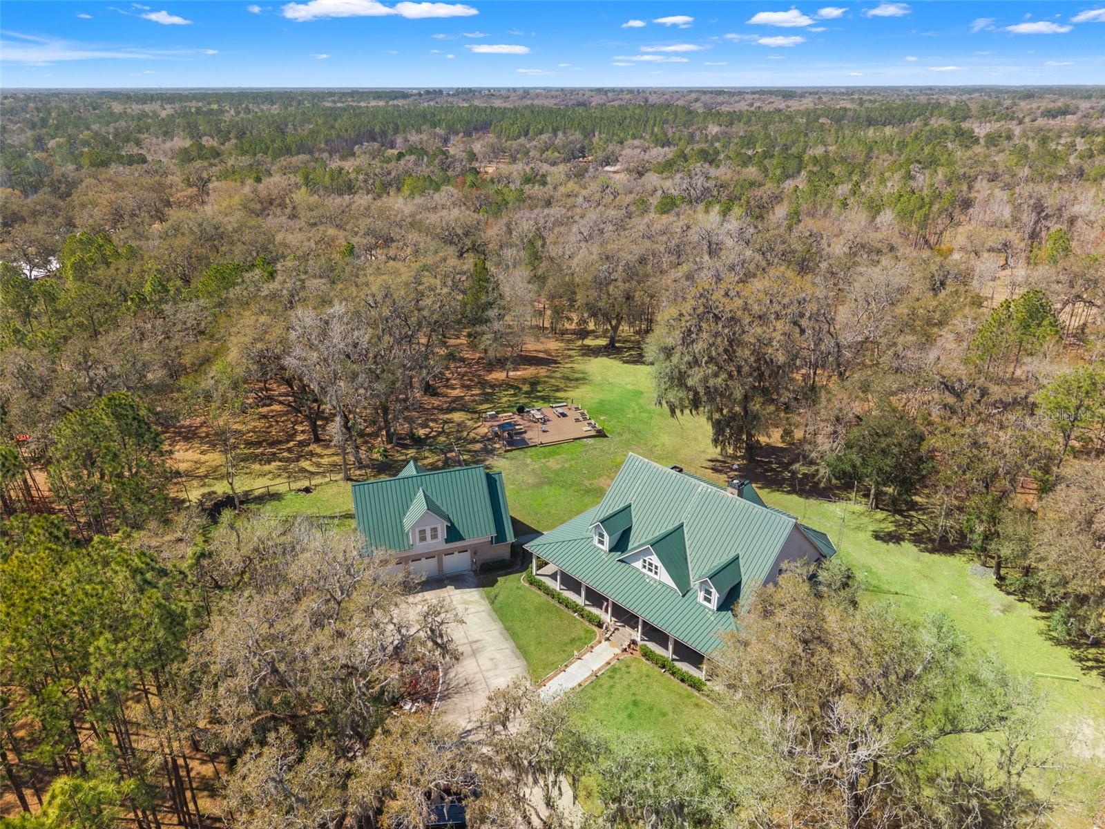 MASSIVE IMPROVEMENTS TO THE ASSET WITHOUT A PRICE INCREASE! Welcome to 105 acres of rolling Florida countryside transformed into a premier equestrian estate—a rare property where professional horse facilities, natural beauty, and luxury ranch living come together on an exceptional scale. Set among towering grandfather oaks and planted pines, open pastureland, and miles of private riding trails, this property has been thoughtfully developed into a fully operational equestrian facility designed for serious horse programs, trainers, and passionate riders alike.  The equestrian infrastructure is both extensive and refined. The remodeled main barn features oversized 12’ x 24’ stalls, wash bays, feed and tack rooms, and functional space designed for efficient daily operations. Expanding the facility is a new 14-stall European-style center aisle barn, creating additional capacity for boarding, training, or breeding programs while maintaining the elegance expected of a premier horse property.  At the center of the riding program is a 150’ x 250’ professional riding arena, providing an ideal environment for training, schooling, and competition preparation.
The land itself has been carefully developed for equestrian use, with 17 rotational pastures, newly installed fencing across the property, cleared grazing areas, and improved paddock systems designed to support both horse health and operational efficiency.
A VIP barn and rider lounge is currently under construction, positioned privately with sweeping views over the arena. Once completed, this space will become the social and operational heart of the facility—featuring a client lounge, bathrooms, VIP bar, office space, and tack room, creating a premium experience for riders, trainers, and guests.  Beyond the barns and arenas, the property offers a lifestyle rarely found in modern ranch properties. Miles of riding trails wind through planted pines and open fields, while a private five-acre stocked lake with dock and picnic area provides a peaceful retreat after a day in the saddle. A private shooting range adds another dimension of outdoor recreation.
Anchoring the estate is a beautifully remodeled brick residence offering over 4,600 square feet of refined living space. The four-bedroom, four-bath home blends modern upgrades with classic ranch charm, highlighted by a sweeping wraparound porch overlooking the rolling landscape of the ranch.  Inside, expansive gathering areas create the perfect setting for entertaining or relaxed country living, while three of the four bedrooms feature private en-suite baths, providing comfort and privacy for family and guests.
Above the oversized garage, the loft is currently being converted into a full two-bedroom, one-bath apartment, ideal for staff housing, guest accommodations, or additional income potential.  With significant infrastructure already completed and continued improvements underway, this 105-acre estate represents far more than a private ranch. It is a growing equestrian compound designed for lifestyle, training, and long-term opportunity—a place where the passion for horses meets the refinement of luxury country living.