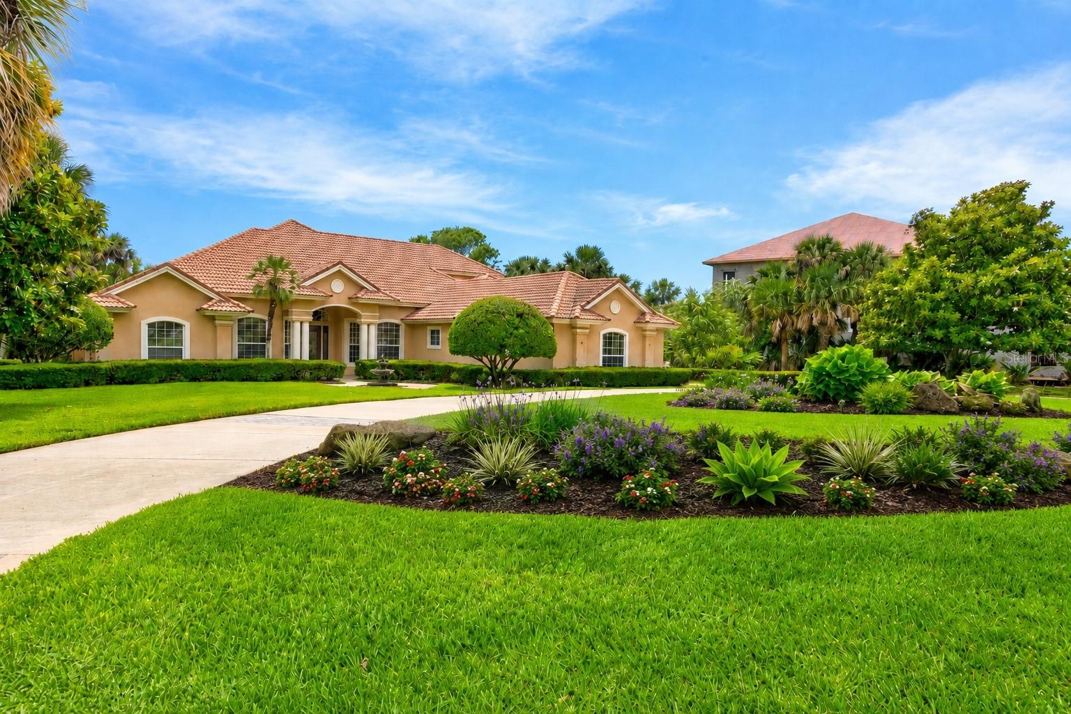 One or more photo(s) has been virtually staged. Set within the private island enclave of Island Estates at Hammock Dunes, this custom Machin Design Builders waterfront estate delivers the scale, privacy, boating access, and coastal presence buyers hope to find but rarely see in one complete property. Positioned on more than an acre along Fox Cut, the home offers direct boating access to the Intracoastal Waterway, Matanzas River, and beyond to the Atlantic, with a covered boathouse, covered lift, seawall, dock, and floating jet ski dock already in place. The main residence offers more than 4,100 sq. ft. of heated living space, a flexible floor plan designed for everyday comfort, extended guests, entertaining, and multi-generational living. The layout functions as a spacious 6-bedroom main home with multiple suite-style options, including two primary-style retreats, while a detached guest/in-law suite with private entry, kitchenette features, and bathroom access creates a rare opportunity for visiting family, live-in help, a private office, fitness studio, or separate guest quarters. From the circular drive, Spanish tile roof, mature landscaping, and estate-level curb appeal to the warm interior spaces, the property feels substantial without losing its sense of comfort. Recent improvements give the home a fresh, polished feel, including all-new ductwork, professional interior paint throughout, and an updated kitchen with quartz counters carried up the backsplash, stainless appliances, center island, built-in cooking features, beverage refrigeration, and a walk-in pantry. The heart of the home opens naturally from the kitchen and breakfast area toward the living spaces and pool, creating the flow that makes casual mornings, waterfront weekends, and large gatherings feel effortless. A main living room with gas fireplace, built-ins, speakers, and crown molding anchors the home, while a separate family room/den, formal dining room with statement lighting, and private office with built-ins allow the home to adapt to real life. The downstairs primary suite offers tray ceilings, crown molding, poolside connection, dual walk-in closets, walk-in shower, and jetted tub. Upstairs, the second oversized primary-style suite adds flexibility with its own bath, walk-in closet, and large private balcony, while additional bedrooms throughout the home provide rare space for guests, hobbies, work, or long-term living needs. Outside, the screened pool and spa area becomes the natural gathering place, with waterfall detail, tile accents, covered outdoor living, porch fans and lighting, outdoor shower, pool bath access, and a summer kitchen with grill and sink. The climate-controlled four-car garage is a major advantage, offering nearly 40 feet of width, two double garage doors, and room for vehicles, tools, fishing gear, golf carts, and coastal toys. With public utilities, underground utilities, propane, recycled irrigation, mature landscaping, and Flood Zone X positioning, the property balances luxury appeal with practical peace of mind. Island Estates is one of Flagler County’s premier private coastal settings, offering staffed gated access, private beach access, waterfront living, and optional Hammock Dunes Club membership with golf, dining, fitness, racquet sports, croquet, bocce, pool amenities, and social activities. For buyers seeking a true coastal estate with room to live, host, boat, relax, and entertain, 67 Island Estates Parkway delivers the complete Hammock Dunes lifestyle.