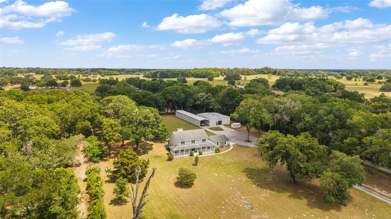COMMERCIAL/AGRICULTURAL OPPORTUNITY. Situated on 10 private acres in Summerfield, just minutes from The Villages, this exceptional gated estate offers the perfect blend of luxury living, multi-generational flexibility, and equestrian-ready acreage. A long, paved driveway welcomes you into a true family compound designed for those seeking space, privacy, and versatility for both lifestyle and business needs. For car enthusiasts, business owners, or hobbyists, the property is equipped with a 10+ car garage capacity and multiple outbuildings. The impressive 1600+/- square foot of AC space in the workshop and total 4600+ square foot enclosed steel building includes a fully insulated expansion, offering enhanced usability along with three dedicated office spaces—ideal for running a business from home, storing equipment, or creating a private studio environment. Additional features include RV and boat storage, roll-up access, and covered parking.

The residence has been thoughtfully enhanced with the addition of a primary suite on the first floor, providing convenience and privacy with a beautifully appointed ensuite bath. Several bathrooms throughout the home have been recently updated with elegant marble tile finishes, elevating the overall design with a refined, modern touch.

Inside, the home features 4 bedrooms, 3 full baths, and a half bath, highlighted by a grand foyer, soaring two-story ceilings, and a spacious living area centered around a wood-burning fireplace. The gourmet kitchen is designed to impress with high-end appliances, a large center island, and both casual and formal dining spaces, making it ideal for entertaining and everyday living. A bonus room on the main level offers flexibility for a den, office, or media space.

Upstairs, additional bedrooms and living areas provide separation and comfort for guests or family, while the original loft-style primary retreat remains a unique feature with expansive closet space and a spa-like bath.

Outdoor living is equally impressive, with a wraparound porch overlooking the expansive grounds, mature landscaping, paver walkways, and multiple storage structures. The property is well-equipped with extensive parking, security lighting, and functional infrastructure to support a variety of uses, including equestrian pursuits—bring your horses and enjoy the open acreage.

Additional highlights include Andersen double-pane windows, crown molding, wood and tile flooring, a detached two-car garage with epoxy floors, an oversized laundry room, and additional flex spaces including a “she-shed.” The property is also offered with a home warranty and termite bond for added peace of mind.

Located within close proximity to shopping, dining, medical facilities, and entertainment, while still offering the privacy of acreage living, this is a rare opportunity to own a versatile estate in one of Central Florida’s most desirable and growing areas.