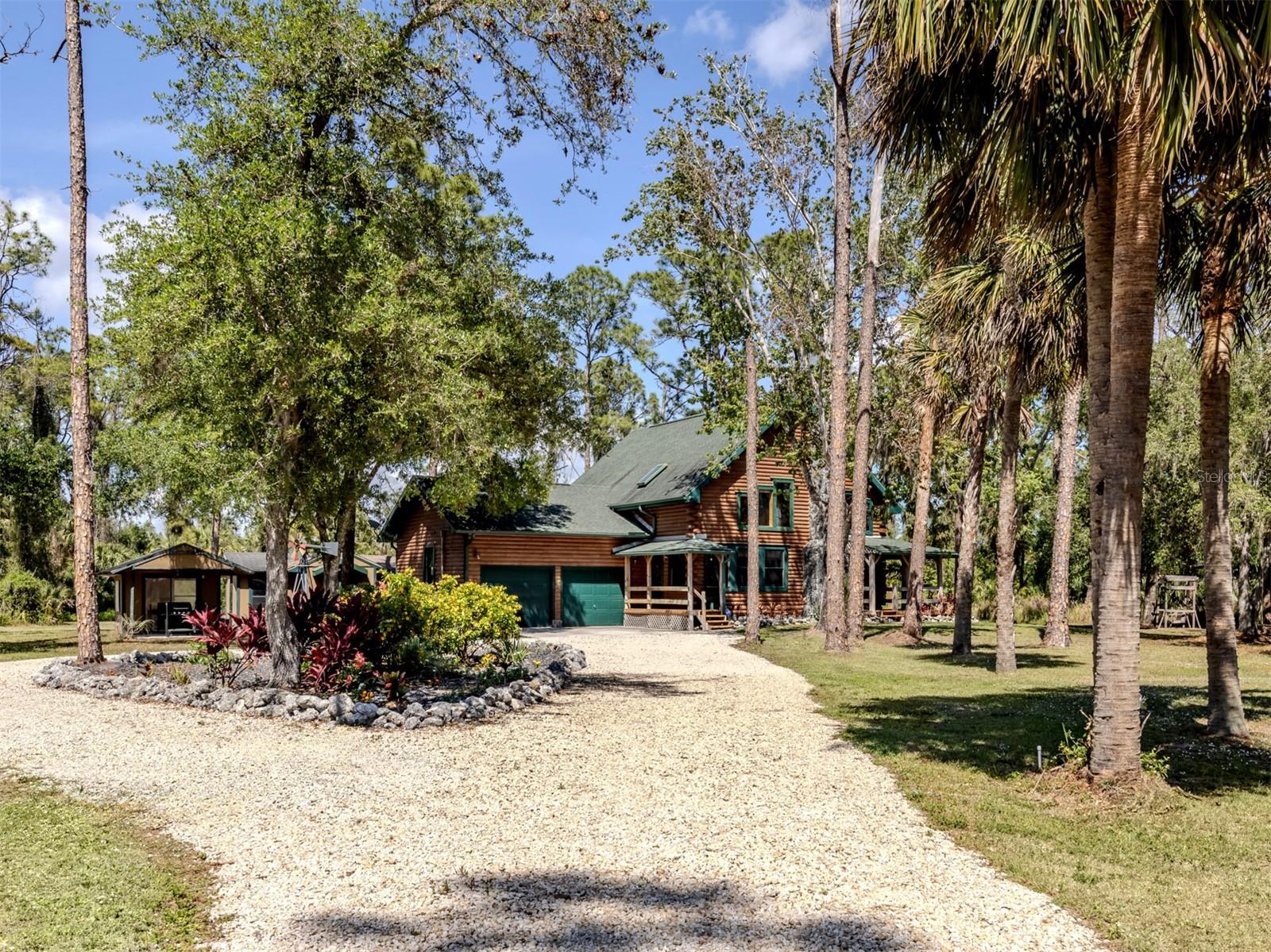 Tucked away on more than three acres of natural Florida landscape, this custom-built log home delivers the charm of a rustic retreat with the comfort of modern living. From the moment you arrive, the warm cabin aesthetic sets a welcoming tone, while inside, contemporary updates and gleaming newer appliances make everyday life effortless. The open kitchen, dining, and great room flow together beneath soaring two-story ceilings, anchored by an impressive stone wood-burning fireplace. A beautiful knotty-pine staircase leads to a spacious 22×13 loft, illuminated by a skylight and framed by rich wood-clad ceilings. The home offers two generously sized bedrooms and baths, one conveniently located on the main level and the other upstairs.
Step outside to expansive wood decking that extends your living space and creates the perfect backdrop for relaxing or entertaining. Two detached buildings provide excellent flexibility for storage, workshop space, or hobby use. While the area immediately surrounding the home feels like a large, cheerful yard, the remainder of the acreage is filled with native Florida foliage, creating a natural privacy buffer on three sides.