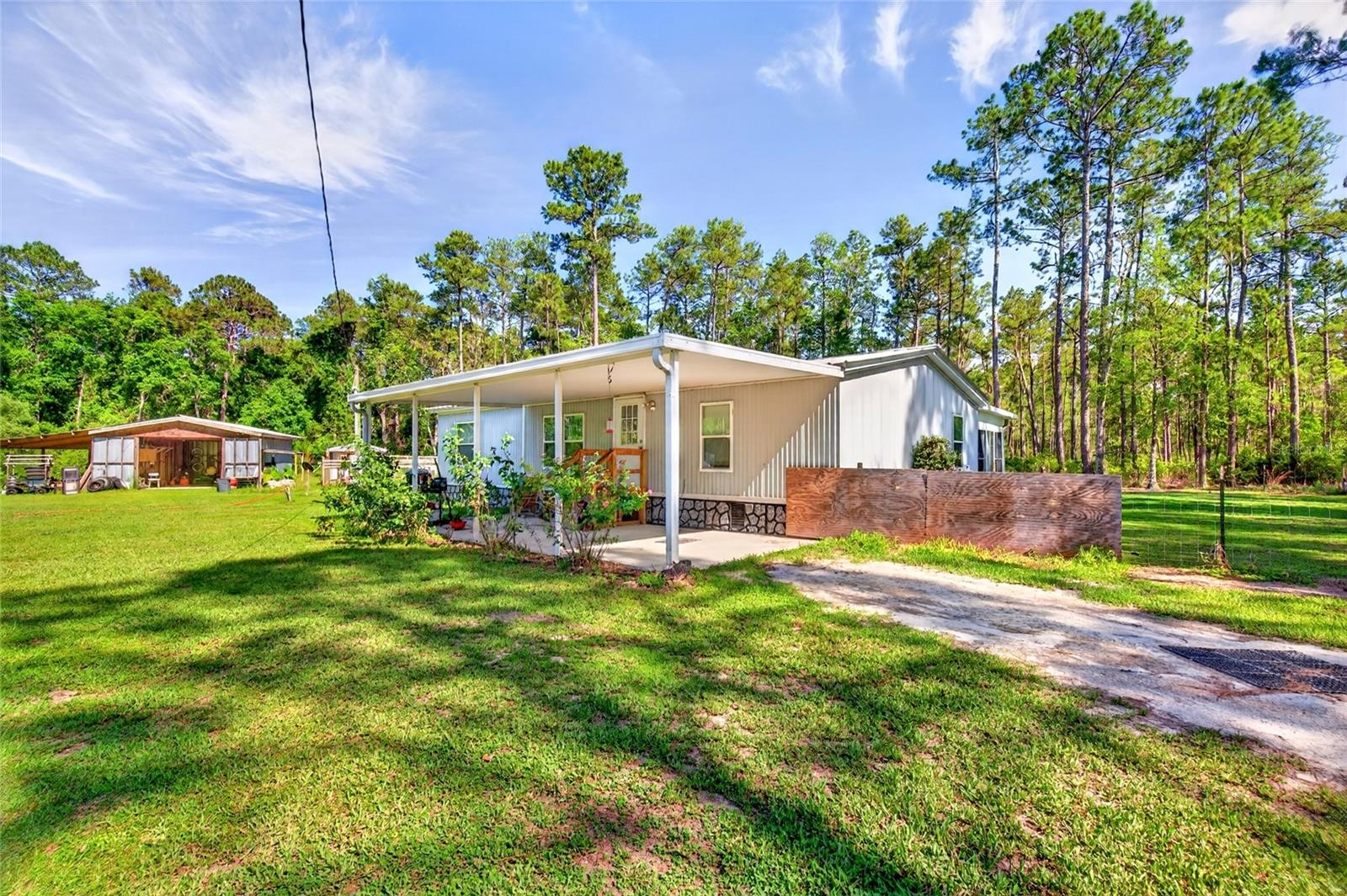 Virtually Staged. Escape to your own private retreat with nearly 4 acres of secluded Florida countryside! Nestled on 3.97 peaceful acres with no HOA, this 4 bedroom, 2 bathroom manufactured home offers the perfect blend of privacy, functionality, and outdoor lifestyle. Surrounded by mature trees and tucked away from the hustle and bustle, this property creates a true sense of seclusion while still offering the conveniences of everyday living. Inside, the 1,648 square foot home features a spacious and functional layout with an open living and dining area, abundant natural light, and generously sized bedrooms to accommodate family, guests, hobbies, or a home office. The kitchen offers plentiful cabinet and counter space, making meal prep and entertaining easy, while the oversized enclosed Florida room provides additional flexible living space with beautiful views of the property. Step outside and discover what truly makes this property special. The expansive acreage provides room to roam, ride, store equipment, or simply enjoy the peace and quiet of country living. A large storage barn/workshop offers excellent space for tools, projects, equipment, recreational vehicles, or outdoor gear. For the outdoor enthusiast, this property is packed with opportunity, featuring a private shooting range and a secluded setting ideal for enjoying nature right in your own backyard. Whether you're looking for space to spread out, room for hobbies and recreation, or simply a quiet property away from neighbors, this one checks all the boxes. Properties offering this much privacy, usable acreage, and functionality are hard to find — schedule your private showing today!