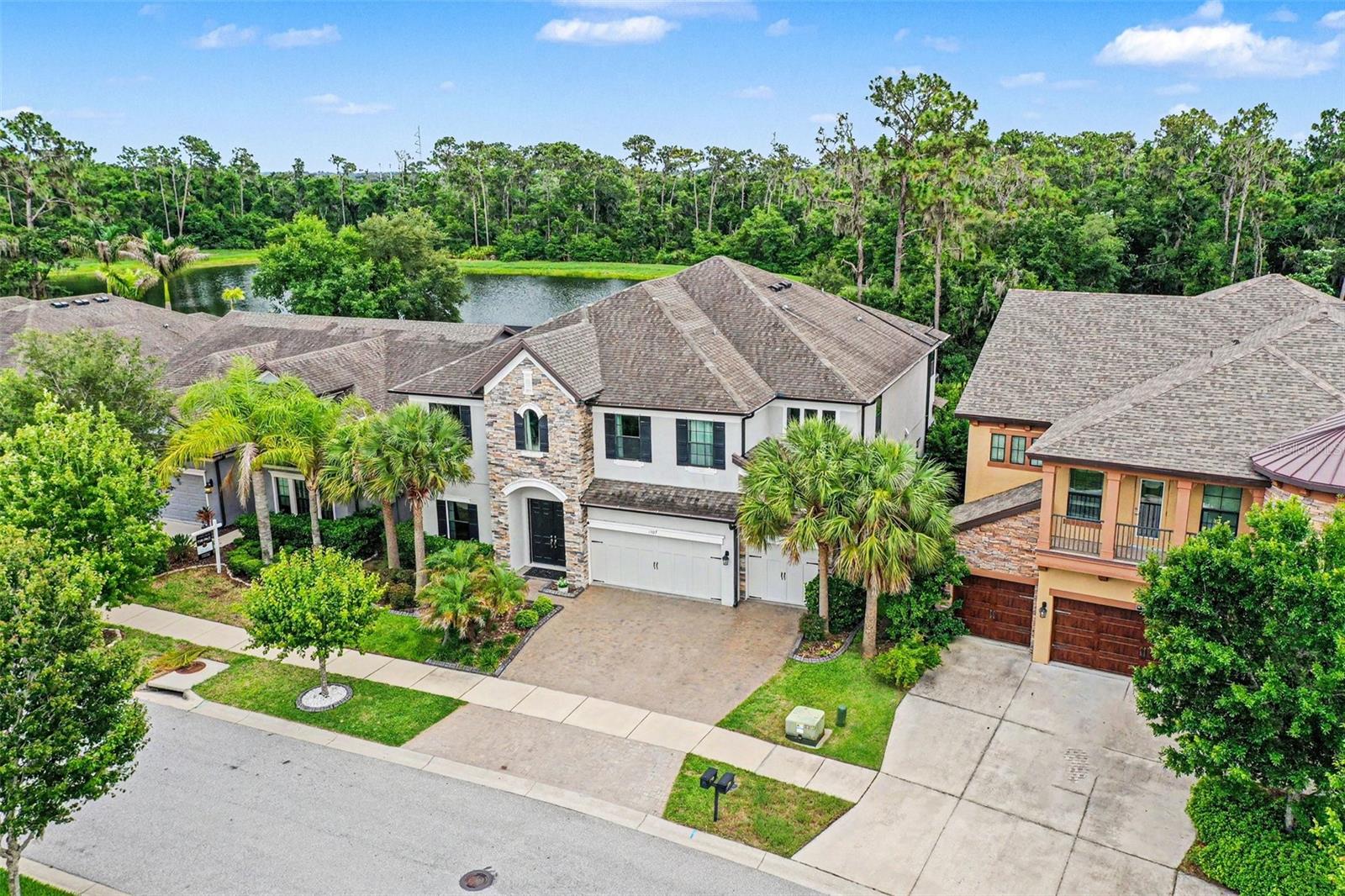 Located in a private, gated executive enclave, this stunning 5-bedroom, 5-bathroom estate offers a rare and highly desirable layout featuring two complete primary suites and a dedicated home office. Backing up to a lush nature preserve and two peaceful ponds, this private sanctuary features a 3-car garage and a spectacular, solar-heated pool with three cascading waterfalls. Inside, the open floor plan flows seamlessly from the formal dining room and a private office behind French doors into a light-filled family room with four large sliding doors. The adjacent chef's kitchen is a masterpiece, boasting quartz countertops, an oversized island, a massive walk-in pantry, high end cabinetry, and premium stainless steel appliances including a cooktop, wall-mount hood, and a built-in oven. Rare and highly desirable, this home features two complete primary suites: one on the main floor with a private bath and garden tub, and a grand executive suite upstairs with a Jacuzzi tub, a massive walk-in shower, and a private balcony overlooking the pristine preservation views. The second level also hosts three additional bedrooms, two full baths, a convenient laundry room, and a massive bonus/TV room with a separate loft area. Perfect for entertaining, the outdoor oasis includes a covered lanai and a fully equipped summer kitchen with a built-in grill, side burner, and sink. Exceptional upgrades like four 72-inch ceiling fans, whole-house gutters, exterior security cameras, and quartz or granite in every bathroom complete this masterpiece. Residents enjoy South Fork’s resort-style amenities—including a community pool, sports courts, and walking trails—along with an effortless commute to Tampa via I-75, the Selmon Expressway, and US-301