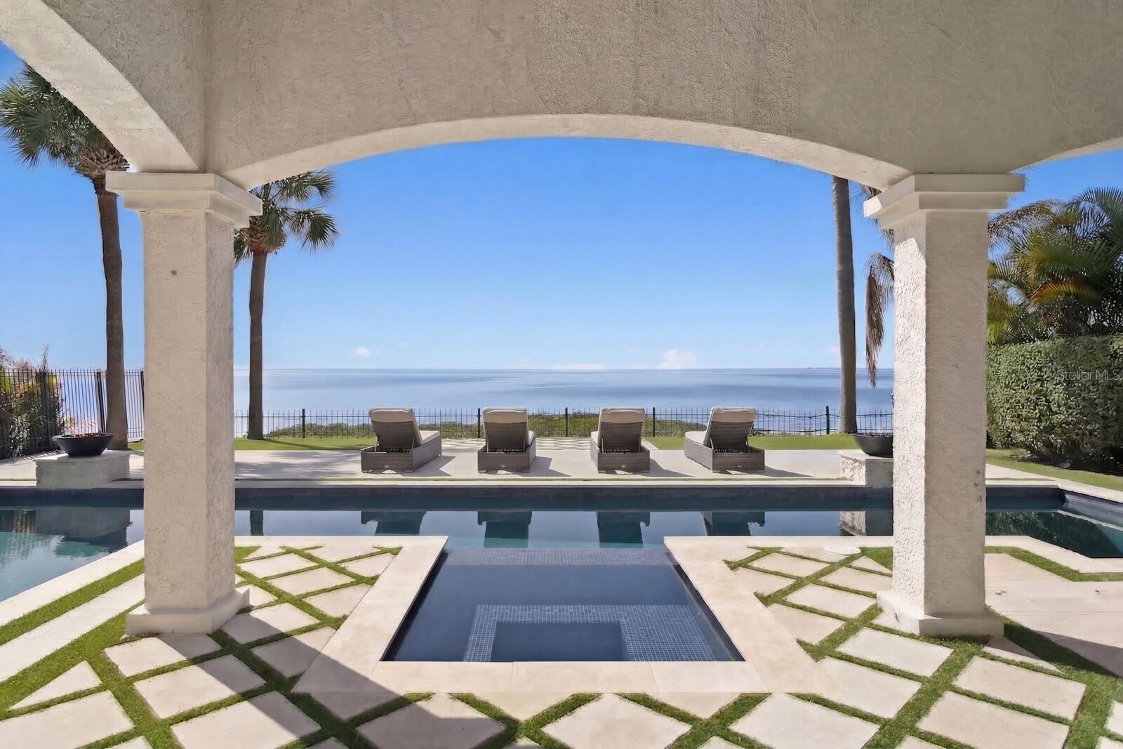 Positioned among Tampa Bay’s BEST VALUES for open-bay luxury waterfront living. Masterfully renovated Mediterranean waterfront home in the gated community of Bridgeview Estates overlooking Tampa Bay. Featuring wide open bay views, 5,175 square feet of living space, and extensive designer-curated upgrades. Embrace a refined waterfront lifestyle on the bay with a boat slip/lift and resort-style outdoor living. A circular paver driveway leads to a covered entry framed by arched architectural details, illuminated by gas lanterns and featuring an imported handcrafted carved wood door. Inside, a dramatic two-story foyer boasts a sweeping staircase, custom iron balusters, and statement chandelier. Wide-plank hardwood flooring, coffered ceilings, custom lighting, wood beam accents and elevated ceilings carry throughout the home. The main living area has been reimagined with an open-concept design, anchored by a fireplace feature wall and expansive glass doors that frame water views and provide seamless access to the covered lanai. A dedicated lounge with custom bar features a fireplace, a waterfall-edge stone island, custom cabinetry, and mirrored accent walls with integrated shelving. Additional first-floor living spaces include a wainscoted game room with an adjacent study or dining room, offering flexibility for everyday living. The kitchen includes quartz countertops, Sub-Zero, Thermador, and Wolf appliances, a 6-burner gas range, wine refrigeration, a wine storage feature wall, and a dining area positioned to capture natural light and waterfront views. The first level also features a guest suite, laundry room, and a pool bath with convenient exterior access. Outdoor living is designed to maximize your waterfront lifestyle with a heated saltwater pool and spa, outdoor kitchen, pergola, custom geometric turf and paver inlay, along with multiple lounging areas. A covered lanai with wood ceiling and a gas firepit lounge creates inviting space for entertaining. Enjoy access to a common dock, with a private low-profile boat lift equipped with electric and water service. The second level includes a primary suite with fireplace, waterfront balcony, and dual walk-in closets. The primary bath features a soaking tub and glass-enclosed shower. An adjacent sitting area offers flexible living space and balcony access. Four additional bedrooms include two ensuite baths. A bonus room is positioned alongside one of the ensuite bedrooms, offering a flexible option for extended guests or a private suite-style living arrangement. Modern refinements complement the home’s architectural character, including custom interior arched doors and Spanish tile accents. Recent updates include PGT impact-rated doors, a whole-home generator, EV charger, mechanical systems, and integrated audio/visual and security features. Enjoy the amenities of waterfront living, stunning views and sunsets in this exclusive South Tampa gated community offering fishing and kayaking opportunities nearby, with access to a sandy beach area along the shoreline. Seller reports home did not experience flooding during storms due to its higher ground elevation. Buyer to verify.
