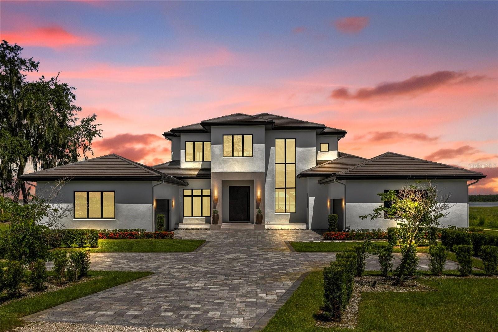 One or more photo(s) has been virtually staged. Do not miss this hidden gem of Lake Nona on stunning Lake Hart and one of the last rural settlements in this progressive area. You will be welcomed by ancient oak trees and a rustic gravel driveway which takes you to a modern masterpiece created by Valdara Homes. You will be in awe by the stillness and sounds of nature despite being two miles away from local shopping, restaurants, schools, and minutes away from the USTA, Lake Nona Medical City and A rated schools. This 2022 Parade of Homes winner has large windows built on a modern Balinese design and zen culture. Behind a grand pivoting door lies  20-foot ceilings, wood accents, clay painted accent walls and large hurricane proof glass sliders which frame a stunning view of Lake Hart. The abundance of natural light will give you a feeling of being connected to the nature that surrounds you. The kitchen is equipped with Sub Zero appliances and custom-made cabinetry. Key features include a professional Wolf gas range and griddle, custom concrete countertops and a hidden pantry. The open floor plan provides a seamless flow to the outdoor kitchen with a built-in grill and a Sonos system throughout. Enjoy the saltwater pool or relax in the gas heated spa with a 140 ft lake view. The master bedroom design has unobstructed views of the lake, staggered tray ceiling, dark wooden floor and automated blackout curtains. It hosts a custom-built vanity housed in custom concrete and custom-made wooden cabinetry with accent lighting. A stunning dual facing gas fireplace with water vapor provides a real fire effect creating a soothing ambiance. His and her custom walk-in wardrobes and separate custom-built wooden storage cabinetry finish off this grand master bathroom. The downstairs guest room features a custom-built wardrobe, large bathroom, dark wooden flooring, and its own entrance. The floating staircase, which is more of a piece of art, transports you upstairs to a large loft with large windows providing you with a bird’s eye view of the beautiful Lake Hart. Two large bedrooms include one with a custom-built wardrobe and the other a walk-in wardrobe, a private bathroom, and a jack and jill bathroom connected to a bonus room designed to be converted to a third bedroom if needed. The many hidden details have led to it’s Florida Green Building Coalition Platinum certification. A Building Biologist provided input from the ground up on how to create a home that enhances the health of the occupants. The home is painted with low VOC paint and has technology to ensure the highest level of indoor air quality. The home is fed by its own well, filtered by whole home filtration as well as a point of use filtration system ensuring the cleanest water. It is hard wired with ethernet capability to accompany the Wi-Fi. Bedrooms are uniquely wired so that no electrical wires run behind headboards to interfere with a restful sleep. The master bedroom and downstairs bedroom have kill switches to cut off all electricity to the room providing an electrically free sleeping environment. Outside, you will find lush landscape fed by well water to utilize natural resources. A separate 2000sqf building with its own kitchenette can serve as an office, a gym space, a den, or a guest home. This space would make a great source of income through short- or long-term tenancy. A full-size tennis court, paved driveway finish this spectacular estate which is secured with security cameras and a monitored alarm system.