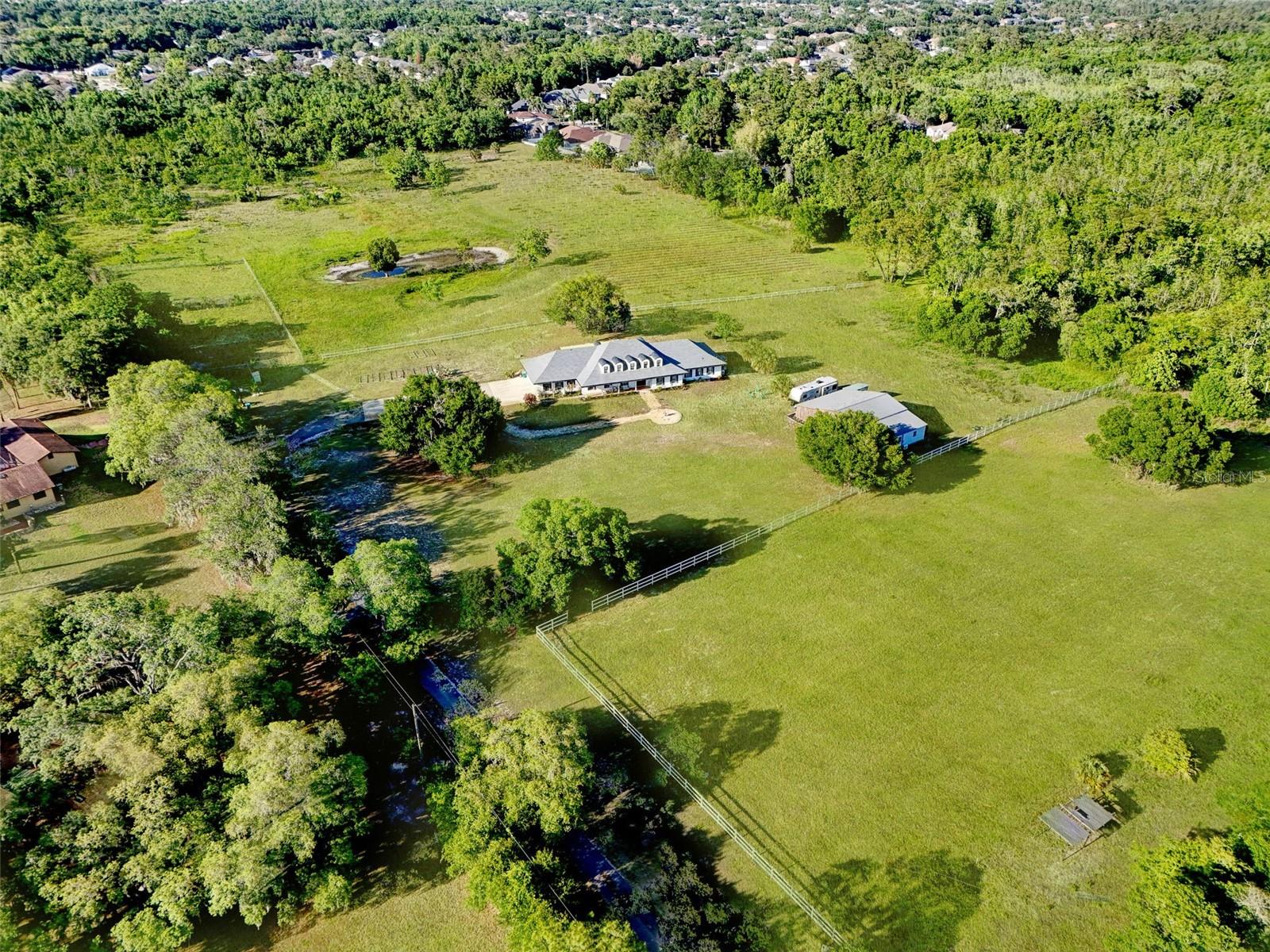 One or more photo(s) has been virtually staged. Welcome to Oak Hollow Manor, a rare 20-acre gated equestrian estate and private family compound tucked into one of Oviedo’s most desirable acreage corridors. Set deep within the property and surrounded by mature trees, open pasture, and high-and-dry usable land, this Southern ranch-style estate offers a unique combination of privacy, flexibility, and lifestyle opportunity just minutes from Oviedo, Winter Park, UCF, and Central Florida’s major conveniences.
Built in 1985, the main residence features 6 large traditional bedrooms, 4.5 bathrooms, two large bonus rooms (that can be bedrooms as well), and approximately 5,737 square feet of living space designed for comfortable estate living, multigenerational households, entertaining, working from home, or simply enjoying room to spread out. The downstairs primary suite includes a spacious bedroom, sitting area, and his-and-her closets, while the flexible floor plan also allows for a potential second downstairs primary-style suite with direct access to a full bathroom.
Warm and inviting living spaces, generous room sizes, and timeless Southern estate character create a welcoming atmosphere while still offering the next owner opportunities to personalize and modernize to their taste.
The land itself is one of the property’s most exceptional features. With approximately 5 fully fenced acres currently dedicated to horse grazing, A-1 zoning, and wide-open usable acreage, the property is ideally suited for equestrian enthusiasts, boutique farm operations, hobby farmers, bonfire gatherings, agricultural use, or buyers seeking long-term land value, privacy, and lifestyle flexibility in a highly sought-after Central Florida location.
Major recent improvements provide additional value and peace of mind, including a new roof installed in 2022, a permitted 2,500+ square-foot metal barn with electric completed in 2022, and a newly constructed resort-style saltwater in-ground pool completed in 2026 and luxury vinyl plank flooring installed in 2025. Other recent improvements completed between 2022 - 2024 are kitchen updates, bathroom updates, interior and exterior paint, lighting and fixtures. The barn offers exceptional flexibility as an equestrian barn, workshop, hobby space, equipment storage building, or future entertainment pavilion. Two additional storage buildings provide even more utility and functionality.
Out back, the newly completed pool creates a peaceful private retreat overlooking scenic acreage and mature natural surroundings, offering the feel of a secluded countryside estate while remaining close to everyday conveniences. Despite its private setting, the property is surrounded by established and desirable communities, including neighboring Aloma Woods.
Additional features include three HVAC systems, with two replaced in 2021, no HOA, and zoning for top-rated Seminole County schools including Evans Elementary, Tuskawilla Middle, and Lake Howell High School. Trinity Prep is located just minutes away.
With 20 acres and A-1 zoning, the property may also offer future flexibility for additional accessory structures or a potential accessory dwelling unit up to approximately 1,000 square feet, subject to Seminole County approval, permitting requirements, setbacks, and buyer verification.