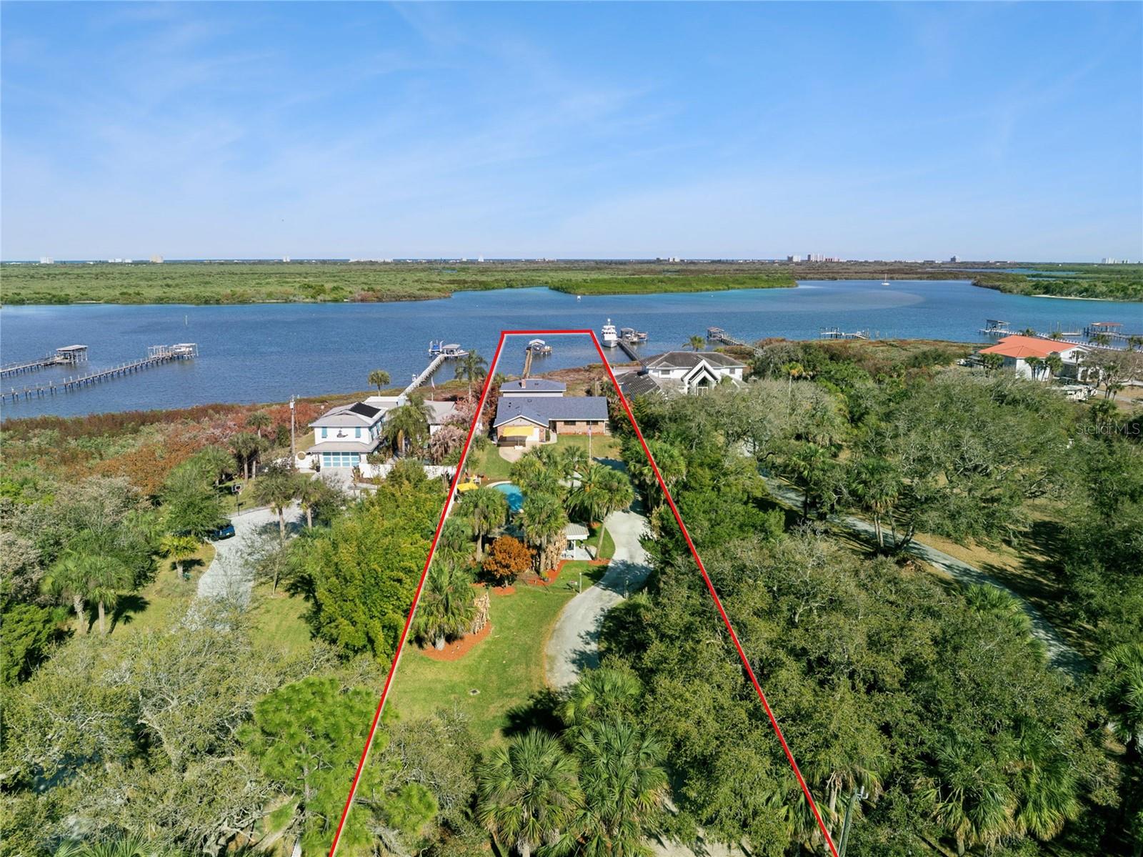 Welcome to 1703 S Riverside Drive—an exceptionally rare ±1.1-acre waterfront estate offering ±80 feet of direct deep-water Intracoastal frontage in the heart of New Smyrna Beach. Perfectly positioned along prestigious Riverside Drive, this extraordinary property presents a unique opportunity to either build your custom waterfront dream estate or enjoy the beautifully maintained existing 5-bedroom, 3.5-bath pool home—both options delivering an unmatched coastal lifestyle on over an acre of prime waterfront land. With deep-water Intracoastal access, the property easily accommodates larger boats or yachts right in your backyard, providing unparalleled boating convenience. To the east, panoramic sunrise views stretch across a protected mangrove conservation area, ensuring permanent natural beauty and privacy that will never be developed. The existing residence captures timeless coastal charm, featuring expansive windows that fill the home with natural light and framed stunning water views from the moment you step inside. The open kitchen and living area create an inviting space for gathering, highlighted by a wood-burning fireplace and a well-appointed kitchen with granite countertops, stainless steel appliances (gas), and abundant prep and entertaining space. The first-floor primary suite offers breathtaking waterfront views along with a spacious primary bath, creating a peaceful retreat within the home. Outdoor living is equally impressive, with a heated saltwater pool and spa, a covered boat dock with lift, and a generous waterfront deck—perfect for enjoying morning sunrises and watching dolphins and native wildlife glide through the Intracoastal. Ideally located just minutes from the Canal Street Historic District and Flagler Avenue, you’ll enjoy easy access to New Smyrna Beach’s beautiful beaches, renowned dining, boutique shopping, and vibrant entertainment—just a short golf cart ride away.  Opportunities like this are exceptionally rare. Properties offering more than an acre with deep-water Intracoastal access in New Smyrna Beach seldom come available. Schedule your private tour today and experience the possibilities of this remarkable waterfront estate. Must see Virtual Tour Video!