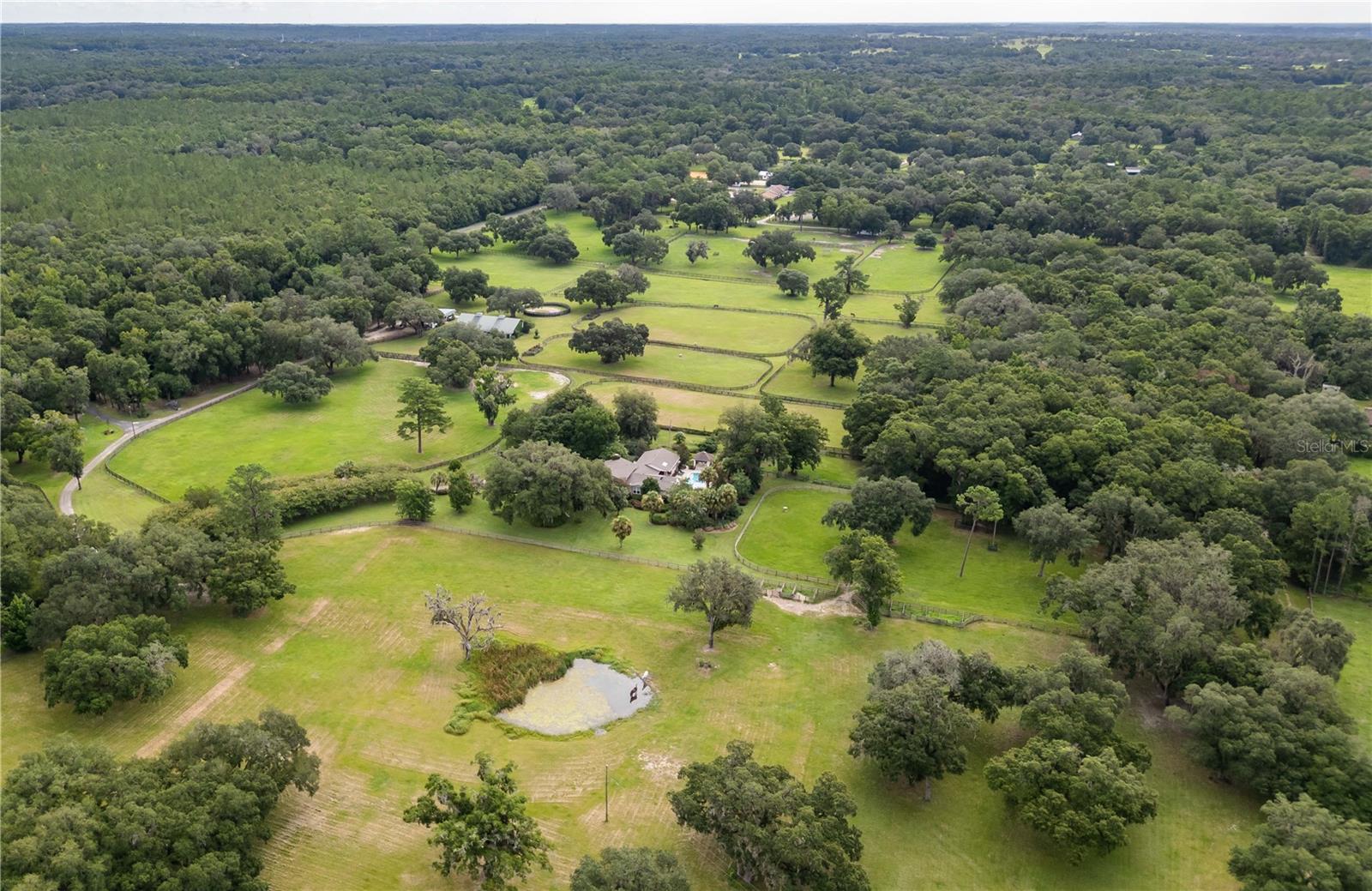 Located on a quiet country road in NW Marion County, River Mist Farm offers 42 stunning acres of lush pastures, majestic live oaks, beautiful gardens, and exceptional privacy. A newly added driveway winds beneath crepe myrtles to the front of the 3-bedroom, 3.5-bath multi-story home, freshly painted inside to create a light and bright atmosphere throughout. With nearly 4000 sq ft the home features bamboo wood flooring, abundant natural light, a spacious chef’s kitchen with Thermador gas range and Sub-Zero refrigerator, expansive living areas, flex spaces, wine cellar/safe room, and a luxurious primary suite with wood-beamed ceilings and private pool access. Designed for both relaxation and entertaining, the outdoor living area includes a sparkling pool, summer kitchen, gazebo, koi pond, bocce court, and beautifully established gardens with a greenhouse/garden shed. Additional highlights include high-impact windows, whole house generator, tornado closet, and a 2024 roof. Equestrians will appreciate the impressive 8-stall block barn with office, bathroom, and loft, plus a secondary 4-stall barn, 12 paddocks, feeder pens, and round pen. Ideally located less than 10 minutes from HITS and 15 minutes from WEC and OBS, this exceptional farm offers the perfect opportunity to live the Ocala equestrian lifestyle.