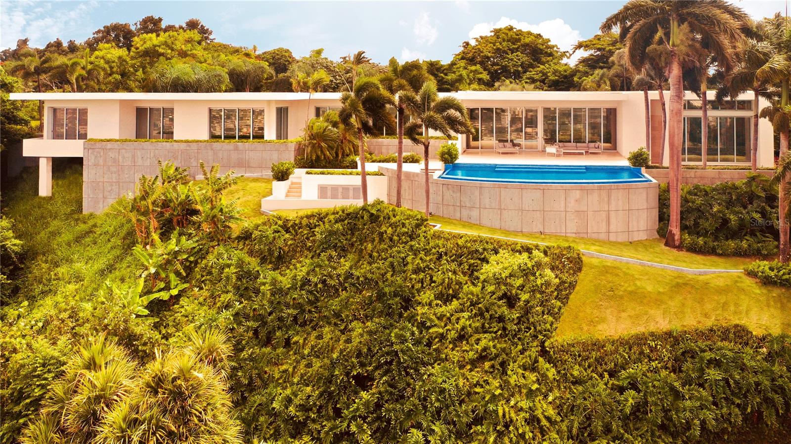 Perched on the rolling hillsides of Guaynabo, Puerto Rico, The Hilltop Residence offers a unique and unparalleled living experience where luxury meets breathtaking natural beauty. Seamlessly integrated with its surroundings, this extraordinary property captivates you from the moment you arrive.

Crafted to fit the landscape, The Hilltop Residence showcases bespoke craftsmanship and elegant design. This predominantly single-story home stretches along a narrow spine, ensuring every room captures natural light and city views. High ceilings and floor-to-ceiling sliding doors pocket into the walls, blurring the lines between indoor and outdoor spaces and creating a harmonious flow throughout the home.

With 7,306 sq. ft. of indoor living space and 4,296 sq. ft. of outdoor areas, the property boasts a total livable space of 11,602 sq. ft. Expansive, open-concept living areas extend effortlessly onto vast terraces, perfect for entertaining guests while enjoying breathtaking panoramic vistas. The infinity pool serves as the centerpiece of outdoor gatherings, offering a serene spot to lounge and soak in the stunning scenery. Spanning 1.22 acres of land, The Hilltop Residence embodies elegance and features essential modern resilience. It is equipped with a robust underground cistern and full-power generator, each with dedicated rooms, ensuring uninterrupted comfort and security.

Embracing tropical modernism, this custom home epitomizes elegance, sophistication, and a living experience unlike any other. Schedule a private showing today to witness firsthand the seamless blend of luxury and natural beauty that defines The Hilltop Residence.