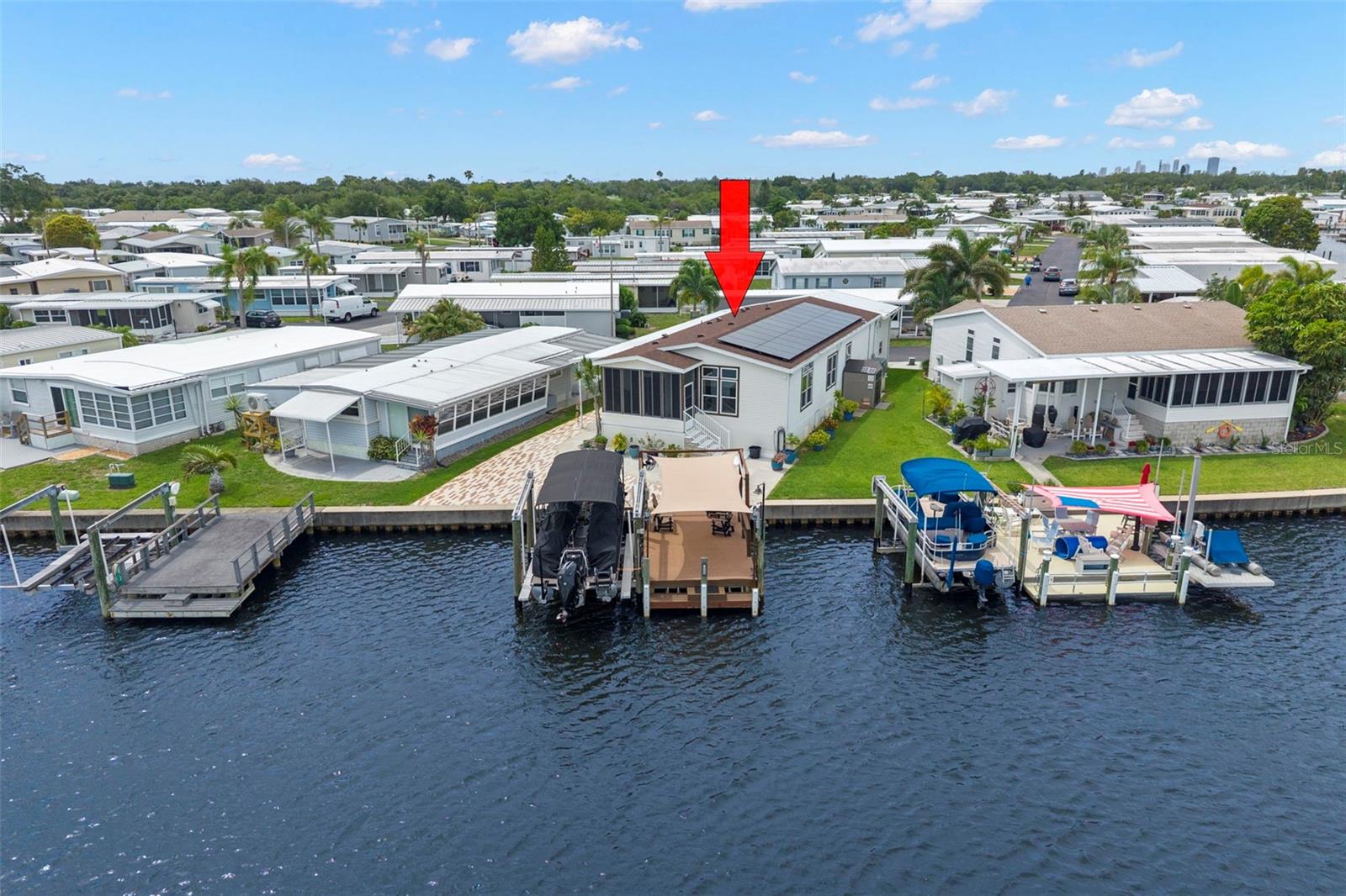 You will be impressed! For the discerning buyer who appreciates a well-maintained waterfront property that is filled with little extras that will make your retirement living carefree. This 1,500 sq. ft 2 bed/2 bath/den home custom-built in 2010 to Winds Zone III standards does not disappoint. The upgrades and features are exceptional: 1). 2025 composition shingle roof with solar panels and transferrable warranty--electric bills average $40 monthly! 2). Central air/heat new in 2024. 3). Upgraded 30 gal water heater. 4). 2022 composite dock with sunshield and 2025 boat lift--take a cruise to Tampa Bay with no bridges. Concrete seawall is maintained by the Co-op, a great value for owner! 5). 2-story golf cart garage with hand painted tropical mural and two-car carport. 6). Extra storage shed on west side of home. 7). Chef's kitchen with high-end stainless appliances, large island and views of the water! Kitchen opens to living room and porch with vinyl windows to enjoy even on windy days. 8). Primary bedroom with ensuite bath is an owner's retreat complete with walk-in closet and additional large closet in bathroom. 9). Comfortable guest bedroom and bath offers guests a hotel like stay! 10). Utility room with 2024 washer and dryer, sink and storage. 11). Details like modern ceiling fans with remotes, custom blinds, 5" crown molding and baseboard, custom shelving in closets and artist painted horizon window showcase the luxury feel of the home. 12). Irrigation system, pavers to dock and lush landscaping round out the outdoor setting. Price includes share for the lot and ownership in the Co-op. This quality home is located in one of the most popular factory-built housing communities in the county that is located only 10 mins to downtown St. Petersburg, 20 mins to downtown Tampa and two airports and 25 mins to beautiful beaches. 4th Street shopping, dining, grocery are minutes away.  2 pets (dogs or cats) up to 35 pounds are welcomed. Renting is allowed with 2-month minimum. Low monthly maintenance fee of $410 includes clubhouse, fitness center, heated pool and tiki area, billiards, two private boat ramps, 24 hr manned gate and so much more! If it sounds too good to be true, then come and take a look!