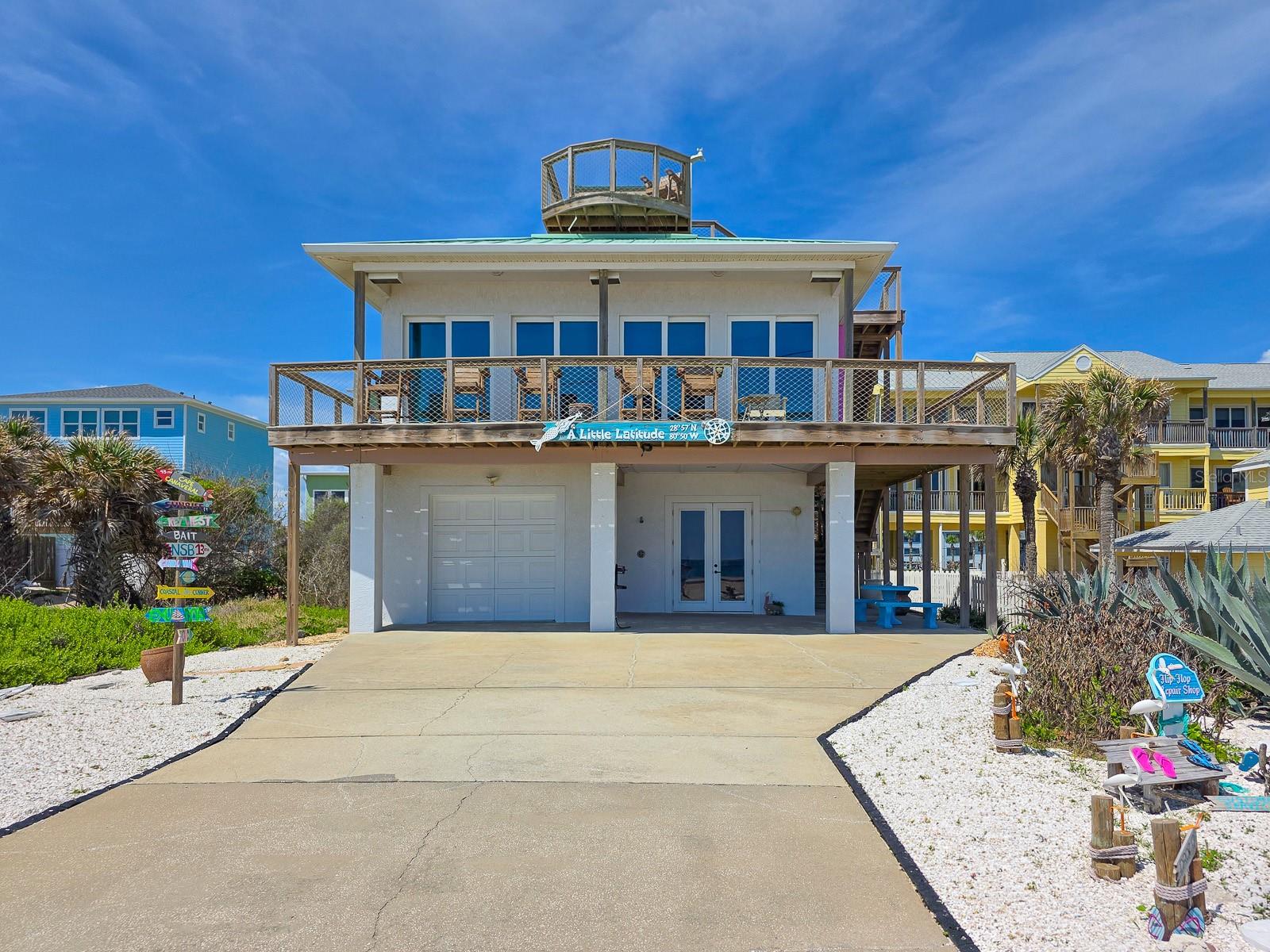 Welcome to “Little Latitude,” a one-of-a-kind oceanfront retreat set along the picturesque Bethune Beach Promenade. This vibrant beach house captures the carefree Margaritaville spirit with a perfect blend of coastal charm and relaxed elegance. Step into a world where every detail invites tranquility — where dual panoramic views of the Atlantic Ocean and Intracoastal Waterway frame your days. This custom home features over 1,100 SF of elevated outdoor living space, including multiple oceanside decks and a sheltered rooftop crow’s nest offering breathtaking views of rocket launches from the Kennedy Space Center. Designed for versatility, this property offers two separate living spaces with private entrances—ideal for multi-generational living, guest privacy, or rental income potential.  The main level offers 2 bedrooms and 2 full baths with an open-concept living area, floor-to-ceiling oceanfront sliders, a spacious kitchen with breakfast bar, and a dining area showcasing panoramic views. The lower level features 2 bedrooms and 1 bath, a cozy living area, and a kitchenette with full-size appliances.  Enjoy seamless indoor-outdoor living with wrap-around decks, tropical landscaping, and beach access just steps away. Whether watching dolphins at sunrise, rockets launching at sunset, or relaxing under the stars, “Little Latitude” is a coastal haven where every day feels like a vacation. Additional features include: laundry rooms on both levels, multiple smart TVs, separate entrances for privacy and flexibility, and completely furnished. The county-maintained concrete seawall and staffed lifeguard station provide peace of mind. Meticulously maintained and updated with new windows, sliders and exterior doors, tile flooring throughout, two HVAC systems, and a new metal roof (2023). The property also offers an outdoor shower, firepit, BBQ area, and enclosed garage.  Manatee Park, located nearby, features a volleyball court, fishing pier, and kayak launch where dolphins and manatees are frequently seen. Within minutes of upscale dining, boutique shopping, private marinas, and the charm of historic Flagler Avenue, this beachfront home offers the perfect balance of exclusivity and accessibility. This is your ultimate entertaining beach home — offered fully furnished, where all you need to bring is your toothbrush --and maybe your flip flops. Come see this unique property for yourself and make it yours today!