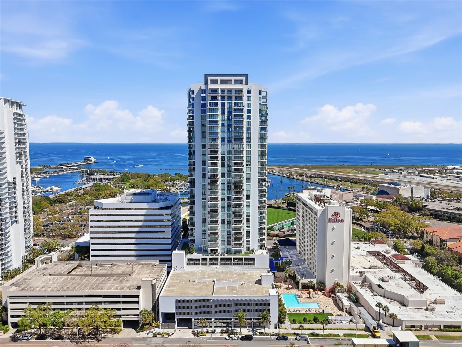 SEASONAL RENTAL at St. Pete’s newest luxury downtown waterfront building, the SALTAIRE. Choose your months between October-June! Nestled in the heart of downtown St Pete, this luxurious fabulously furnished rental offers breathtaking city, water and sunset views. The spacious master features a king bed, spacious ensuite bath with double sinks, huge shower, private toilet area, and an enormous closet. The second bedroom features a queen Murphy bed with a super comfortable mattress, an ensuite bathroom with shower, plus  a sit/stand desk on wheels with a Thunderbolt plug in (just bring your laptop, plug in and you can use the keyboard, mouse and two large monitors. There is also a large DEN with a 75” smart TV, featuring motorized stadium leather couch seating across from a guest half bath.  The huge “smart” family room features a comfortable leather sofa with three motorized loungers, a 120” state-of-the-art projection TV that rises from the floor and a Sonos surround sound system. Electronic motorized blinds have been installed throughout the entire condo which include black out shades and sunscreen shades. The fully-equipped kitchen includes granite countertops and backsplash, gourmet, stainless steel JennAir appliances (a 42” built-in, French door refrigerator, microwave, convection oven, flat cooktop, and stainless-steel exhaust hood), imported Nolte European cabinetry and an island bar with adjustable height bar stools should you need to seat more people at the large stone-top dining table. This unit has literally everything you need to enjoy a winter in St. Pete including a large private balcony where you can unwind while soaking in the panoramic sunset vistas. The building’s enormous 7th floor amenity deck features a huge resort-style pool & Whirlpool spa overlooking Tampa Bay, the GRAND PRIX and the Rowdies stadium, pool cabanas, cozy fire pits with couch seating, gas and electric BBQ’s, lounging areas and a large bar with an oversized flat screen TV. There’s also a state-of-the-art fitness center, large social room for entertaining or just relaxing, a Club area for working, card and board game playing, a catering pantry, and complimentary wireless internet access. In addition to these resort quality amenities, Saltaire residents enjoy 24/7 front desk staff, a concierge, and a social director who organizes lots of social activities from canasta and trivia games to weekly yoga classes. Enjoy the convenience of walking to shops, restaurants, local events and area attractions. If you want to winter in St. Pete, or are thinking of moving to the Tampa Bay area, this is your chance to experience luxury downtown living at its finest.