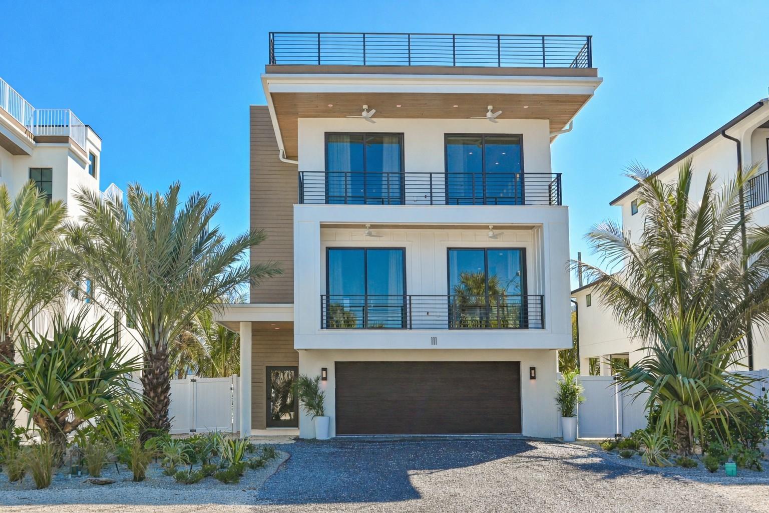 Experience elevated island living in this exceptional brand-new custom four bedroom four and a half bath coastal retreat by Eason Builders Group Construction, ideally positioned west of Gulf Drive on Anna Maria Island just moments from the sugar-white sands and turquoise waters of the Gulf. Thoughtfully designed to capture both refined personal enjoyment and outstanding vacation rental performance, this architecturally striking residence blends sophisticated design, superior craftsmanship, and effortless indoor-outdoor living in one of the island’s most coveted locations. From the moment you enter, soaring ceilings with rich wood detail and expansive walls of impact-rated glass create a dramatic yet relaxed coastal ambiance filled with natural light. The open-concept floor plan is ideal for entertaining, seamlessly connecting the main living areas while maintaining an intimate, luxurious feel. The chef’s kitchen serves as the heart of the home, featuring an oversized quartz island with ample seating, custom cabinetry, premium appliances, designer lighting, and abundant storage. The kitchen flows effortlessly into the spacious great room, highlighted by a sleek modern fireplace and dramatic sliding glass doors that open to covered terraces, creating the ultimate setting for indoor-outdoor gatherings. The private elevator offers convenience & accessibility. Step outside to your private resort-style backyard oasis where a stunning heated pool with elevated spa takes center stage. Generous covered lounge areas, outdoor dining space, and lush tropical landscaping provide both privacy and year-round enjoyment, offering owners & guests a true boutique resort experience. Whether hosting sunset cocktails or enjoying a quiet afternoon poolside, this outdoor environment is designed for relaxation and entertainment. Each beautifully appointed bedroom offers a tranquil retreat, while spa-inspired bathrooms elevate daily living with freestanding soaking tubs, glass-enclosed showers, dual vanities, & upscale designer finishes. A thoughtfully designed custom bunk room enhances flexibility & maximizes short-term rental occupancy, making the home especially appealing for larger groups & multi-generational stays. Crowning the residence is an expansive rooftop deck delivering sweeping Gulf views. This spectacular vantage point creates an unforgettable setting for sunset gatherings, morning coffee, or evening stargazing—one of the most desirable features for both homeowners & vacation guests alike.
Beyond the property itself, embrace the quintessential island lifestyle. Leave the car behind & explore by golf cart or bicycle, cruising to the charming boutiques, art galleries, & acclaimed restaurants along Pine Avenue. Enjoy morning beach walks, afternoons on the water, and evenings filled with breathtaking Gulf sunsets just steps from your door. Built with impact windows and doors, high-end designer finishes, and meticulous attention to detail throughout, this residence offers both peace of mind and enduring quality. With projected annual rental revenue of approximately $400,000, the home presents a compelling investment opportunity while delivering an unparalleled luxury lifestyle. Combining prime west-of-Gulf Drive positioning, exceptional craftsmanship, resort-style amenities, and strong income potential, this remarkable property represents the very best of Anna Maria Island living.