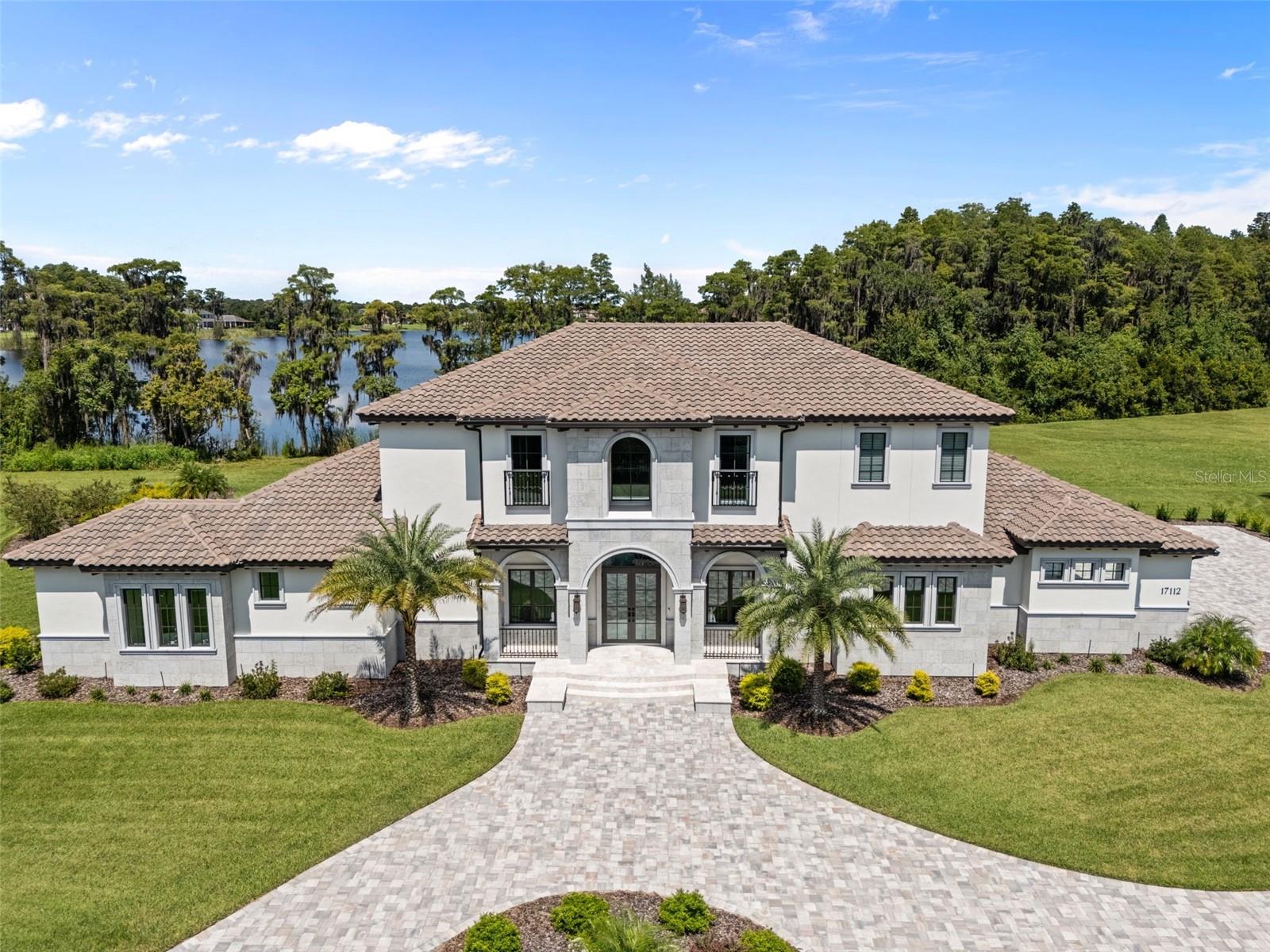 Experience luxury lakefront living in this elegant 2-story Italian-inspired Mediterranean home located on 12 acres (approx. 6 acres upland and 6 lowland) in an exclusive gated enclave of the equestrian friendly community of Steeplechase. Custom-built by Charter Bay Home Builders in 2023, this home boasts 5,563 sq ft of living space and overlooks the picturesque 26-acre Velburton Lake, a private, nonmotorized lake. This home offers the ultimate in peace, quiet, and privacy. The oversized lot is ideal for horse enthusiasts, as it allows (w/ HOA approval) for the construction of a barn and up to 2 horses—an option available to only a handful of Steeplechase properties. This expansive home features five spacious bedrooms, five bathrooms, a den/office, a bonus/media room, and a 3-car garage. Designed for entertaining, the open floor plan boasts 12’ ceilings, a gorgeous gourmet kitchen equipped with a 48” gas range, 30”column refrigerator and 30” column freezer, and an impressive kitchen island that comfortably seats five. The spacious walk-in pantry provides ample storage space with built-in cabinets. The Great Room features a wall of glass doors which flood the space with natural light and offers exceptional views and access to the pool and lake. The fenced pool and spa overlook the lake alongside a large screened outdoor living area which includes a built-in BBQ, wet bar and fridge, as well as access to the pool bath. The primary bedroom is located on the first floor with french doors offering sunset views of the lake and access to an outdoor sitting area, the pool and spa. The luxurious primary bath includes separate vanities, a soaking tub, and an expansive walk-in shower. A large office/den is located on the 1st floor off the Great Room which could also be used as a nursery, exercise room, or 6th bedroom. Four additional bedrooms are located upstairs, offering privacy and comfort. One of the bedrooms, along with the bonus/media room, lead to a screened balcony, perfect for enjoying sunsets over the lake. For added convenience, the home includes two well-appointed laundry rooms, one on each floor. Just 20 minutes from Tampa International Airport, this home combines luxury, tranquility and convenience.