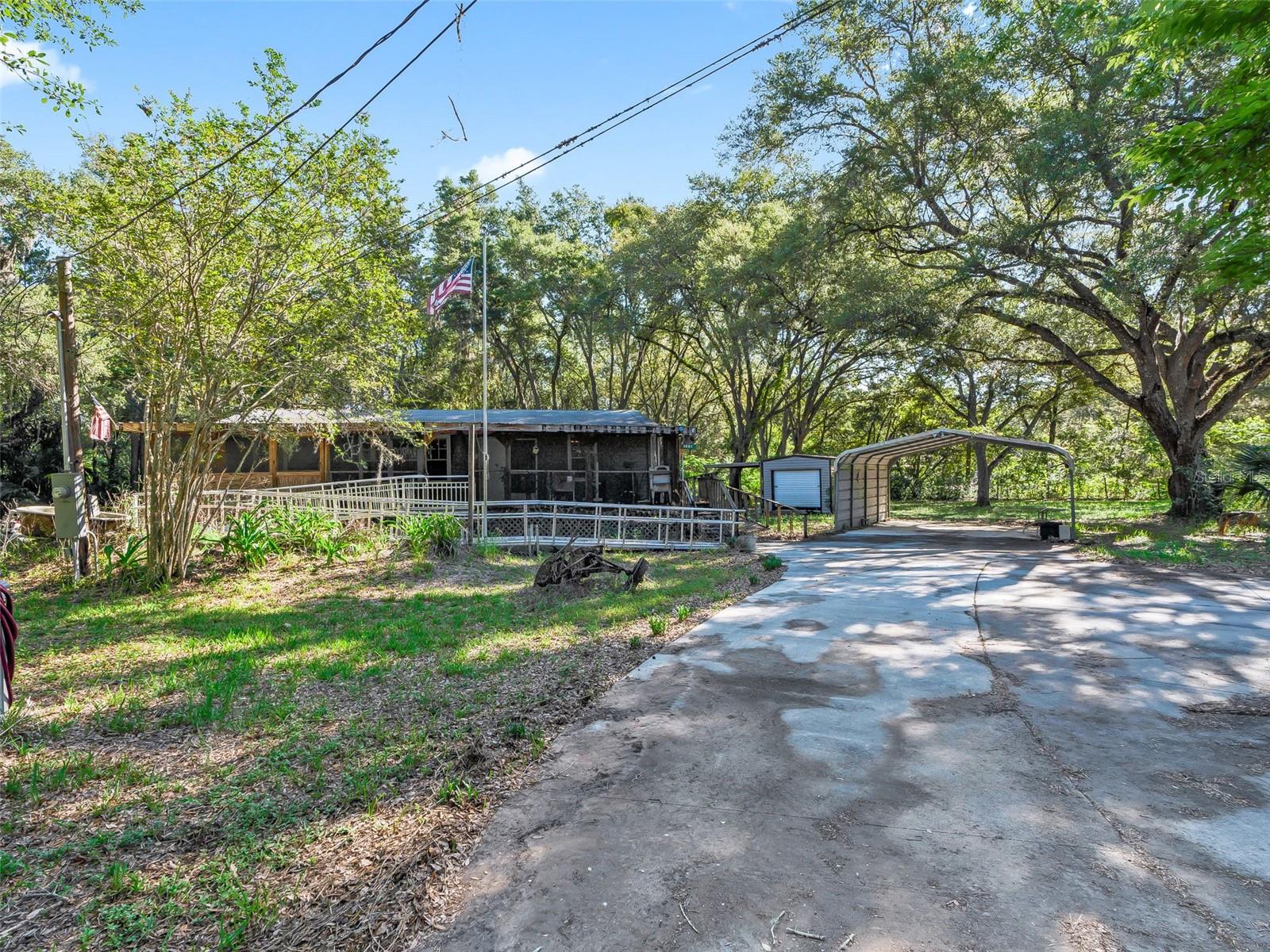 NO HOA!! Affordable country charm with privacy, space, and potential. Bring your vision and make this peaceful retreat your own. This 2015 3-bedroom, 2-bath home is a wonderful opportunity for first-time homebuyers, downsizers, or anyone seeking peaceful country living with convenience. Situated on just under an acre at the end of a quiet road, this private setting is surrounded by beautiful oak trees and backs up to 800 acres, offering a serene backdrop and added privacy.Enjoy relaxing mornings on the screened porch or entertain outdoors with the cozy outdoor kitchen area. Inside, the cute country-style kitchen features an island and opens to comfortable living spaces ready for your personal touch. The home offers a handicap-accessible ramp to the front entrance, a covered carport, a storage shed with electric, and an additional lean-to for extra storage.Centrally located with convenient access to the Turnpike and within reach of Ocala, Tampa, and Orlando, this property offers peaceful living without sacrificing accessibility. With a little love, this could be the perfect place to call home. Schedule your private showing today!