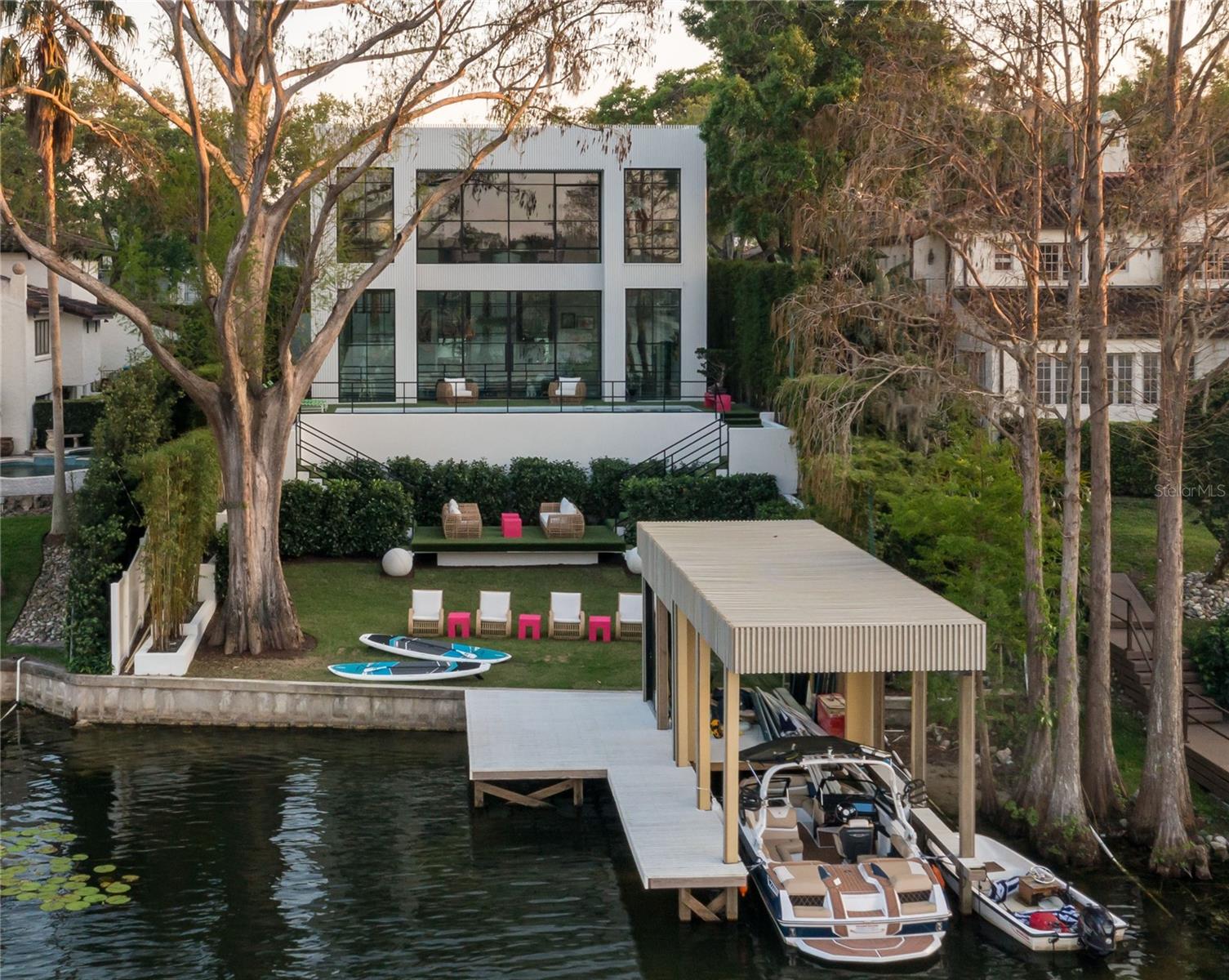 An architectural triumph, this one-of-a-kind modern masterpiece was custom designed and built in 2023 by the award-winning Z Properties and is ideally sited on the shores of Lake Osceola, part of the Winter Park Chain of Lakes. Radiating bold sophistication and contemporary elegance, the residence is a curated work of art, where floor-to-ceiling glass walls and striking steel windows and doors flood the interiors with natural light and deliver unobstructed panoramic lake views from nearly every room. Enter through a dramatic 12-foot glass pivot door into a 21-foot-long art gallery foyer adorned with a sculptural linear chandelier and Venetian plaster walls and ceilings that lend a soft, refined texture. The open-concept living spaces are accentuated by terrazzo floors, 12-foot ceilings, and thoughtful spatial design—including a great room with a sitting area and dining space, a separate media room concealed behind custom 12-foot decorative doors, and a sleek galley-style kitchen outfitted with fully integrated Miele appliances and a secondary glass pivot door for seamless indoor-outdoor flow. Ascending one of two custom staircases, the second floor features warm hardwood floors and a showstopping primary suite that feels suspended above the lake, backyard and pool. This serene retreat offers an all-glass shower, spa-inspired soaking tub, beautifully finished bath cabinetry, and an upholstered wall that subtly conceals a walk-in closet and built-in storage. A second bedroom suite offers an inspired use of space with clever screen walls for privacy and flexibility. Detached from the main home, a third bedroom suite doubles as a guest house, home office, or gym, complete with an en-suite bath, custom built-ins and a wet bar. Outside, the terraced backyard is a tranquil oasis with a saltwater pool and spa, turf lawn for year-round perfection, dual staircases leading to a sundeck and a private, covered boat dock crowned by a glass-enclosed studio mirroring the home’s signature design. Bamboo privacy walls, soaring palms, and a Banyan tree imported from South Florida create a lush and artful landscape. The two-car garage includes epoxy flooring and dual EV charging stations. A singular residence in every sense, this home blends innovative architecture, luxurious finishes and thoughtful design into a rare offering unlike anything else in Winter Park. Built by Z Properties, celebrated in Florida Design and numerous design publications, this is a home for those who appreciate beauty, intention and the art of living well.