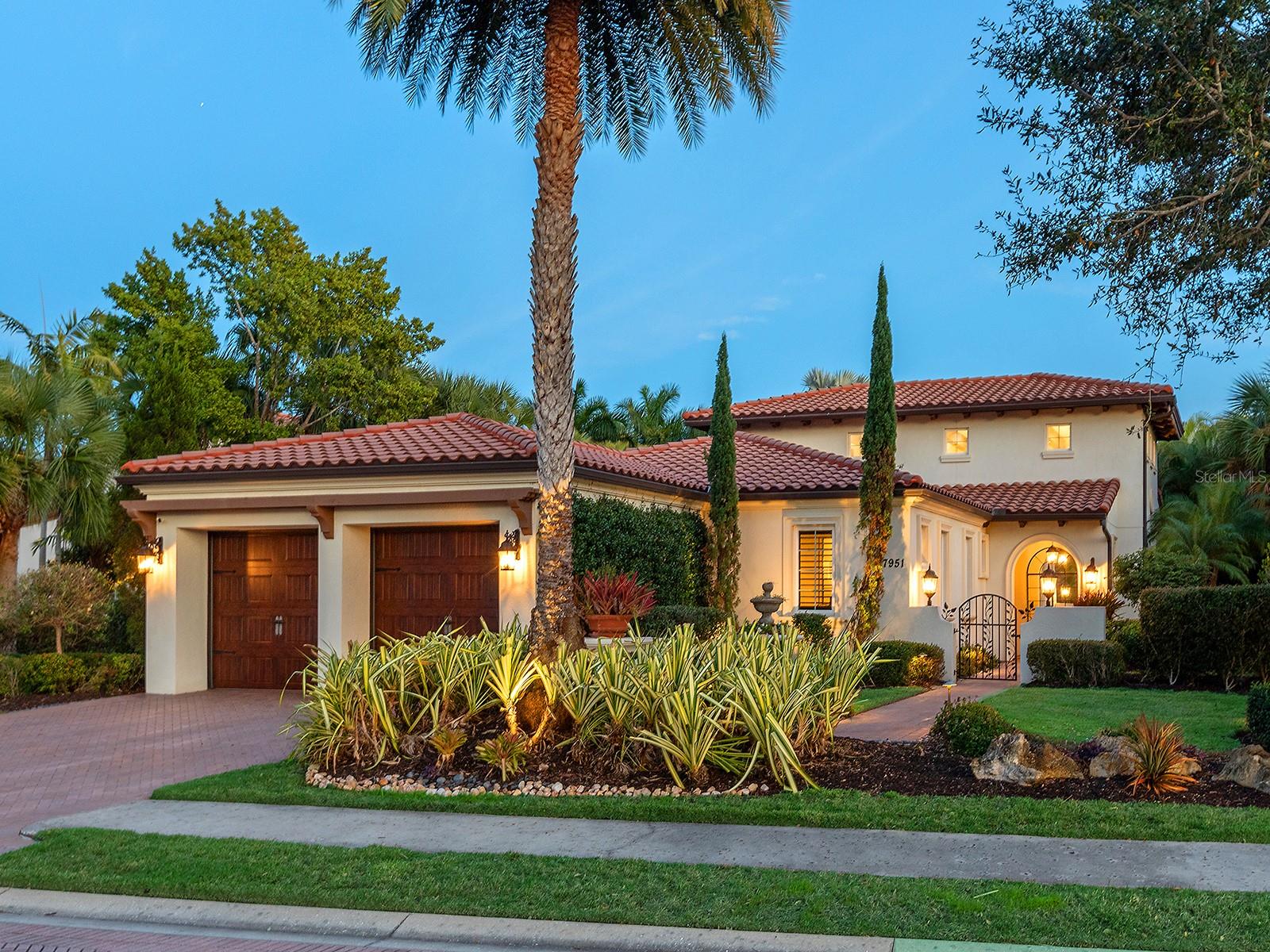 Set within The Lake Club at Lakewood Ranch, this home offers thoughtfully designed indoor–outdoor living, introduced by a gated courtyard entry, paver drive, paver walkways, landscaped grounds, exterior lanterns, and a landscaped front island. Travertine flooring spans the main living areas, with engineered wood floors throughout all bedrooms. A glass front door opens to a foyer with grasscloth wallcovering, while center-pocketing impact-rated sliders connect the great room directly to the lanai. The great room features plaster-textured walls, crown molding, brick archways, soaring 18-foot ceilings with exposed beams, abundant natural light, and motorized shades. The kitchen centers around an oversized island with extended breakfast bar seating and includes a Thermador appliance suite with a paneled refrigerator and freezer, a gas cooktop with griddle, double ovens, a warming drawer, a microwave, a paneled Bosch dishwasher, and a U-Line wine cooler. Additional features include granite countertops, a coffee bar, pot filler, decorative backsplash framed by wood and brick, custom pantries, and upgraded lighting, with the dining area positioned nicely between the kitchen and family room, making it ideal for entertaining. The primary wing features French doors to the lanai and is adorned with walls of windows overlooking the pool, fire pit, and lake. Additionally, this primary suite is appointed with crown molding, designer draperies, and motorized blinds. The luxurious bath offers separate granite vanities, a floor-to-ceiling tiled walk-in shower, a sunken soaking tub framed by windows, and a private water closet. The expansive custom closet includes built-ins, a center island with locking drawers, an integrated hamper, and a chandelier. Both guest bedrooms are en-suite. One guest bedroom is equipped with a double-door entry and a custom Murphy bed, and the other offers a built-in closet, granite vanity, and a walk-in shower with ceiling-height tile and a window. Interior features also include a half bath with a brick archway and linen storage, hallway storage, and a laundry room that includes granite counters, ample cabinetry, a sink, a window, and trim detailing. The lanai features a heated saltwater pool and spa with a Pentair heater, paver decking, exposed ceiling beams, dual ceiling fans with lighting, motorized shades, remote-controlled awnings, and brick archways. A linear electric fireplace finished in Crema Marfil marble with built-in bench seating and a gas fire pit overlooking the lake. The outdoor kitchen includes granite countertops, a sink, hood, new beverage refigerato and complementary brick and Crema Marfil finishes. FGBC-certified for energy efficiency and comfort, this smart home features Icynene spray-foam insulation, LED lighting, tankless gas water heater, whole-house generator, EV charger, whole-house water filtration with reverse osmosis, and Control4 and Sonos whole-home audio. Smart controls manage security, cameras, thermostat, garage doors, motorized blinds, and water heater, while the epoxy-finished garage includes EV and generator hookups. Located in The Lake Club’s maintenance-free section with pool care and landscaping included, residents also enjoy resort-style amenities such as a clubhouse, pool, fitness center, tennis and pickleball courts, dining, social events, and scenic lakes for kayaking and fishing, just minutes from top-rated schools, shopping, dining, and Sarasota’s beaches.