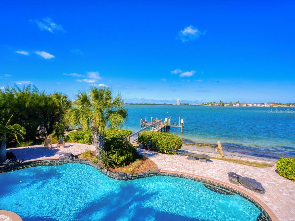 Take advantage of this rare opportunity to own your very own slice of paradise along the crystal blue waters of world-famous Siesta Key. Located in an ideal location on the preferred north end of the island, and boasting stunning panoramic views of Downtown Sarasota, Bird Key, Lido Key, the John Ringling Causeway, and Big Pass, this property encompasses over 161’ waterfront feet on 2 sides (98’+ on the bay and 63’+ on the protected water of Bayou Louise) and offers one of the area’s most coveted lifestyles. For the avid boater, there is a brand new fully equipped dock with 16,000lb lift and seating to take in the amazing views and daily sunsets. In addition, there is a boathouse with a dock on Bayou Louise. Relax after a day on the water in the resort-style backyard featuring a private beach, a pool with a rock waterfall, covered and uncovered seating areas, and a putting green. Complementing the exterior, the interior exudes a laid-back island vibe and boasts a large living and dining room featuring original Terrazzo floors, a wood-burning fireplace, a built-in bar, and a wall of windows on either side of the home that let the natural light shine through providing incredible water views. The kitchen remains true to the style of the home yet updated for today’s needs and features abundant natural light, functional cabinet space, stainless steel appliances, a large butler’s pantry, and a corner banquette. The master suite is located on the second floor with a private terrace overlooking the water while the three ensuite bedrooms on the main living level offer plenty of privacy for family and guests. Enjoy it just the way it is right now while you design your new dream waterfront home. The current owners have had a plan created by award-winning architect Mark Sultana of DSDG Architects.
