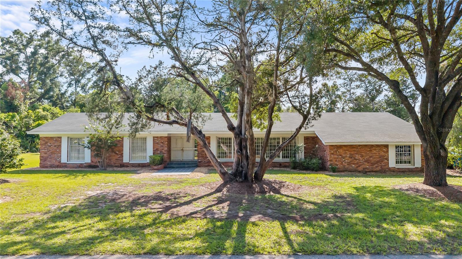 Virtually Staged. A Timeless Southern Classic in the Heart of Chiefland!

Welcome to 214 SE 2nd Street, a truly one-of-a-kind residence where timeless elegance, exceptional craftsmanship, and enduring quality come together on 1.55 beautifully landscaped acres in the heart of Chiefland. Built in 1963, this remarkable home offers 2,622 heated and cooled square feet, 4 bedrooms, 3 full bathrooms, and architectural details that are nearly impossible to find in today's homes.

Constructed of concrete block with hand-selected brick, this home was built to stand the test of time and showcases a level of craftsmanship rarely seen today. From the moment you step through the slate tile entry into the stunning marble-floored foyer, you'll immediately appreciate the quality, attention to detail, and timeless character found throughout. Floor-to-ceiling windows bathe the home in natural light, highlighting the rich hardwood floors, elegant marble accents, and unique antique architectural features that make this home truly unforgettable.

Designed for both gracious entertaining and comfortable everyday living, the spacious floor plan features formal living and dining rooms separated by a striking decorative marble and slate divider wall, creating an elegant centerpiece unlike anything found in modern construction. The inviting family room and adjoining dining nook offer custom built-in bookshelves and a charming corner brick fireplace, providing the perfect gathering place for family and friends.

The kitchen is rich with vintage charm and craftsmanship, featuring a brick breakfast bar, solid wood cabinetry, pantry, and original vintage appliances that beautifully complement the home's classic design and enduring appeal.

The spacious primary suite and three additional bedrooms all feature beautiful hardwood flooring, while the three tiled bathrooms continue the home's timeless style and quality finishes.

Practicality meets beauty with an oversized attached two-car garage offering generous storage and workspace, along with a large detached storage building/workshop that's ideal for hobbies, woodworking, gardening, equipment storage, or creating your dream studio.

Step outside to experience your own private park. Majestic granddaddy oak trees, towering magnolias, mature camellias, and lush landscaping surround the property, creating a peaceful, picturesque setting that feels worlds away while remaining conveniently located in the heart of Chiefland. This rare in-town acreage offers the perfect balance of privacy, beauty, and convenience, just minutes from schools, shopping, restaurants, parks, and medical facilities.

Homes of this caliber are rarely offered. More than just a house, this home is a piece of Chiefland's history—a home built with pride, designed to last for generations, and filled with character that simply cannot be recreated. If you've been searching for timeless Southern charm, exceptional craftsmanship, and a truly distinctive property, this is your opportunity.

Don't miss your chance to own one of Chiefland's iconic homes. Schedule your private showing today and experience the elegance, history, and craftsmanship this remarkable property has to offer.