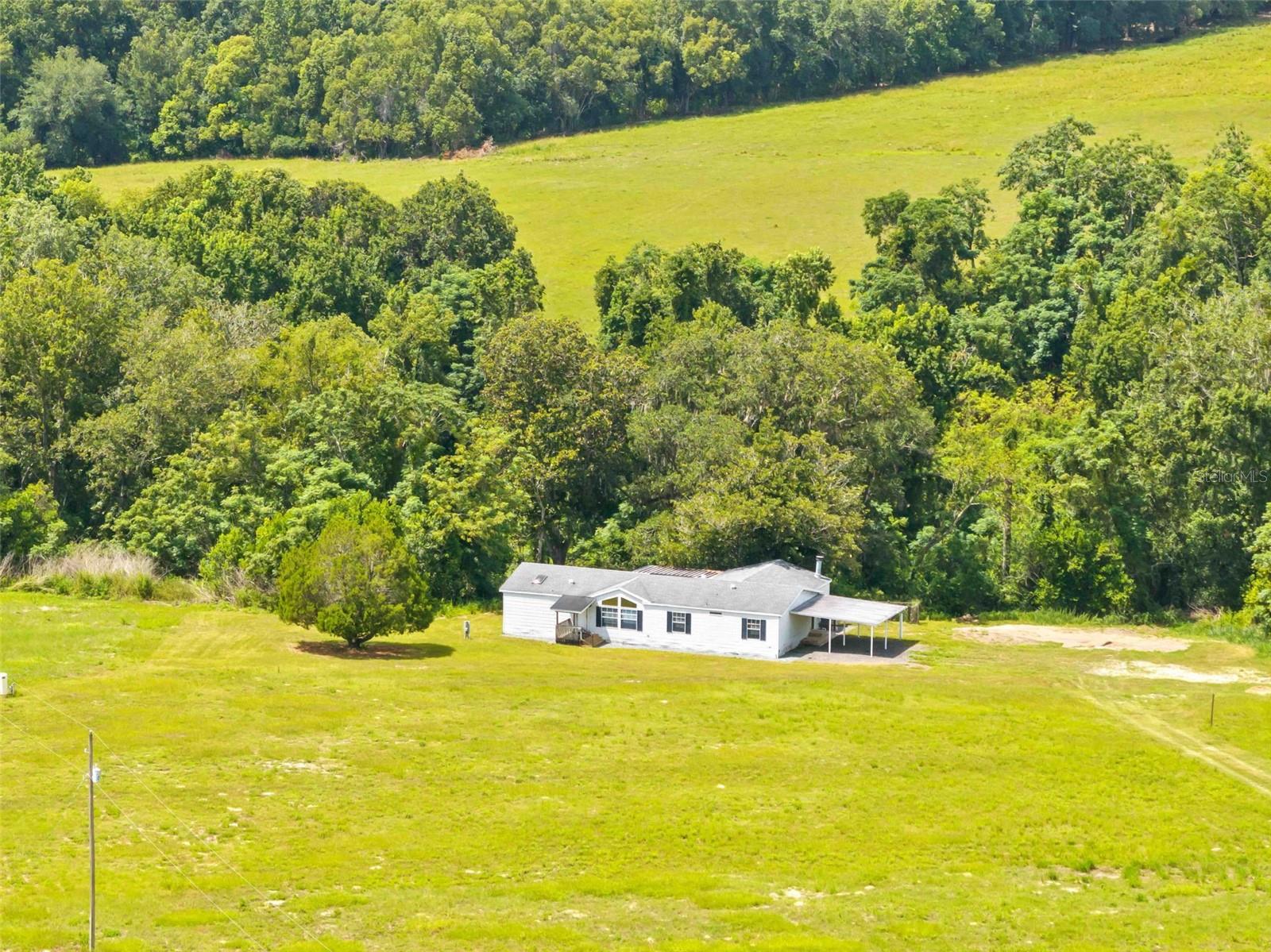 NEED ROOM TO ROAM, START A HOBBY FARM, OR SIMPLY ENJOY PEACE & PRIVACY? This is the opportunity you've been waiting for! Nestled on 10 BEAUTIFUL ACRES in the HIGHLY DESIRABLE DADE CITY AREA, this spacious 2,040-square-foot triple-wide home offers the perfect blend of country living and modern comfort, with 2,801 square feet under roof. Thoughtfully maintained, the home features 3 BEDROOMS and 2 BATHS, including an OVERSIZED PRIMARY SUITE complete with a PRIVATE EN SUITE BATH featuring a relaxing GARDEN TUB, separate WALK-IN SHOWER, WALK-IN CLOSET, and DIRECT ACCESS to a LARGE REAR DECK overlooking the backyard. Bedrooms two and three are generously sized and share a well-appointed guest bath. The OPEN-CONCEPT living and dining areas are ideal for entertaining, featuring a breakfast bar overlooking the kitchen, a cozy WOOD BURNING FIREPLACE, and French doors leading to a LARGE SCREENED PORCH where you can relax and enjoy the peaceful surroundings. MAJOR UPDATES provide peace of mind, including a 2020 ROOF, HVAC and WATER HEATER approximately 3 YEARS OLD, and a NEW WELL installed in 2025. The home is constructed with DRYWALL THROUGHOUT, offering the look and feel of a site-built residence. Outside, a 2 CAR CARPORT provides covered parking, while the home is POSITIONED WELL OFF THE ROAD to maximize privacy. A SEASONAL CREEK winds through the rear of the property, attracting abundant wildlife including deer, turkey, and other native species, creating a true nature lover's paradise. Conveniently located JUST 3 MILES FROM I-75, this property offers an easy commute to Tampa, Orlando, and surrounding communities, while still providing the tranquility of country living. You're also approximately 30 miles from the Gulf of America, where boating, fishing, scalloping, swimming, and Florida's beautiful Nature Coast await. Just minutes away, HISTORIC DOWNTOWN DADE CITY offers charming local shops, restaurants, and year-round community events, including the nationally recognized Kumquat Festival, festive Christmas parades, farmers markets, and numerous seasonal celebrations that make this community such a special place to call home. Whether you're looking to establish a hobby farm, bring your horses and livestock, or simply enjoy wide-open spaces and country living, THIS EXCEPTIONAL 10 ACRE PROPERTY OFFERS ENDLESS POSSIBILITIES IN ONE OF DADE CITY'S MOST SOUGHT-AFTER RURAL SETTINGS!!