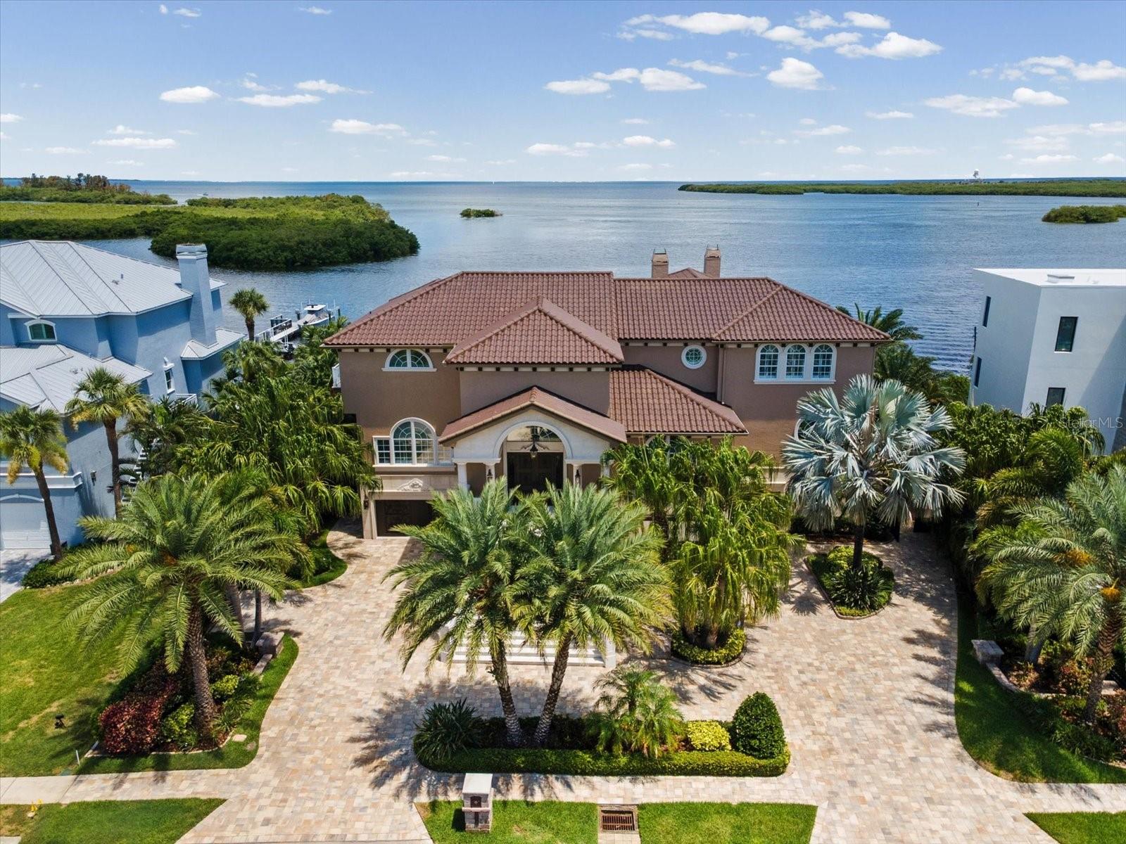 Welcome to an extraordinary waterfront estate in the prestigious gated community of Harbour Watch in Tarpon Springs. Situated on nearly half an acre with 128 feet of protected open-water frontage, this magnificent residence offers breathtaking sunrise and sunset views, abundant wildlife, and direct access to the Intracoastal Waterway, Gulf of America, Anclote River, and the world-famous Tarpon Springs Sponge Docks. Designed for the boating enthusiast, the recently completed custom Ipe wood dock features two 10,000-lb boat lifts and provides the perfect setting for fishing, entertaining, or simply enjoying crystal-clear waters frequented by dolphins and manatees. The seawall and rip-rap shoreline provide added protection and peace of mind. Harbour Watch offers 24-hour gated security and resort-style amenities including a community pool, spa, tennis courts, private dock, and more. The home itself showcases exceptional craftsmanship with soaring coffered ceilings, extensive custom millwork, a dramatic grand staircase, elegant chandelier, and a private elevator servicing all three levels. The main living level is designed for both everyday comfort and grand-scale entertaining. Enjoy a spacious waterfront living room, formal dining room, expansive chef’s kitchen featuring dual Sub-Zero refrigerator/freezers, a gas Wolf range with pot filler, walk-in pantry, wine cellar, and a family room with a gas fireplace. A large climate-controlled enclosed patio extends the living space while capturing stunning water views. This level also includes a full laundry room and three generously sized guest bedrooms with large closets and convenient bath access. Upstairs, a versatile loft entertainment area offers a full bath, wet bar, cooktop, and dual balconies—ideal for hosting gatherings, watching the big game, or enjoying movie nights. Across the catwalk, the luxurious primary retreat spans over 1,400 square feet and features separate his-and-hers walk-in closets, a private waterfront balcony, and a spa-inspired ensuite with a pass-through gas fireplace, copper clawfoot soaking tub, and steam room. Additional highlights include a heated pool and spa, oversized garage with space for up to eight vehicles, bonus room ideal for a golf simulator, theater, fitness studio, or game room, and extra-wide side yards that provide exceptional flexibility for storage, entertaining, or catering access to the backyard. A charming cabana with a large fireplace enhances the resort-style outdoor living experience. At night, the estate transforms into a private waterfront resort, illuminated by authentic Bevolo gas lanterns and extensive custom landscape lighting. Built with quality construction and located within a highly sought-after A-rated school district, this one-of-a-kind residence offers luxury, privacy, and an unparalleled Florida waterfront lifestyle.