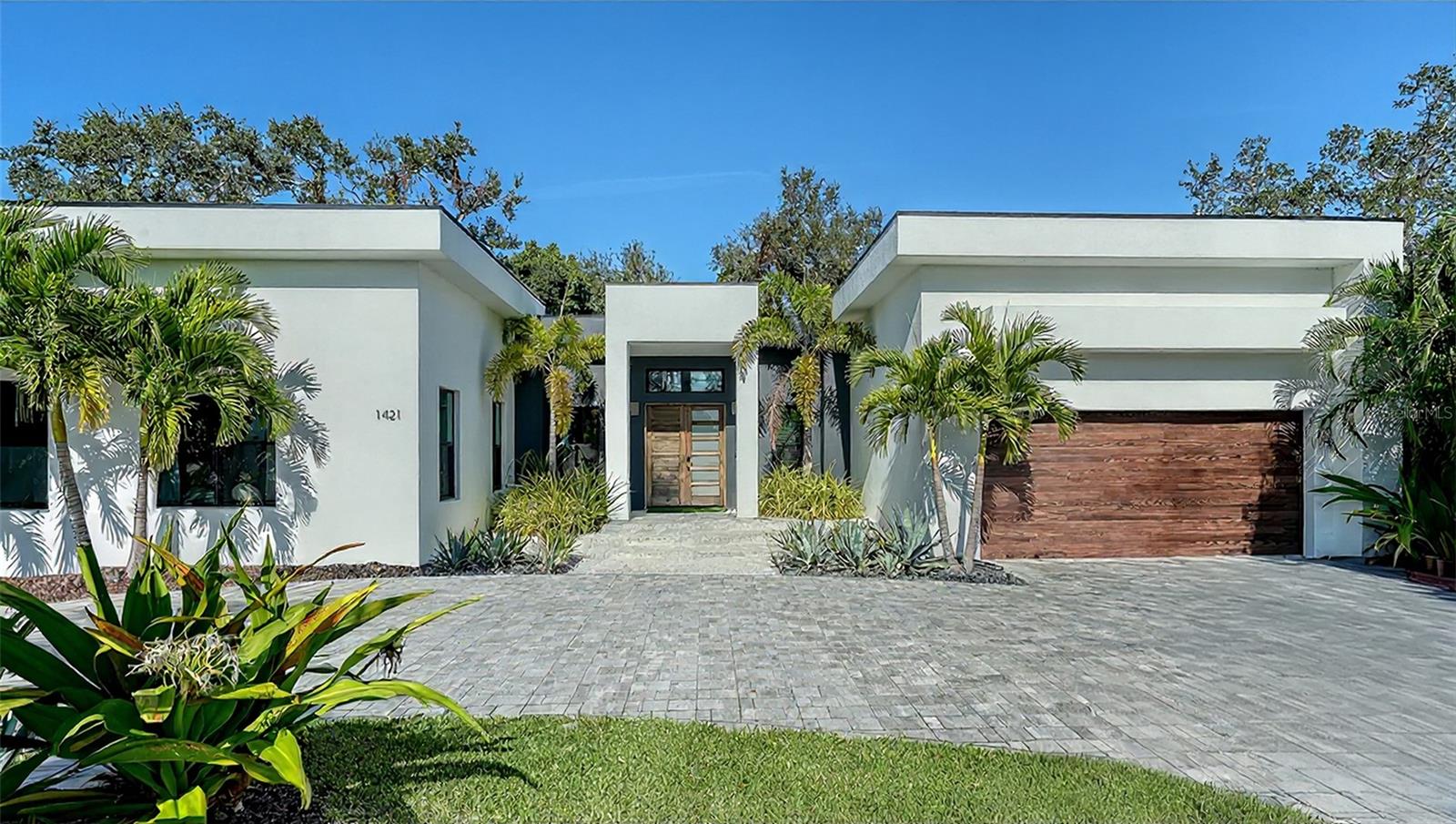 Perfectly positioned on a spacious, private lot in the prestigious and highly sought-after Oyster Bay Estates community, the residence embodies exceptional design, architectural intention, and refined livability. Custom designed and built by distinguished, award-winning Platinum Coast Construction and completed in 2021, this 4-bedroom / 4 full & 2 half bath modern masterpiece was crafted with uncompromising detail and a focus on seamless indoor–outdoor living.  Inside, a host of elevated finishes creates a sophisticated yet welcoming atmosphere. Level 5 flat-smooth walls, engineered oak hardwood flooring, 8' solid-core and obscure glass interior doors, 10" baseboards, floating vanities in all baths, and Quartz surfaces throughout promote a clean, modern aesthetic. A dramatic 72" glass fireplace anchors the living area, while the gourmet kitchen boasts high-performance appliances including a Thermador push-to-open column refrigerator, column freezer, 24" wine preserver, Bosch dishwasher, Bosch combo oven/microwave, and 36” induction cooktop. The striking 175-bottle wine room with stone wall adds a stunning design focal point for entertainers and collectors alike. The primary suite offers a spa-like retreat with marble finishes, a Wetstyle soaking tub, and an enclosed outdoor garden area with tropical landscaping, wood decking, and a private outdoor shower. Guest suites each feature en-suite baths and access to a serene outdoor spa-like space with lush plantings, decking, and an outdoor tub and shower—creating peaceful, private escapes separate from the main living areas. Designed for true resort-style living, the exterior features a spectacular 18' x 30' pool and spa with a custom waterfall wall, surrounded by tropical landscaping. The fully equipped outdoor kitchen includes a 42” Blaze gas grill, under-counter refrigerator, outdoor sink, and storage drawers. Additional features include hurricane-impact windows, an advanced security system, irrigation system, and a distinctive 2-car garage with wood-look paneling and a stunning mahogany double-door entry with obscure glass. Situated just moments from Siesta Key, downtown Sarasota, and within walking distance of the prestigious Field Club, Oyster Bay Estates is celebrated for its beautiful streetscapes, active social atmosphere, and proximity to the water and premier amenities. This exceptional residence offers luxurious contemporary living in one of Sarasota’s most desirable neighborhoods.
