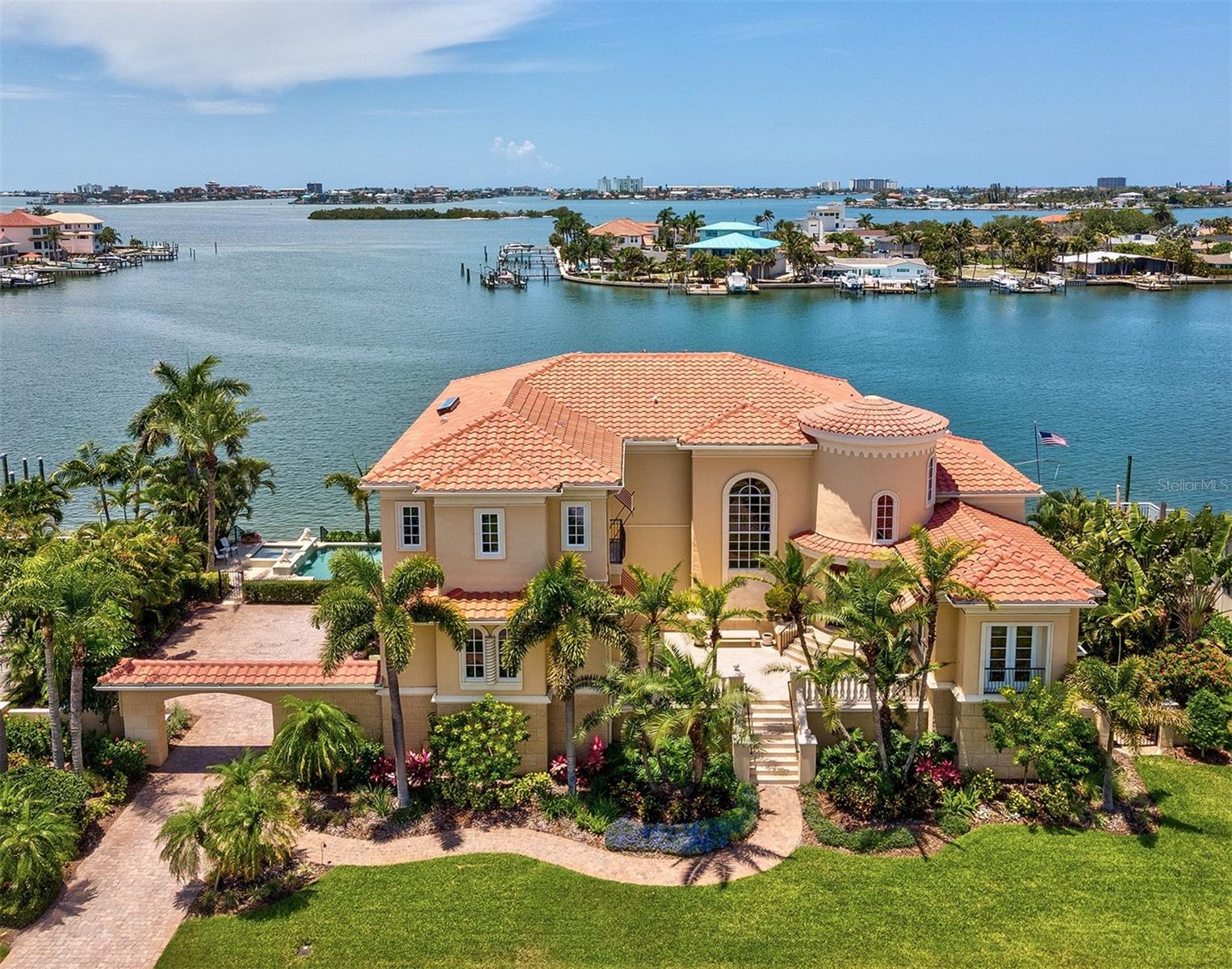 A MAGNIFICENT LUXURY WATERFRONT ESTATE SUPPORTED BY AN IMPRESSIVE DEEP-WATER DOCK WITH MOORINGS FOR A 100FT YACHT! Located in renowned Pasadena Yacht and CC, south Pinellas County’s only gated golf and boating community, this remarkable Windstar Home rests on a wide, 1 ½ lot footprint, with beautiful open water view of Boca Ciega Bay. Step up to the elevated courtyard entry and take in rich cast stone and travertine exterior finishes. Soaring 25 feet high, the majestic rotunda foyer introduces exquisite cherrywood and marble floors, dazzling faux paintwork, elegant detailed woodwork, radiant lighting, brilliant custom ceilings and unforgettable waterviews. The superb CEO-quality executive office provides extensive sumptuous built-ins, wonderful matching coffered ceilings and a double-sided fireplace. Lovely casual waterfront dining is complemented by a gorgeous formal dining room with 12ft-high ceilings. The sublime chef’s kitchen is a deeply-satisfying culinary experience. Artisan quality raised-panel wood cabinetry and superb Ogee-edge granite surfaces support high-end Gaggenau steam, convection and gas cooking, Subzero refrigeration, built-in Miele coffee system, warming drawers, refrigeration drawers, large walk-in pantry, and a built-in workstation center. You’ll love the fabulous butler’s pantry, multi-level breakfast bar (with beverage chiller and ice maker), and dedicated wine closet that support this incredible kitchen. Relax in the resplendent waterfront living room with custom designer entertainment center, rich marble-encased fireplace, fine coffered ceilings, and terrific window treatments (all windows are elegantly encased in wood). Step out to the enticing 450sqft covered waterfront balcony with remote controlled sunshades. Balcony offers a built-in tumbled marble/granite gas cooking center, and spacious seating/dining areas. Huge guest bedroom suite has a lavish, adjacent luxury bath. Upstairs, you’ll discover a spectacular owner’s suite: a full-height cast stone double-sided gas fireplace separates the bedroom from the plush sitting area with Juliette balcony and magnificent built-in entertainment center. The grand walk-in closet system features numerous built-ins and a generous center island dresser. The owner’s bath is a posh, pampering retreat with commanding views of the water, exceptional marble/granite surfaces, built-in microjet spa tub, custom designer vanities, a dedicated sit-down cosmetics center, and a superb glass-enclosed marble rain shower/steam room. Bedrooms 3 & 4 are oversized and en suite, with beautiful, luxurious baths. Your massive lower level is ideal for fitness/gaming/storage. Lushly landscaped, out back you’ll find the perfect blend of luxury, entertainment and waterfront adventure. A 460sqft covered lounging/dining deck transitions to a stunning Pebbletec pool/elevated spa overlooking the water. An expansive composite dock supports a 16,000 lb boat lift with cat walk, shore power, water, lighting, shower and deep water mooring with tie poles for yacht with 22ft beam. This luxury estate is a true rarity and boasts countless amenities and highly-desirable extras. One of the finest waterfront homes in Tampa Bay! Pasadena Yacht & CC enjoys an extensive list of world-class amenities including golf, tennis, fitness center, marina, restaurant, community pool and clubhouse. A great location and an extraordinary community! Dimensions are estimates, buyer to verify.
