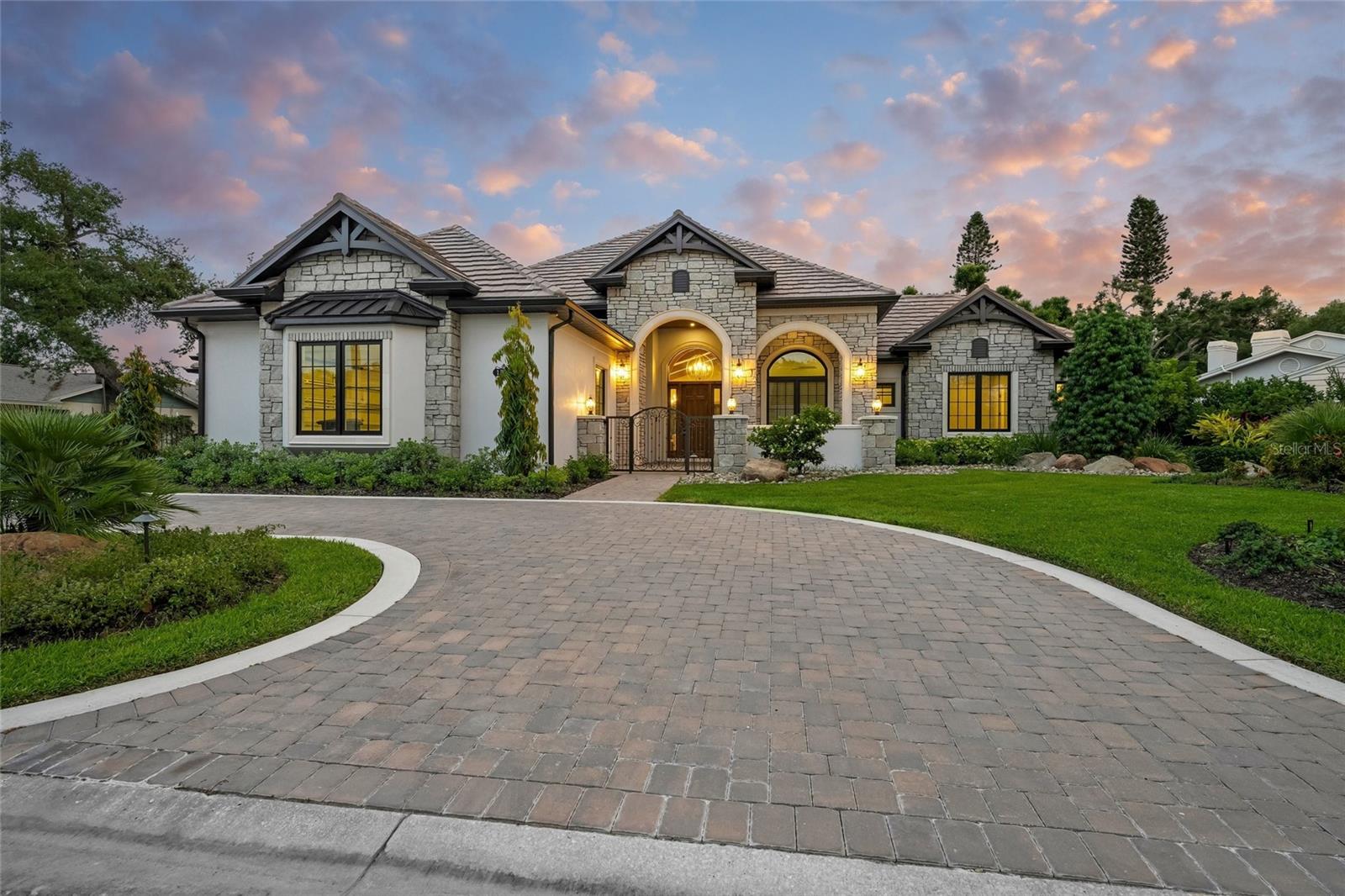 Behind one of Sarasota’s highly coveted Kentwood Estates, this extraordinary custom-built estate by award-winning Trinity Custom Homes delivers a level of luxury, craftsmanship, and architectural sophistication rarely seen in today’s market. From the moment you arrive along the sweeping circular driveway, the residence commands attention with its striking stone facade, dramatic rooflines, and manicured grounds, evoking the presence of a five-star private resort. Perfectly positioned on a serene lakefront homesite just moments from Siesta Key and Sarasota’s renowned waterfront lifestyle, this one-of-a-kind property was masterfully designed for the buyer who expects exceptional quality, timeless design, and elevated everyday living.

Built with superior construction standards and cutting-edge technology, the home showcases Timberstrand engineered framing for long-term structural integrity, precision layout using a Trimble HP printer robot, and expert masonry by BMMI (Bob Miller Masonry), ensuring both durability and refined exterior detail. Andersen windows and exterior doors provide energy efficiency, storm resilience, and timeless design, while ISO insulation, enhances year-round comfort and performance.

Inside, soaring vaulted ceilings with exposed architectural beams create a breathtaking first impression, while walls of glass frame tranquil water views and flood the home with natural light. The expansive open-concept floor plan blends warmth and sophistication, featuring wide-plank engineered hardwood flooring, solid custom poplar trim, solid-core Trustile interior doors, designer lighting, and curated high-end finishes throughout. The great room is anchored by a dramatic floor-to-ceiling stone fireplace, flowing seamlessly into the showpiece chef’s kitchen.

Designed to rival the finest luxury residences, the gourmet kitchen features oversized dual waterfall islands, solid-ply Crystal Cabinetry, premium appliances, elegant stone countertops, designer backsplash details, double wall ovens, and a fully equipped wet bar—ideal for entertaining at the highest level.

The luxurious owner’s retreat offers a private sanctuary with serene lake views, direct outdoor access, custom ceiling details, and a spa-inspired bath complete with dual vanities, a freestanding soaking tub, oversized walk-in shower featuring a Kerdi waterproofing system, and sophisticated designer finishes. Four additional bedrooms, a private den, and 5.5 beautifully appointed bathrooms provide exceptional comfort and flexibility for family and guests.

Outdoor living is equally impressive, with an expansive screened lanai showcasing a resort-style pool and spa overlooking sparkling lake views and lush tropical landscaping. A fully equipped outdoor kitchen and multiple covered lounge areas create the perfect setting for both grand entertaining and quiet relaxation. Additional features include a whole-home generator, oversized garage space, and a PEX plumbing system for enhanced efficiency, durability, and long-term reliability.

Located west of the Trail in one of Sarasota’s most desirable luxury neighborhoods, Kentwood Estates offers unparalleled proximity to Siesta Key Beach, Southside Village, downtown Sarasota, premier dining, shopping, marinas, golf courses, and top-rated schools. This is more than a home, it is a statement property defined by elite craftsmanship, advanced building techniques, and luxury living in the heart of Sarasota.