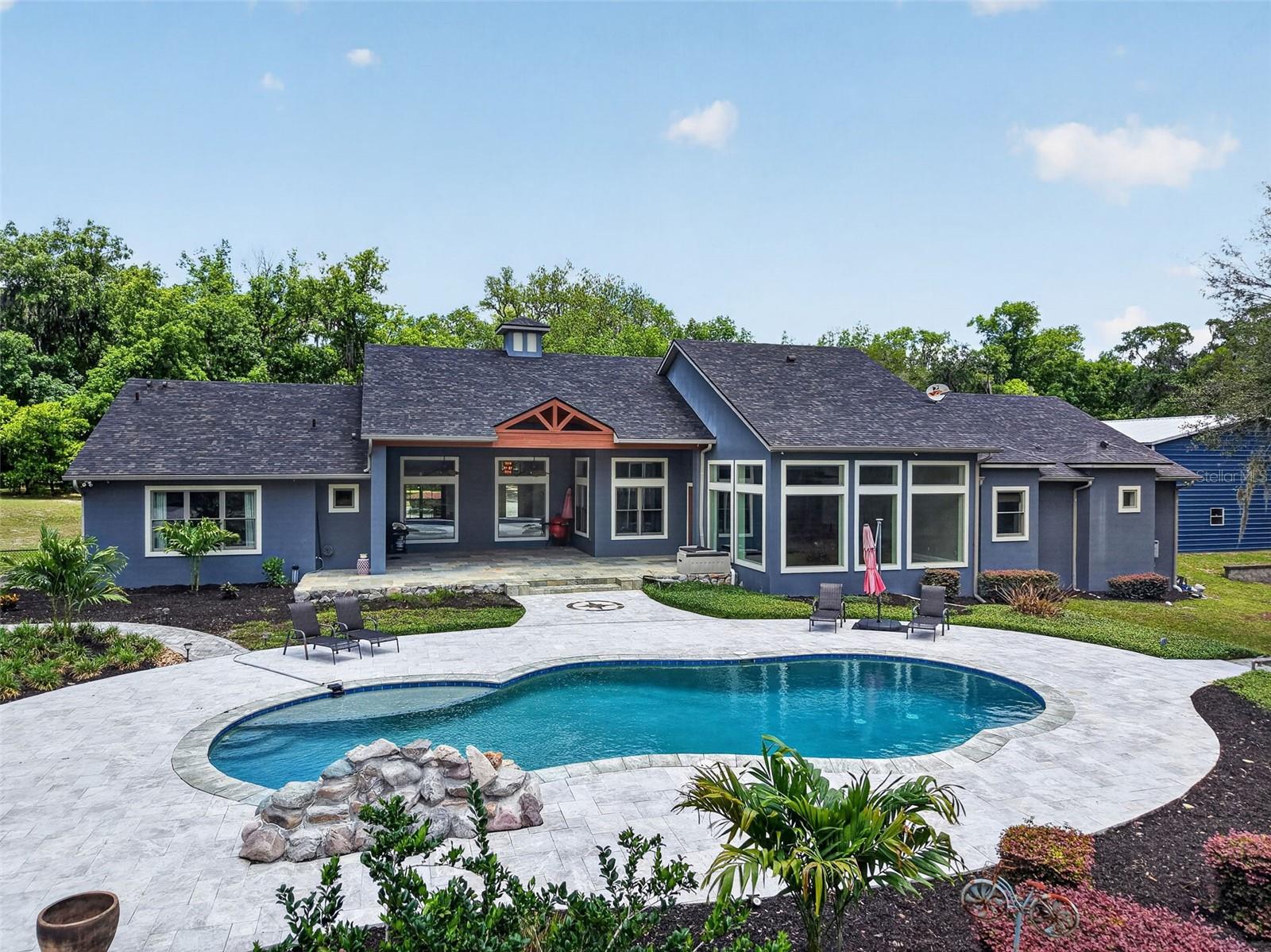 Stylish and timeless, this Southern Living Idea House was custom built in 2008 and is privately nestled on 5 high and dry, fully fenced acres zoned for horses in beautiful DeLand, Florida with NO HOA. This exceptional 4-bedroom, 6-bath estate featuring a 2020 insulated 40 x 60 warehouse with two bay doors, heated saltwater resort style pool with new spa added in 2020 and a 2020 outdoor pavilion perfectly blends luxury, craftsmanship, privacy, and functionality while offering convenient access to downtown DeLand, the St. Johns River, bike and riding trails, shopping, dining, I-4, and Florida’s beaches and attractions. From the moment you arrive, the attention to detail is undeniable — featuring Pella wood insulated windows, wood flooring, crown molding, tray ceilings, whole-home audio, in-wall vacuum system, fresh interior paint, newly added floor to ceiling windows in living room and a newer roof installed in 2024. Designed for entertaining, the home features a spacious game room, private 6-seat movie theatre room complete with a half bath and kitchenette, and an expansive open-concept layout ideal for hosting gatherings. The chef’s kitchen is a dream with premium gas stove appliance, custom cabinetry, granite breakfast bar, butler’s pantry, bar space, and dedicated workspace.  The inviting living room centers around oversized picture windows overlooking the stunning outdoor living space. Step outside to your private resort-style saltwater pool, outdoor pavilion, and expansive backyard retreat perfect for year-round Florida living. The luxurious primary suite offers a spa-inspired experience with a Jacuzzi tub, oversized pass-through shower featuring dual Moen shower heads and seven valves, dual oversized closets with custom shelving systems, and stackable washer/dryer hookup. The thoughtfully designed split floor plan provides privacy with the additional bedrooms located opposite the primary suite, including a private guest suite featuring its own en-suite bathroom and private exterior entrance — ideal for guests, multigenerational living, or a home office setup. The remaining bedrooms are connected by a Jack-and-Jill bathroom, and all bedrooms feature walk-in closets with custom shelving systems. Car enthusiasts, hobbyists, and business owners alike will appreciate the massive insulated  40x60 warehouse with two electric bay doors along with two oversized two-car garages,  offering endless storage and workspace possibilities. The newly built outdoor pavilion (25 x 50) features two oversized fans and electricity for all of your entertaining needs. 
Additional upgrades added spa with waterfalls, Ham Radio, security system, automatic viking gated entrance, transferable termite bond, reverse osmosis kitchen water purification system and countless luxury touches throughout. This truly one-of-a-kind estate must be experienced in person to fully appreciate the quality, privacy, and lifestyle it offers.
