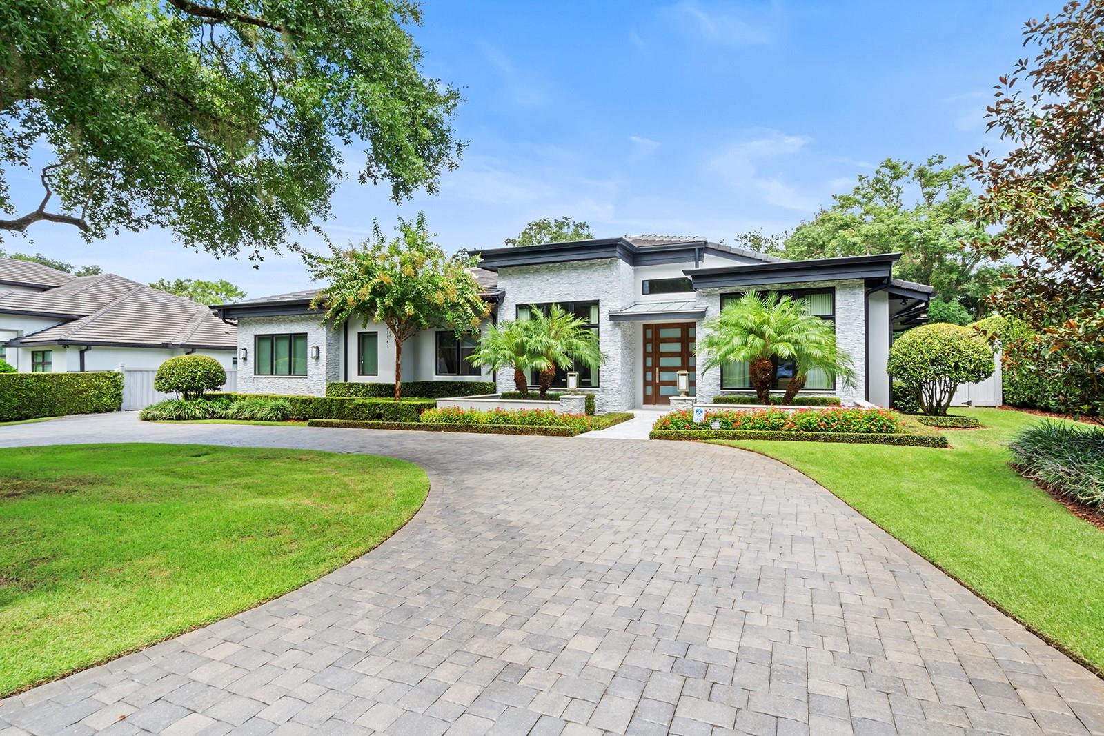 Welcome to this stunning well-appointed home in the highly desirable Via's of Winter Park. This one-level home offers a blend of modern design, luxury and functionality. Nestled on a tree-lined street, this four-bedroom, four-bathroom home with two-half baths is designed for comfort and entertaining. Upon entering you are immersed in 25-foot-high ceilings and greeted by an expansive, light-filled space featuring gorgeous hardwood floors in all main rooms of the home. With custom details throughout, the main living room has custom built-in shelving and a remote-controlled fireplace. The dining room showcases a beautiful, custom wood drop-ceiling feature, elegant chandelier, custom drapes and remote-controlled blinds, plus a show stopping glass-enclosed wine cellar with wine refrigerator and dimmable LED lights. The chef’s kitchen is a culinary masterpiece with extra-tall cabinetry, and has an enclosed coffee station, over and under dimmable lighting, Thermador appliances including a six-burner natural gas range/oven, a second built-in convection oven, microwave, and two full-size dishwashers along with a huge walk-in pantry with custom shelving. The oversized quartzite island features a large sink and room for plenty of seating. A separate breakfast area creates an inviting space for casual dining and entertaining. The primary suite is made extra private by the split plan layout and features an open yet separate 7-by-10-foot flex space for a reading nook, an exercise area, a desk for extra office use or a makeup vanity area. The bedroom with wood floors has a custom wood accent wall with dimmable LED lighting along with the home's signature private outdoor shower. The spacious, open spa-like bath includes separate vanities, tons of storage at each sink, two separate water closets, one with a bidet, a modern soaking tub, and large marble walk-in shower with body sprays. The two extra large walk-in closets with custom built-ins ensure ample wardrobe and storage space. All additional bedrooms are spacious with full en-suite baths and walk-in closets with custom built-ins. The dedicated office offers a large viewing window, wall mounted TV, built-in shelving and cabinets, custom leather-look wallpaper and remote-controlled blinds with custom drapes. The outdoor living space is equally impressive featuring a covered lanai and a full summer kitchen with grill, marble countertops and flooring, an oversized ceiling fan and large screened TV. The pool and spa, controlled by Aqua Link App, provides tranquility and relaxation with a waterfall feature and safety screens. Additional features of the home include a Lutron lighting system with app control, Sonos speaker in all main rooms including outdoor lanai, custom window treatments and custom lighting throughout. The oversized yard is meticulously landscaped and is made extra private by the low-maintenance vinyl fence. The attached oversized two-car garage includes custom shelving and a finished air-conditioned attic for extra storage. This stunning property is ideally just steps from Winter Park Racquet Club and within proximity to the renowned shopping and unique dining options on Park Avenue. With easy access to downtown Orlando, and sporting and entertainment venues, there is also access to Orlando’s International Airport and the area’s famous theme parks. This home, which has too many features to list, offers the best of luxury and convenience.
