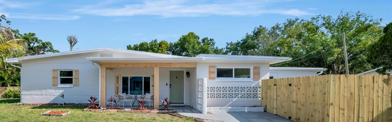 Welcome to this beautifully updated mid-century block home in the heart of St. Petersburg. Thoughtfully refreshed inside and out, the home blends classic Florida charm with modern finishes, from the painted brick exterior, cedar-accented covered front porch, and signature breeze-block detail to the crisp, light-filled interior. Inside you'll find 3 bedrooms, 2 full baths, and 1,354 square feet of tile-floored living space. The updated kitchen features shaker cabinetry, granite countertops, and stainless steel appliances, and opens to an expansive dining and gathering room with sliding glass doors to the backyard. The split floor plan places the primary suite on its own wing, complete with a walk-in closet, a stylish step-in shower with mosaic tile accent, and its own slider to the yard. Two additional bedrooms share an updated hall bath with tub and decorative tile, and an interior laundry area with stacked washer and dryer adds everyday convenience. Outside, a fully fenced backyard with mature shade trees, an open patio, and fresh landscaping provides plenty of room to relax, garden, or entertain. Centrally located minutes from downtown St. Petersburg, Tyrone-area shopping and dining, parks, and the Gulf beaches, this move-in-ready home puts the best of the city within easy reach.