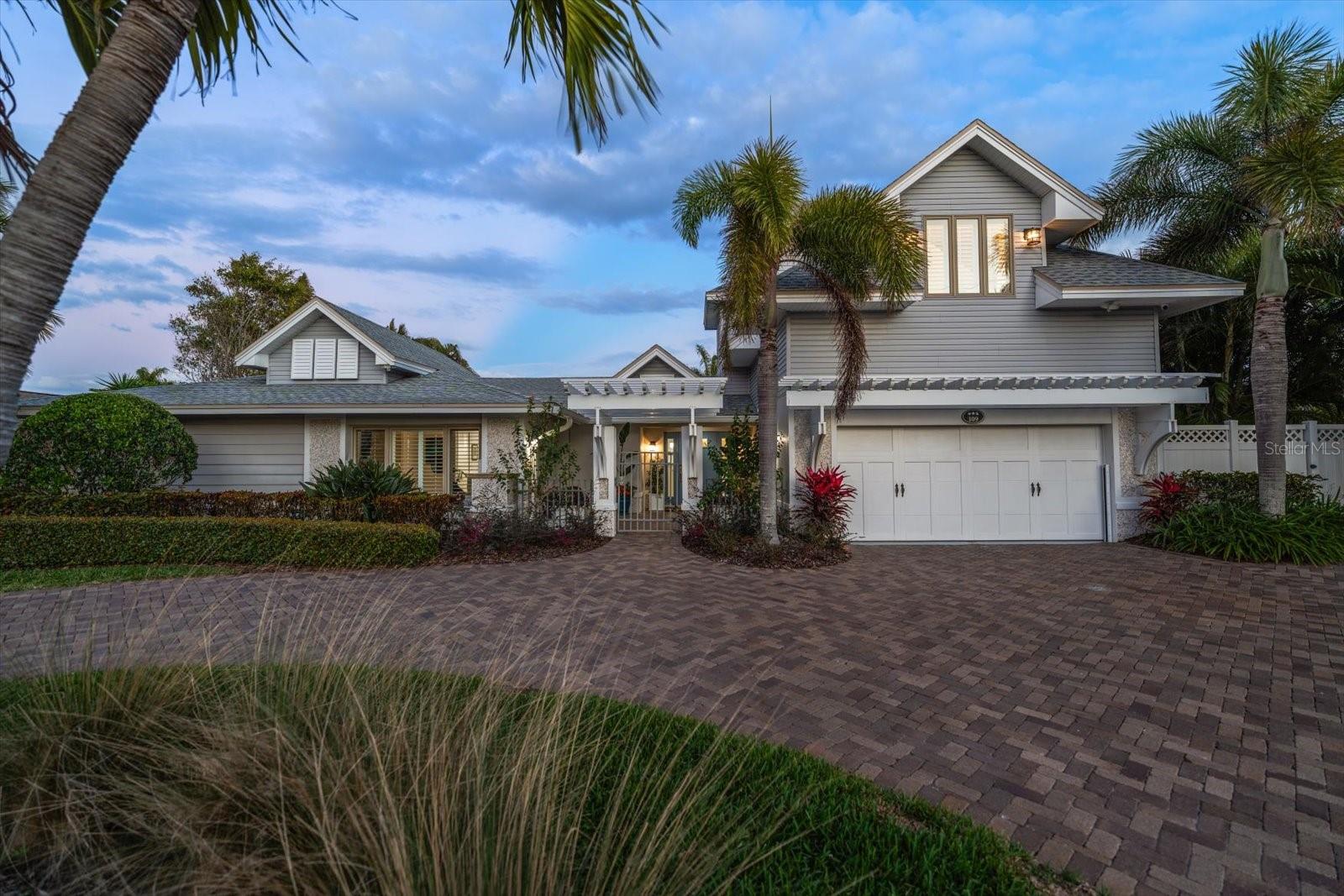 Perfectly poised in the highly sought-after Harbor Bluffs, this stunning move-in ready waterfront residence offers the ultimate blend of luxury, comfort, and effortless Florida living. From the moment you arrive, the pavered circular driveway and welcoming courtyard create unforgettable curb appeal, setting the tone for the designer finishes found throughout. Inside, limestone floors flow through an open, light-filled interior where a striking family room with a beamed ceiling and a dramatic wall of sliders seamlessly connects indoor and outdoor living. Step outside to your backyard oasis—fully fenced for privacy—where a beautifully refinished pool with elegant marble pavers and a spillover spa create a true resort-style setting. Designed for unforgettable entertaining, this outdoor retreat offers expansive lounging areas and seamless access from multiple rooms of the home. Double doors reveal a versatile flex room—ideal as a home gym, craft studio, or additional bedroom—with a full bath conveniently nearby. The showstopping dine-in kitchen is a chef’s dream, featuring quartz countertops, a six-burner gas range, double ovens, a Bosch dishwasher, pantry, oversized island with prep sink, and a breakfast bar illuminated by elegant pendant lighting. A stylish dry bar with wine fridge and abundant storage, along with a charming coffee bar for relaxed poolside mornings, elevate everyday living. Sliders off the dining area open directly to the pool, enhancing the home’s seamless flow, while a dedicated office provides quiet productivity. The exquisite primary suite is a serene retreat filled with natural light and private pool access. Its spa-inspired ensuite boasts dual vanities, custom tilework, a jetted tub, walk-in shower, and an extraordinary custom walk-in closet with built-ins and center island. Each additional bedroom is spacious and well-appointed with its own ensuite bath. Upstairs, a flexible bonus space—currently a billiard room—offers a full bath and kitchenette with beverage area, refrigerator, and disposal, making it ideal for guests or multigenerational living. For boating enthusiasts, this property is a true paradise, set on protected water and complete with a 14,000-pound boat lift that accommodates a 24–26 ft boat, providing quick access to open water and endless days cruising the Intracoastal. With a whole-house generator, tankless water heater, flood barriers for every opening, a newer roof, and a quiet location close to dining, shopping, and the area’s beautiful beaches, this exceptional waterfront home truly has it all.