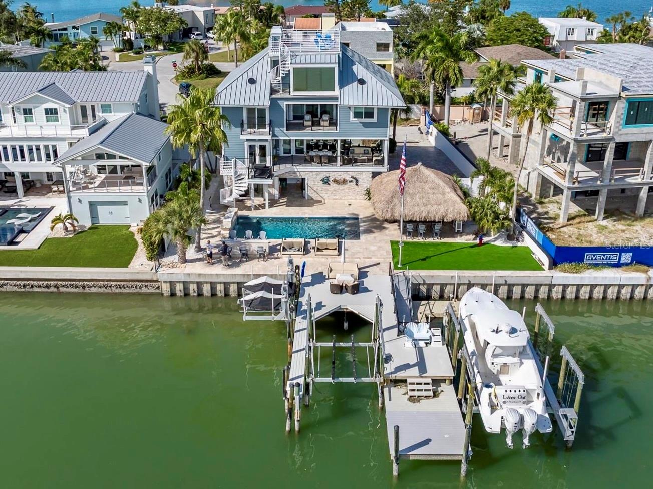 85ft OF WATER FRONTAGE | 2 BOAT LIFTS | 2 JETSKI LIFTS | PANORAMIC WATERVIEWS | PRIVATE ELEVATOR. Welcome to the most remarkable waterfront residences on St. Pete Beach, where coastal living, craftsmanship, and pure relaxation unite. The ultimate outdoor experience while maintaining peace of mind with full elevation, impact-rated windows and doors, and an outdoor oasis that surpasses every expectation. Step onto your own PRIVATE MARINA with an expansive composite dock featuring two boat lifts (30K and 10K), dual jet ski lifts, water, electric, newer seawall, and a fish-cleaning station for your fresh catch. Located on the Intracoastal waterway with quick Gulf access this is a fisherman/boater's dream. The backyard transforms into a resort-style escape with a SALTWATER PEBBLE TECH POOL featuring three cascading waterfalls, in-water seating, a sun shelf, and a heater/chiller system for ideal comfort in every season. Surrounding it all is elegant Travertine tile connecting multiple entertaining areas, a massive authentic TIKI HUT (22' x 24'), and low-maintenance artificial turf ensures your time is spent relaxing, not mowing. Step through the custom front door and enter into 3,489 square feet of luxurious living space (4,856 Total Gross Area) where an abundance of light fills every room, high ceilings and uninterrupted water vistas through floor-to-ceiling hurricane-rated frameless windows. The open-concept great room boasts a custom bar accented with wood trim and complete with its own refrigerator and sink. Designed for the modern chef, the custom kitchen boasts stainless-steel cabinetry, Quartz counters, four THOR refrigerator drawers, and premium stainless-steel appliances throughout. A dining area, half bath, and a butler’s pantry/utility room complete this level. The second-level covered porch overlooks the INTRACOASTAL and is complete with tongue and groove wood ceilings, tile floors, ceiling fans, electric shades, and a built-in propane gas connection for your grill. Enjoy Sonos-powered music throughout every level, inside and out. The third floor offers a split-bedroom layout with a cozy entertainment lounge and fireplace with sliders leading the third level covered balcony. Two guest bedrooms share a well-appointed bath, while the primary suite enjoys dual closets, a gas fireplace, and a private balcony. It's SPA-INSPIRED bathroom completes the retreat with sophistication and serenity. The fourth floor presents a versatile guest suite with its own bath, an all-glass sitting area, plus direct access to the ROOFTOP DECK which is the highest residential vantage point in St. Pete Beach. From here, take in 360-degree panoramas of downtown St. Petersburg, Tropicana Field, the Don CeSar, Boca Ciega Bay, and the Gulf. This deck is the ultimate perch for sunrise coffees, sunset toasts, and dolphin watching. The ground floor has a two-car garage, dual storage rooms, a bar area with roll-up door to the pool, a bonus recreation room, and a full bath. The oversized paver driveway offers ample space to accommodate multiple vehicles with ease. The entire exterior was reimagined with maintenance free Hardie Plank siding, new eaves, PVC fascia, gutters, and lifetime metal roof (2025), all designed for durability and style. Every surface of this home has been thoughtfully upgraded with precision and purpose. This is not just another waterfront home, it’s a custom-crafted sanctuary designed for those who want to live every day like a vacation.