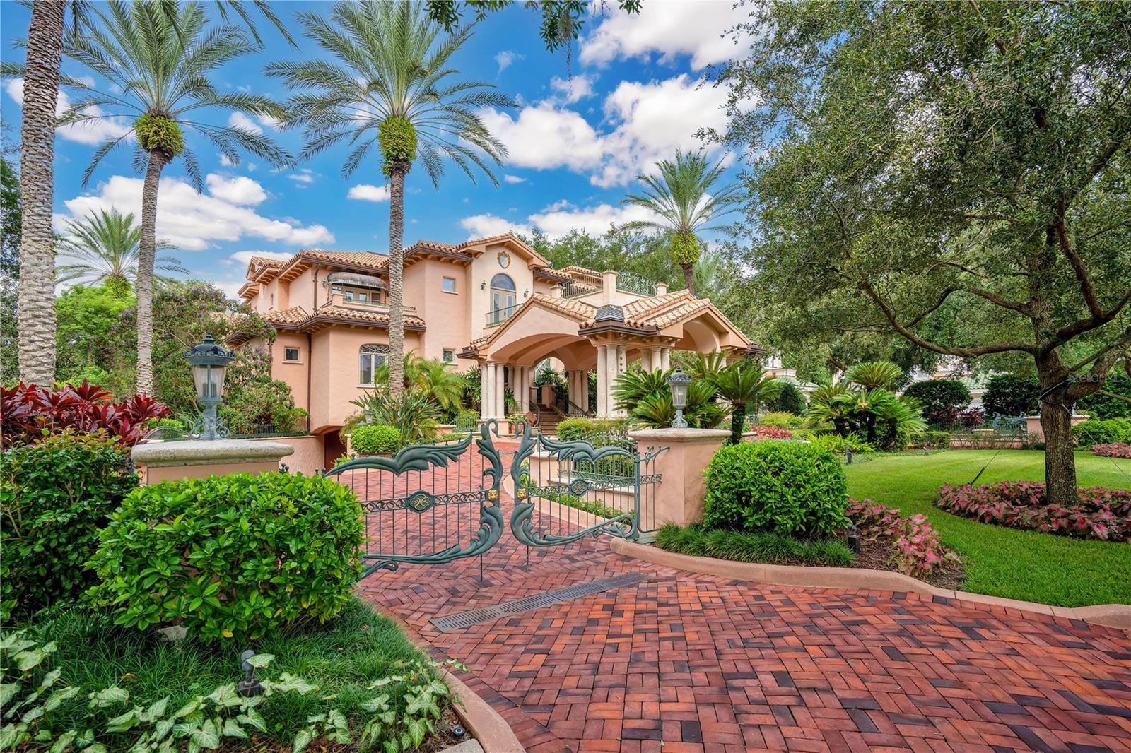 Nestled on the shores of Lake Butler, Puesta del Sol is a masterpiece of design and luxury, just a short walk from the renowned Isleworth Golf & Country Club. Named for the breathtaking sunsets visible from its many terraces, this estate was crafted for grand entertaining and elegant living.

From the bold elegance of the grand porte-cochère entry to the graceful curves of its architectural design, every detail reflects sophistication. Rich finishes of granite, Botticino marble, stone, and iron create a timeless aesthetic, while soaring 26-foot ceilings in the living room highlight the stunning coquina and limestone fireplace. The family room is a refined retreat, complete with a custom bar and fireplace.

The art deco-inspired primary suite offers a private terrace and a balcony overlooking the living room, creating a serene sanctuary. Meanwhile, the Orchid Room, adorned with intricate depictions of exotic species, opens to a 750-square-foot pool, featuring a “Rainbow” Bridge and swim-up bar. Adjacent, a private steam room and sauna provide ultimate relaxation.

An enchanting wine cellar, secured by custom iron gates and dramatic torchieres, accommodates 1,500 bottles—a connoisseur’s dream. The convenience of an elevator seamlessly connects the kitchen to the 7,800-square-foot air-conditioned underground garage, ensuring effortless living.

Beyond, a double-gated entry leads to the boathouse, offering direct access to the Butler Chain of Lakes—13 interconnected lakes where natural Florida beauty meets the magic of nightly fireworks.

For those who seek the very best, Puesta del Sol is an unparalleled opportunity to own a true architectural gem. Discover this breathtaking estate and make it your own.