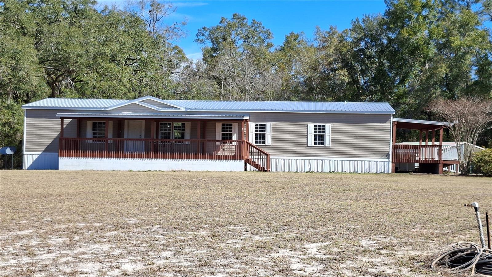 This 5 acre parcel has it all. Starting with a well maintained double wide, this beauty has fresh paint, newly installed Luxury vinyl plank throughout, a new stove and a new metal roof installed in 2025. Originally designed as a 4/2. This unit Combined two of the secondary bedrooms into one large bedroom 21' long, lending itself to many possibilities. Additionally, many handicap accessible features are incorporated, including an inclined walkway to the side entrance, a walk in tub in the primary bath plus many other accessible features throughout.. This lovely property, located just over the Tax friendly Gilcrest County Line, and has paved road frontage. Come watch the sunsets, check out the wildlife, walk in the forested portion of this beautiful property's Granddaddy Oaks, or just enjoy the view with quiet country living on any one of 3 ample covered decks (10'x27', 12'x16 or 10'x36')! Convenient to both Lake City and Gainesville. This area boasts superior recreational activities as well as access to world class healthcare. Ginnie Springs Outdoors LLC , Ruth Kirby Park, The Santa Fe, Ichetucknee Springs State Park, and Suwannee Rives are all within easy driving distance offering something for everyone. Dimensions of interior rooms are approximations believed to be accurate, owner supplied