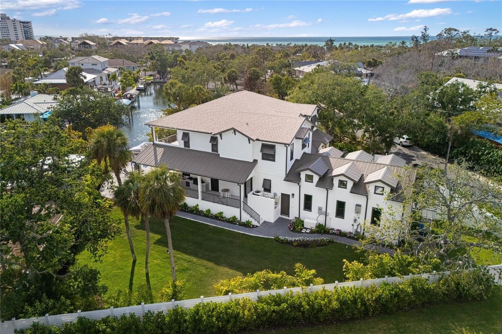 Start living your dream lifestyle on world-famous Siesta Key in this Pham Development custom-built waterfront British West Indies–style home. Located on a quiet street on the north end of the key—close to the beach, Siesta Key Village and Out-of-Door Academy—and just minutes on and off the island, this residence offers island living at its best. Set on a corner canal-front lot, the two-story home features 5 bedrooms, 5 full bathrooms and 1 half bath, with 3,875 square feet under air, a great room floor plan, soaring 22-foot vaulted ceilings, and walls of windows and doors—including large pocket sliders—that bring in abundant natural light and seamlessly connect indoor and outdoor living.

The adjacent dining area provides ample space for entertaining, while the stunning kitchen—completely open to the great room—serves as the heart of the home with a large 9-foot island with extended seating, professional stainless steel gas appliances and a walk-in butler’s pantry. The home also features a fully integrated security system, whole-home sound system and a complete Control4 smart home system. The first-floor owner’s suite offers a private retreat with a walk-in shower, freestanding tub, dual vanities, and a large custom walk-in closet. A laundry room, powder room and mudroom complete the first level, and a 3-car garage provides ample parking and storage.

Upstairs you’ll find four en-suite guest bedrooms, an additional laundry area to service them, and an expansive second-level balcony to take in the views. Outdoor living includes approximately 1,502 square feet of covered lanai, an exterior wrap-around porch, and balcony space designed for enjoying the island lifestyle, complete with SunBrite outdoor TVs, and Brazilian hardwood ceilings. The privately gated driveway and fully fenced property are surrounded by lush landscaping, creating a secluded tropical setting with a large swimming pool, champagne spa and expansive pool deck perfect for relaxing or entertaining. A private well supports irrigation. With 31 linear feet of canal frontage, the property features a 31-by-12-foot electric boat lift rated for 6,500 pounds, two jet ski ramps and about a 4.5-foot draft—ideal for boating and enjoying the water, making this oasis the perfect place to enjoy the Siesta Key lifestyle.