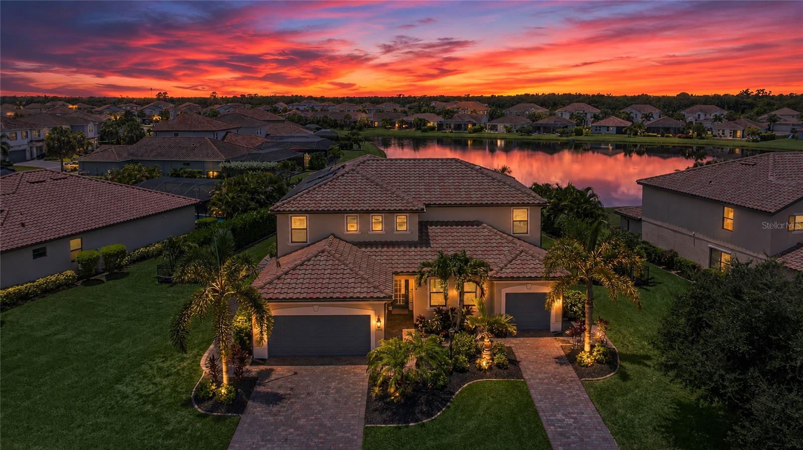 This stunning 4300+ sq ft. Next Gen home® is perfectly situated on a ¼-acre premium waterfront lot in Lakewood Ranch—one of the nation’s top award-winning master-planned communities. The highly sought-after fully upgraded Liberation model offers an exceptional blend of space and versatility, combining main living with a fully private suite that is ideal for multigenerational living, overnight guests, or a young adult who wants the privacy of their own space while still living at home. Entertain guests in this stunning home with beautiful water views in the open floor plan featuring a large updated kitchen with high-end Bertazzoni stainless steel appliances, a gas stove, quartz countertops, abundant cabinetry, and an island that opens to the roomy living room. Just off the kitchen, a versatile flex room can easily serve as a formal dining room, sitting area, playroom, or home office. Step outside to the extended screened lanai where a refreshing heated pool and spa with LED lighting create the perfect setting to relax or entertain while enjoying the tranquil waterfront backdrop. Enjoy exceptional curb appeal with over $60,000 in professionally designed landscaping, custom landscape up-lighting, and lush tropical surroundings that provide outstanding beauty and exceptional privacy. Upstairs, you’ll find 5 additional generously sized bedrooms—including the large primary suite—along with a spacious bonus room and conveniently located laundry room. The primary retreat features an over-sized walk-in closet, dual vanities, a soaking tub, and a separate walk-in shower. The private Next Gen suite offers its own entrance and functions like a home within a home, complete with a comfortable living room with built in Murphy hideaway bed, kitchenette with breakfast nook, wine fridge, generously sized private bedroom, walk-in closet, full bath, in-suite washer and dryer, private lanai access, and a dedicated one-car garage. Thoughtful upgrades throughout include Luxury Vinyl Plank (LVP), Plantation shutters with custom window trim, and custom woodwork throughout home, crown molding, custom drop zone, custom overhead storage systems in both garages with epoxy flooring, ceiling fans, Tesla® Solar Panels, and 2 Tesla Powerwall® backup battery systems that keeps your home powered during outages—eliminating the need for a traditional noisy backup generator while helping reduce utility costs. Located in the highly desirable gated community of Savanna at Lakewood Ranch, residents enjoy resort-style amenities including a clubhouse, fitness center, resort-style pool, playground, dog park, basketball court, and scenic walking trails. Ideally positioned just minutes from A-rated schools, upscale dining, and premier shopping, this home also offers convenient access to the stunning Gulf Coast beaches of Anna Maria Island and Siesta Key—both renowned for their white sand and crystal-clear turquoise waters.