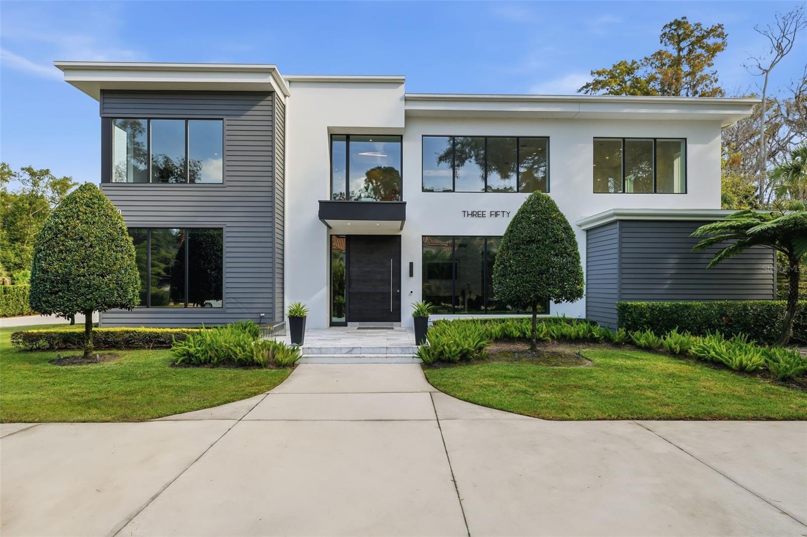 Nestled within the 9-acre Lake Maitland Owl Preserve, this striking contemporary residence—crafted by acclaimed green builder E2 Homes offers a rare blend of architectural distinction, privacy, and natural beauty. Surrounded by protected conservation land, the home delivers a serene retreat just minutes from the vibrant lifestyle of Winter Park.  Designed by internationally recognized architect Jose Vengas, the home showcases dramatic ceiling heights, clean modern lines, and expansive glass walls that flood the interiors with natural light while blurring the line between indoor and outdoor living. The thoughtfully designed open-concept floor plan centers around a show-stopping chef’s kitchen featuring custom cabinetry, a statement marble backsplash, and a full suite of premium Sub-Zero and Wolf appliances perfect for both elevated entertaining and everyday living.  Living and dining spaces flow effortlessly to a covered outdoor lounge with a fully equipped summer kitchen, overlooking a resort-style pool and spa designed for year-round enjoyment. Whether hosting guests or unwinding in private, this outdoor sanctuary is truly exceptional.  All five bedrooms are generously sized private suites, each offering spa-inspired bathrooms with refined finishes and custom detailing. The primary suite is a true retreat, featuring a luxurious bath experience and expansive walk-in closets designed for both beauty and function. A first-floor owner’s suite provides exceptional flexibility for multi-generational living or guest accommodations, while the upper level reveals gallery-style walkways and an elegant terrace that highlights the home’s architectural artistry.
With nearly 5,000 square feet of meticulously curated living space, this exceptional estate delivers modern sophistication in one of Central Florida’s most exclusive and private enclaves—just moments from Winter Park’s renowned dining, boutiques, and cultural destinations.